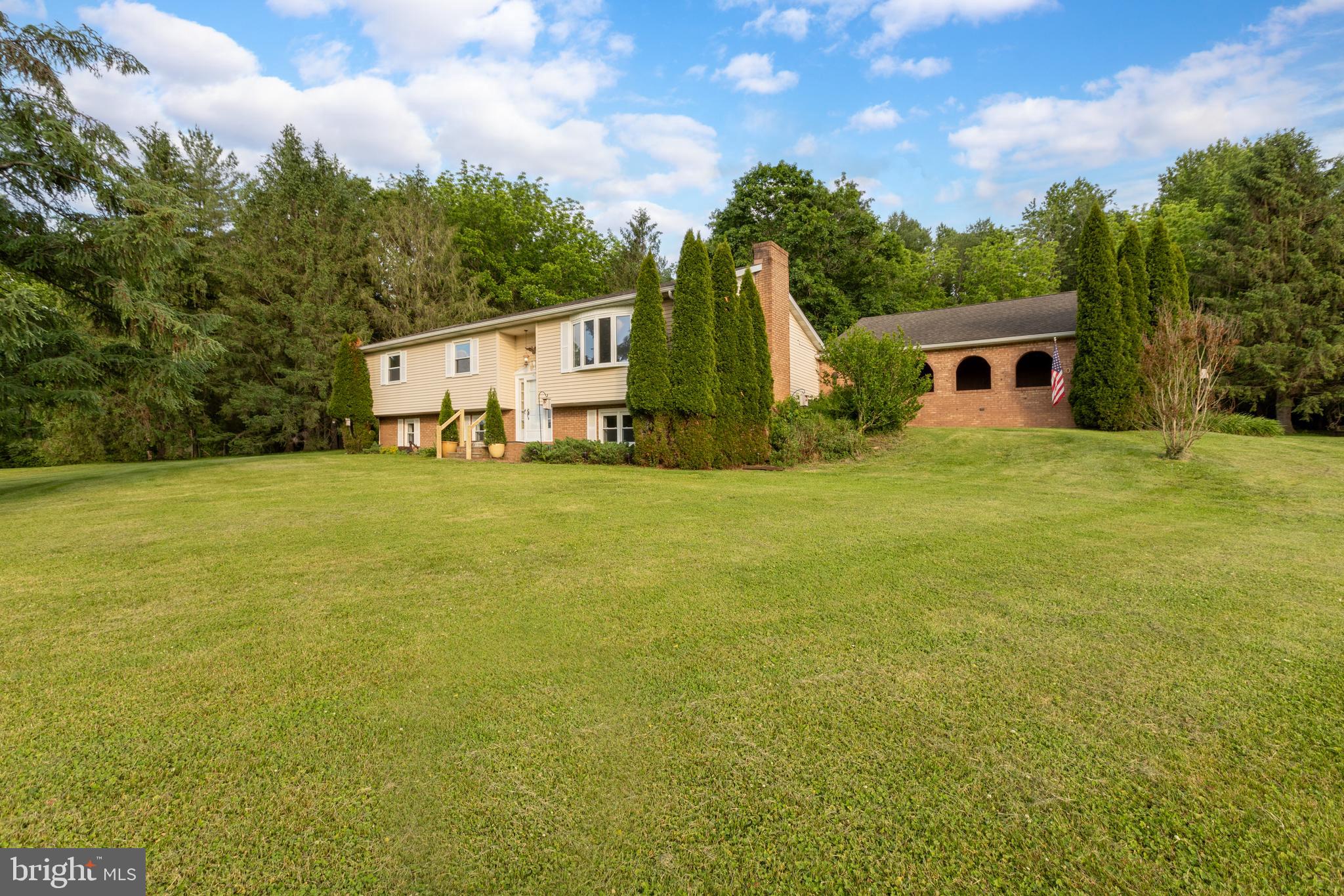 Nestled on a cul-de-sac in desirable Kennett Township, just minutes from the vibrant Borough of Kennett Square, this spacious 4-bedroom, 2.5-bath bi-level home offers the perfect blend of privacy, space, and opportunity. Situated on over an acre of beautifully landscaped grounds, this property is surrounded by mature trees and stunning gardens, creating a peaceful retreat where neighboring homes are barely visible.
The backyard is truly exceptional, featuring an oversized patio, colorful flower beds, mature trees, and breathtaking views. Whether entertaining guests or enjoying a quiet evening outdoors, you'll appreciate the privacy and natural beauty that surrounds you. Inside, the home has been freshly painted throughout and features brand-new carpeting across the main level, along with new luxury vinyl flooring in the kitchen and both full bathrooms. The spacious kitchen offers stainless steel appliances, abundant workspace, and endless potential to customize and update to your personal style. The lower level provides an abundance of flexible living space, highlighted by a large family room with a dramatic floor-to-ceiling stone fireplace. Originally wood-burning and now equipped with a gas insert, it creates a warm and inviting gathering space. This level also includes a fourth bedroom or private office, plus an enormous recreation room complete with a wet bar and mini refrigerator. Owner used it as an art studio, this versatile space could easily serve as a game room, home gym, media room, hobby space, or additional entertaining area. Additional improvements include a new water treatment system installed in 2026 and a new driveway completed in 2022. The detached oversized garage is connected by a convenient breezeway, while the long driveway provides ample parking for family and guests. Enjoy the freedom of no HOA. The lane consists of just five homes, with property owners sharing maintenance responsibilities. Offering privacy galore, beautiful views, generous living spaces, and a prime location close to everything Kennett Square has to offer, this is a rare opportunity to create your dream home in one of Chester County's most sought-after settings.