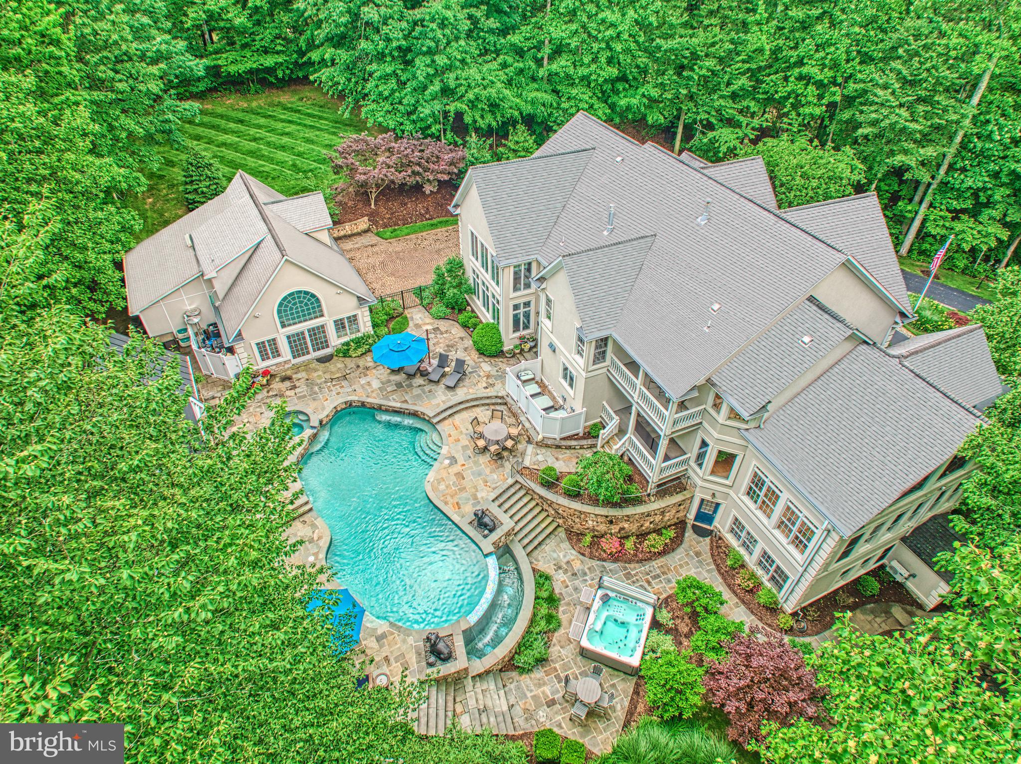 Tucked into more than five acres of wooded privacy, this exceptional residence invites you into a world of elegance, calm, and connection—with nature, with loved ones, and with home. From the moment you turn onto the tree-lined driveway, you’re transported. What unfolds beyond the trees is not just a home, but an experience—a seamless blend of refined living and resort-style amenities, thoughtfully designed for gathering, relaxing, and celebrating life.

Inside, the home opens with timeless warmth. The foyer flows effortlessly to formal living and dining spaces, where a dual-sided fireplace connects to a richly appointed home office—complete with a lofted library accessed by a wrought iron spiral staircase. Anchored by a chef’s dream kitchen, the heart of the home is both functional and beautiful. Custom Amish-built cabinetry, top-tier appliances, leathered quartz surfaces, and a stunning butcher block island come together beneath designer lighting and clever built-ins that maximize both utility and ambiance. A sleek butler’s pantry links the dining room and kitchen, complete with a beverage station and additional prep space.

Adjacent, the great room soars with beam-accented ceilings and a floor-to-ceiling stone fireplace, while diagonally laid wide-plank hardwoods add warmth and movement. The main level also features a well-appointed guest suite, ideal for visitors or multigenerational living.

Upstairs, the primary suite is a peaceful retreat with a cozy fireplace, private balcony access overlooking your home-Oasis, whisper-quiet motorized shades and a spa-inspired bath with custom cabinetry, quartz counters, and a rejuvenating shower panel. Three additional bedrooms each enjoy private en-suite baths, and a reimagined laundry room blends style with efficiency—complete with pet crates, basket cubbies, and granite worktops.

The walkout lower level is an entertainer’s playground: a custom bar with black leathered granite, kegerator, and multiple beverage stations sets the stage for movie nights or game days. A separate craft room with glass French doors and built-in shelving offers creative sanctuary, while the home gym provides daily wellness inspiration.

Step outside, and the magic truly expands. The pool and spa have been reimagined with flagstone, porcelain tile, and smart automation. Nearby, a freestanding hot tub offers additional relaxation. The koi pond has been lovingly restored and now sparkles with life, framed by vibrant landscape design featuring maples, redbuds, and flowering trees. Beyond, the outdoor pavilion is its own destination: over 1,000 square feet of vaulted, covered living and dining space with a full Viking outdoor kitchen, bar seating, stone fireplace, cherry wood ceilings, Big Air wet rated ceiling fans, and curated lighting to extend your evenings under the stars.

The beautifully finished pool house doubles as a guest cottage with its own kitchen, private HVAC system, luxury vinyl plank flooring, and epoxied garage flooring. A newly constructed 24'x14' shed offers elegant functionality with custom storage. The carriage house—part of the eight total garage bays—offers expansive attic storage with pull-down access.

Extensive hardscape and professional landscaping unify the property into a living, breathing retreat. Every element—from the asphalt drive and irrigation systems to the lighting, fencing, and flagstone walkways—has been considered, crafted, and curated.

This isn’t just a property—it’s a personal sanctuary designed to support the full rhythm of life: quiet mornings, lively celebrations, restful evenings, and the beauty of everyday living. Come experience a home that lives as beautifully as it looks.