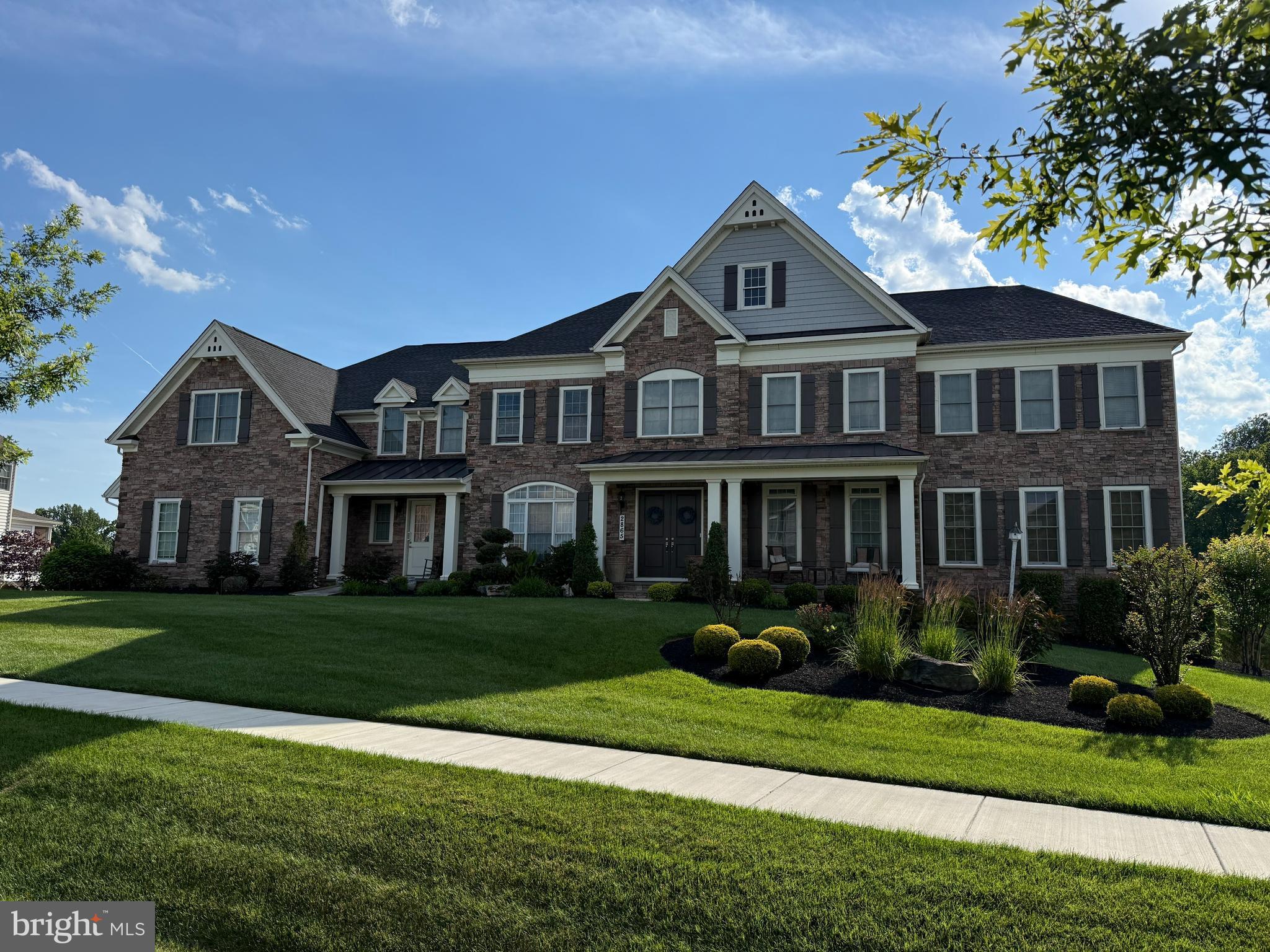 Near the end of a quiet street in Trotters Glen, this extraordinary Toll Brothers Craftsman estate immediately commands attention with its stone-clad exterior, dual front entrances, soaring 8-foot double doors, and unmistakable architectural presence. Set on a premium wooded homesite, the home offers more than 10,700 square feet of finished living space designed for both grand entertaining and everyday comfort. Inside, rich hardwood flooring, custom millwork, tray ceilings, and a breathtaking two-story great room with exposed beam ceilings create a sense of elegance at every turn. Natural light pours through expansive walls of glass, while oversized retractable sliders seamlessly connect the family room and gourmet kitchen to the composite deck overlooking panoramic wooded views. The result is an effortless indoor-outdoor lifestyle rarely found in the area. The kitchen is designed to impress, anchored by a massive double-width island, a 48-inch built-in Monogram refrigerator, stainless steel Monogram double wall ovens, a six-burner Monogram gas range, and a butler’s pantry. The conservatory adds a stunning gathering space filled with natural light, adjoining one of two private multi-generational suites on the main level providing exceptional flexibility.  The upper-level features four additional bedroom suites with private bathrooms and walk-in closets. The remarkable owner’s retreat has a sitting room, two-sided fireplace, dual boutique-style closets, and a spa-inspired bath centered around a freestanding soaking tub. The walk-out lower level extends the experience with a theater room, recreation spaces, second kitchen with bar, guest suite, patio access, and abundant storage. Conveniently located near Olney amenities, parks, golf, and MD-200, this is luxury living without compromise.