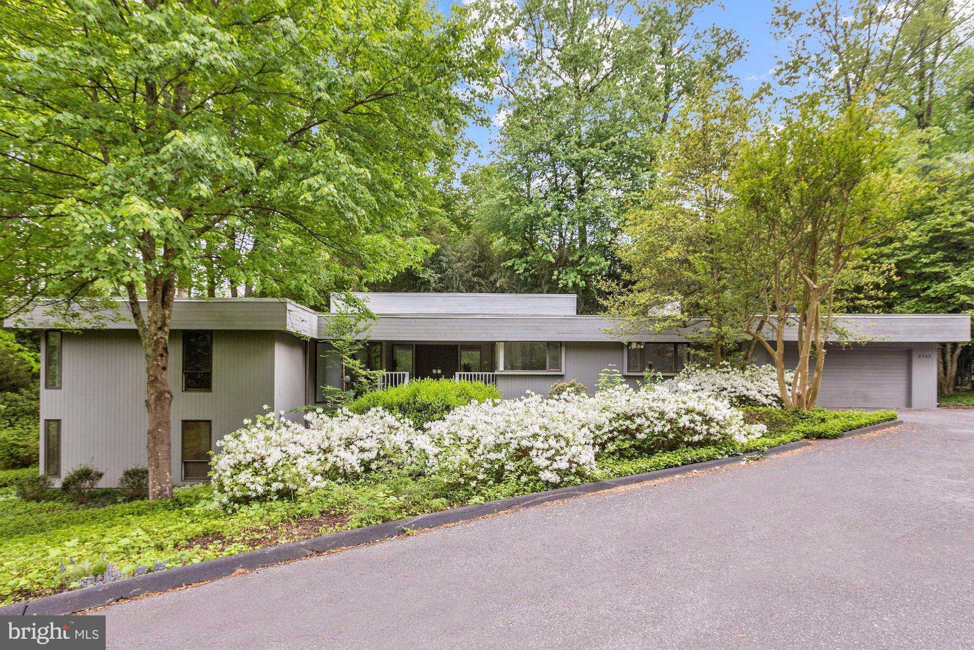 This stunning contemporary home is nestled on a generous lot and enjoys a park like setting with mature trees, plants and flowers that provide tranquility and privacy. A large and open entrance foyer with generous closets is the entry point for this mid-century  masterpiece. A breath taking living room and dining area with soaring ceilings is both elegant and functional. It features a wall of floor to ceiling windows and doors, natural light from two exposures and a fireplace. A spacious gourmet kitchen with table space for six and top of the line appliances is found just off of the dining area. The den is warm and inviting with a fireplace and a wall of windows and doors leading to the private outside deck. A wet bar hidden behind custom cabinetry adds a level of convenience and function to the den. The main level is also home to a generous owner's suite with an office/sitting space, ample closets and en suite bathroom complete with a dual vanity, shower and bath tub. The second bedroom is conveniently situated next to the owner's suite and has a large closet, light from two exposures and an en suite bathroom. The lower level features two impressive multi-function rooms offering tremendous flexibility. The main family room boasts a bar, light from several windows and doors leading to the gardens. Also on this level are two large bedrooms with closets and a full bath. A large two car garage that opens to the kitchen and main level laundry facilities allow for convenient and modern living.  Just steps away is the community swimming pool with club house as well as two lighted tennis courts which serve this boutique enclave exclusively.