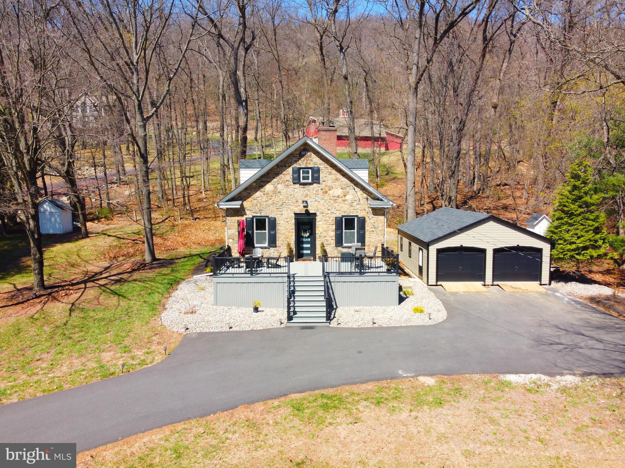 Here’s your opportunity to own a truly special piece of history, beautifully appointed with tasteful modern flair. A pair of stone pillars—constructed during the Roosevelt-era WPA program—stand at the end of the drive, offering a stately welcome to this remarkable natural stone home, originally built in 1897 as a one-room schoolhouse. The main level showcases soaring ceilings, exposed beams, and deep window sills that bathe the space in natural light. A spacious great room serves as the centerpiece, complemented by two generously sized bedrooms and a full bath featuring double sinks and a tiled walk-in shower. The lower level forms the heart of the home, where a well-designed kitchen offers abundant prep space, ample cabinetry, and new stainless steel appliances. Adjacent dining and family rooms create an inviting setting for everyday living and entertaining, highlighted by a cozy pellet stove. A convenient half bath and laundry area complete this level. Upstairs, two additional bedrooms and an updated full bath provide flexible space for guests, family, or a home office. Outside, the property continues to impress. A 32' x 24' detached garage easily accommodates SUVs while offering additional storage. The grounds are rich in character, outlined by historic stone pillar and metal cable fencing, with mature trees framing the expansive front and side yards. Three additional outbuildings provide even more storage and versatility. Set along a quiet township road, this unique property offers peaceful surroundings with easy access to major routes, shopping, and dining. Whether you're seeking a full-time residence or a scenic weekend retreat, this one-of-a-kind home delivers charm, history, and modern comfort in equal measure.
