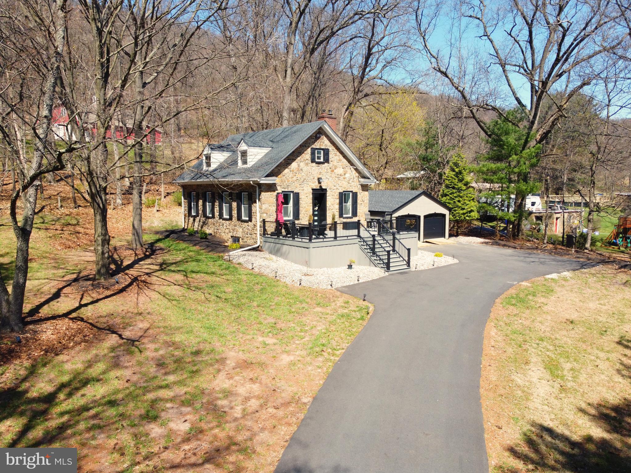 Here’s your opportunity to own a truly special piece of history, beautifully appointed with tasteful modern flair. A pair of stone pillars—constructed during the Roosevelt-era WPA program—stand at the end of the drive, offering a stately welcome to this remarkable natural stone home, originally built in 1897 as a one-room schoolhouse. The main level showcases soaring ceilings, exposed beams, and deep window sills that bathe the space in natural light. A spacious great room serves as the centerpiece, complemented by two generously sized bedrooms and a full bath featuring double sinks and a tiled walk-in shower. The lower level forms the heart of the home, where a well-designed kitchen offers abundant prep space, ample cabinetry, and new stainless steel appliances. Adjacent dining and family rooms create an inviting setting for everyday living and entertaining, highlighted by a cozy pellet stove. A convenient half bath and laundry area complete this level. Upstairs, two additional bedrooms and an updated full bath provide flexible space for guests, family, or a home office. Outside, the property continues to impress. A 32' x 24' detached garage easily accommodates SUVs while offering additional storage. The grounds are rich in character, outlined by historic stone pillar and metal cable fencing, with mature trees framing the expansive front and side yards. Three additional outbuildings provide even more storage and versatility. Set along a quiet township road, this unique property offers peaceful surroundings with easy access to major routes, shopping, and dining. Whether you're seeking a full-time residence or a scenic weekend retreat, this one-of-a-kind home delivers charm, history, and modern comfort in equal measure.