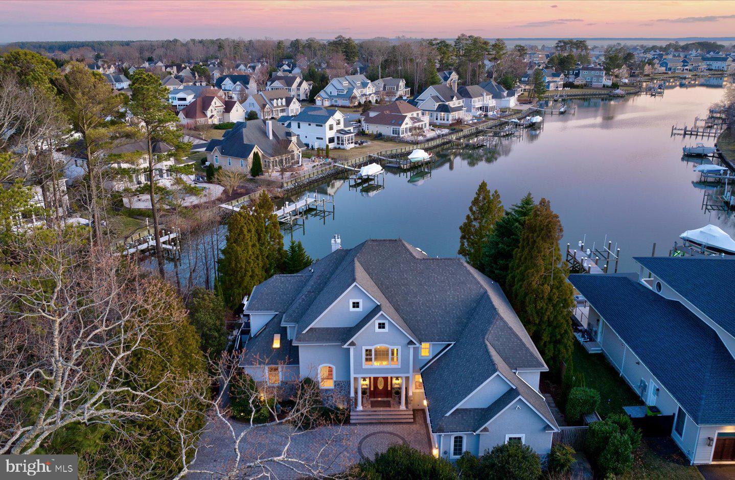 Unparalleled waterfront luxury home with breathtaking views. Nestled along the tranquil shore of the Bald Eagle Lagoon on a high bulkheaded lot, this 5,300 sq. ft. waterfront estate is an extraordinary blend of elegance, comfort, and modern sophistication. Thoughtfully designed to capture unobstructed water views, this stunning residence features 5 spacious bedrooms, 4.5 baths, and multiple indoor and outdoor living spaces, all crafted for the ultimate coastal lifestyle. Upon arrival, you'll be captivated by the hardscape driveway, stone retaining wall, and professionally designed landscaping with accent lighting, setting the stage for the beauty within. Step through the grand 2-story foyer into an inviting living room with a gas fireplace and beautiful water views. Adjacent to this space, the gourmet kitchen is a chef’s delight, featuring granite countertops, 6-burner range, center island, and breakfast area, all open to a cozy family/media room with a second fireplace. Just beyond, a gorgeous sunroom wrapped in glass showcases the tiered landscape grounds and long, serene water views down the lagoon. The first-level primary suite is a private retreat offering a spa-inspired ensuite bath and fireplace, two custom-designed closets, and direct access to the screened porch. The second level boasts 4 additional bedrooms, 2 of which feature ensuite baths with jetted tubs, ensuring ample space and privacy for family and guests. A handsome library doubles as an executive office complete with built-ins, fireplace, and panoramic water views, creating a refined yet functional workspace. Meanwhile, the solarium overlooking the Bald Eagle Lagoon offers a peaceful escape bathed in natural light. The resort-style exterior is designed for relaxation and entertaining. A heated infinity-edge pool, hot tub, and extensive hardscaping create a private oasis while the outdoor kitchen is perfect for al fresco dining. Boating enthusiasts will appreciate the private dock with 2 lifts, offering effortless access to Rehoboth Bay. Additional premium features include a 3-zone HVAC system for customized climate control, a security system for peace of mind, a conditioned crawlspace for enhanced efficiency, and an oversized 2-car garage with ample storage, separate storage/workshop, lightning rods, and generator. Sustainability meets luxury with an owned solar panel system, ensuring energy efficiency. This is more than just a home—it’s a waterfront sanctuary offering luxury, privacy, and an unparalleled connection to nature. Don’t miss this rare opportunity to own a piece of coastal paradise!