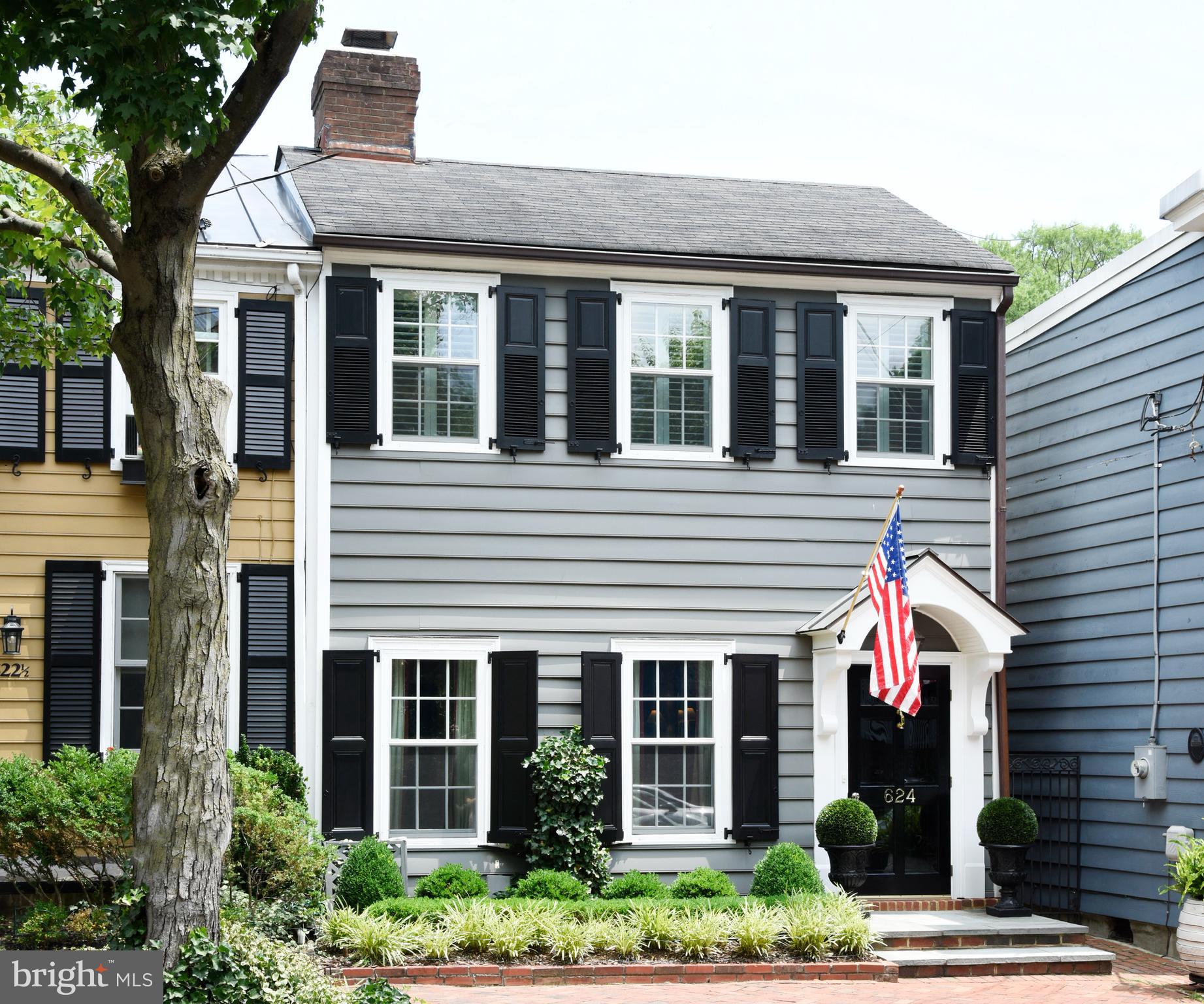 Circa 1875, this semi-detached townhouse offers gracious rooms for entertaining and everyday living, a private outdoor retreat, and one off-street parking space.  The home benefited from Polly Hulfish’s preservation efforts in the 1950s and has been thoughtfully updated and meticulously maintained over the years.
The stylish living room features parquet flooring, crown molding, plantation shutters, and a gas fireplace with a marble surround and ventless gas logs.  The formal dining room offers parquet flooring and crown molding, while a striking chandelier adds warmth and elegance, creating an inviting atmosphere for entertaining.  A conveniently located powder room is finished with herringbone marble tile.
An elegant archway leads to the sun-filled breakfast room, where three skylights with new shades, built-in cabinetry, and abundant storage create a bright, functional space.  Enjoy preparing meals in the adjoining kitchen with cherry cabinetry, brick flooring, and Miele appliances.  Relaxation is effortless in the first-floor family room adjacent to the kitchen.  Anchored by a wood-burning fireplace with new venting, architectural details including decorative paneling and custom bookshelves lend timeless character.
A graceful double staircase with volutes, rake balusters, and a wool runner leads to the upper level.  Handsome matching bell jar light fixtures accent the staircase at both the top and bottom.  A lovely primary suite is a peaceful retreat offering hardwood floors, plantation shutters, and a new Daikin mini-split system.  The en-suite bath includes a seamless glass shower, skylight, and additional storage.  Two generously sized guest bedrooms, one with a custom built-in desk, share a Jack-and-Jill bath with a skylight. 
A delightful surprise, the unique rooftop deck offers a private escape above the Old Town rooftops.  Unwind with a favorite drink as the sun sets, relax in comfort, or enjoy a good book as you slow down and take in the peaceful surroundings.
Savor the outdoors or dine al fresco on the beautifully landscaped patio oasis graced by a pergola, climbing wisteria, gardenia, and lush greenery.  A new brick wall and gate provide access to the off-street parking space for one small car.  Situated on one of Old Town’s most sought-after streets, this historic beauty is just minutes from interesting shops, wonderful restaurants, gourmet food stores, the river, and the Mount Vernon Trail.