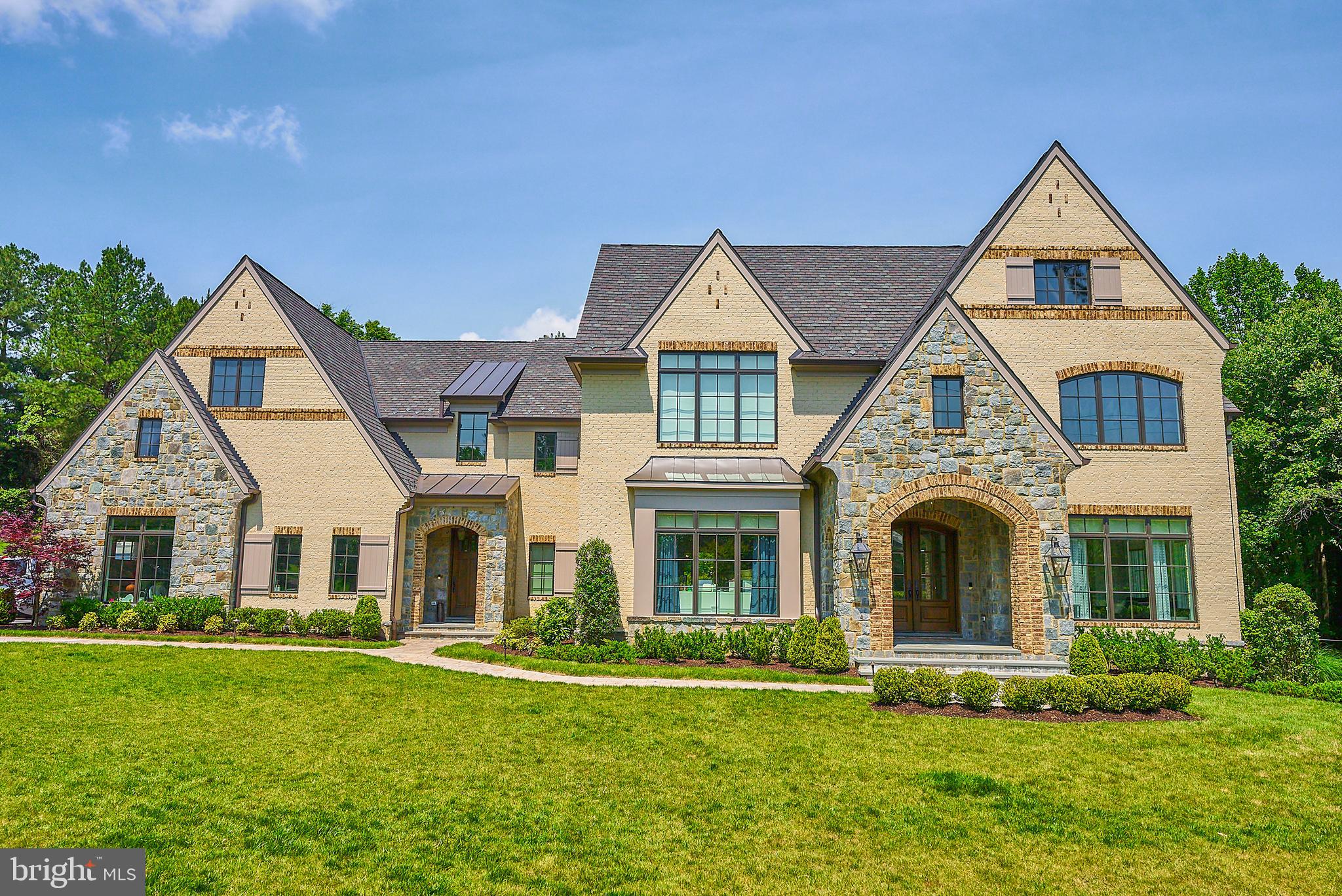 Experience luxury and comfort in this stunning English Manor-style home on over two acres in McLean. Built in 2019 with a stone and brick exterior, this elegant residence is elevator-ready and designed to impress.
From the moment you step through the oversized walnut and glass front doors, you'll notice the exceptional craftsmanship, hardwood floors, intricate millwork, elegant light fixtures, and expansive windows on all three levels. The main floor is warm and inviting, with formal dining and living rooms leading to a more relaxed space featuring a stone masonry fireplace and wood-beamed ceilings.
The professionally designed kitchen is the heart of the home, offering ample cabinet and counter space. Highlights include a large center island with a prep sink, a 48" Thermador gas range with dual ovens, an additional wall oven, built-in microwave, paneled refrigerator and freezer, two paneled dishwashers, and a picturesque window above the sink overlooking the backyard. A herringbone backsplash, custom pantry, and Butler’s Pantry with a beverage cooler complete this culinary masterpiece.
A stately office with 12-foot coffered ceilings, built-ins, and French doors to the rear portico provides a serene workspace. The grand staircase, illuminated by a wall of windows, leads to five spacious bedroom suites, each with a designer bathroom and walk-in closet. The owner’s suite boasts a box ceiling with chandelier, a dressing room with a window seat, two custom walk-in closets, and a spa-like bath with dual vanities, a vessel tub, and a dual-head shower with body sprays.
Convenience is key with two laundry stations, one on the bedroom level and another in the mudroom. The expansive walk-out lower level features a smart media room, guest suite, masonry gas fireplace, wet bar with optional wine room, and a versatile unfinished space for a workshop, gym, or art studio.
Outside, enjoy a covered verandah, deck, paver patio, firepit station, and an obstacle course, making this home a true entertainer's dream. The private lot easily accommodates a pool, detached garage and many other future enhancements. A perfect blend of elegance and functionality, this home is designed for refined living and lasting memories.