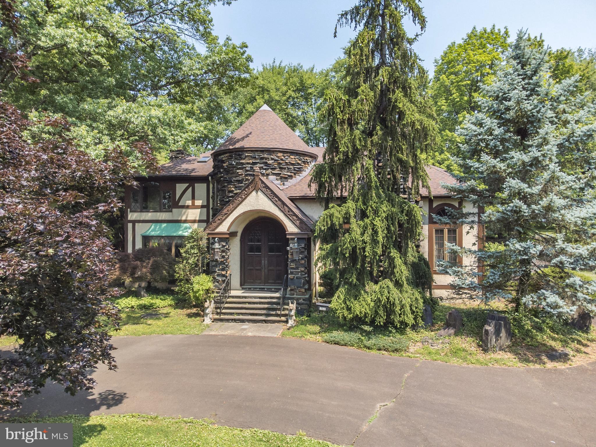 European, old-world elegance abounds in this custom-built Tudor-style home, situated along the 8th hole of Whitemarsh Valley Country Club. It features a turret, a circular driveway, an exquisite backyard with an in-ground pool, two staircases, an abundance of storage, and a myriad of unique architectural characteristics. Upon entering through impressive antique Cathedral double doors, you are welcomed into the turret - a grand foyer filled with natural light. Your eye is immediately drawn to the 27ft ceiling –bordered with intricately hand-crafted inlaid wood. The focal point is the curved wrought-iron-railed staircase, ascending to the second level. From the foyer, step down into the formal living room, boasting a soaring trestle wood ceiling. The original teak hardwood floors in a herringbone pattern are in pristine condition. The centerpiece of this room is the magnificent wood-burning fireplace. Reminiscent of a medieval  castle, the massive hearth is encased with an elaborately sculpted 8ft tall stone mantle, complete with a Coat of Arms. The teak herringbone-patterned floors continue into the formal dining room, illuminated by a wall of windows. The spacious eat-in kitchen flows from the dining room and has a brick wood-burning fireplace, custom cabinets, and a splendid view of the backyard. A hallway connected to the kitchen contains the back stairs leading to the second level and is flanked by a good-sized laundry room, a full bath, and storage closets. Access to the garage is located off this hallway. Adjacent to the kitchen is a capacious bi-level family room with a wet bar, gas fireplace, and backlit stained-glass inlays above the bar. Step outside through the sliding doors into a secluded haven. The in-ground pool is surrounded by a flagstone patio and is hedged with a distinctive stone wall with a built-in water fountain. A few steps up from the pool area sits a sweeping manicured lawn, overlooking the golf course. The second level highlights four bedrooms, three full baths, and two cedar closets. The primary en-suite is striking, with a wood-burning fireplace, a separate walk-in dressing room, and a 4-piece tiled bath which includes a jetted tub. The second bedroom has a tiled, 4-piece private bath. The third and fourth bedrooms are large with plenty of closet space and share a hall bath. A walk-up attic is located on the third floor, yielding a wealth of storage. The immense basement is a blank canvas, with outside access. It contains a powder room and a plethora of storage space. This enchanting property leaves an indelible impression and yearns for your personal touch with some TLC. Conveniently located to shopping, restaurants, center city Philadelphia, and all major highways. Schedule a tour today. Don’t miss an opportunity to make this house your ultimate dream home!