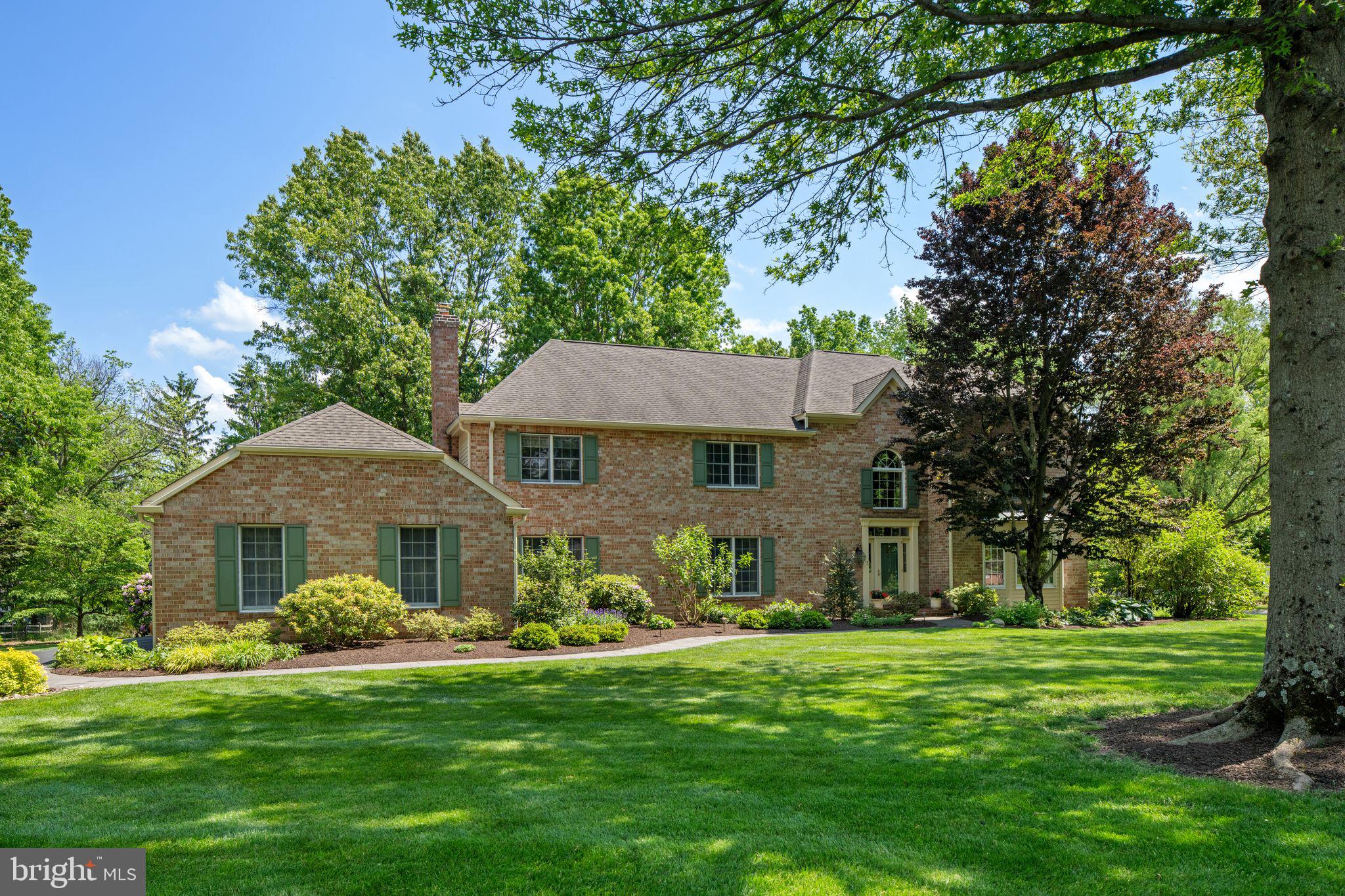 Nestled along one of the most sought-after streets in the coveted Pebble Hill neighborhood of Doylestown, this grand brick home with a three-car garage is an exceptional offering in the heart of Bucks County. Surrounded by mature trees and thoughtfully designed landscaping, the property offers an elegant, park-like setting within a vibrant peaceful neighborhood where neighbors stroll tree-lined streets just moments from the charm of Doylestown Borough. Step through the front door into a soaring two-story foyer where crisp, classic, and a refined  design and timeless sophistication immediately set the tone. Pristine hardwood floors flow throughout the home, creating warmth and character. To the right, the formal living room features generous proportions and a dramatic picture window overlooking the manicured lawn. Straight ahead, the spacious dining room celebrates indoor-outdoor living with French doors overlooking the deck, creating a seamless transition for entertaining and al fresco dining. Adjacent to the dining room, a stately professional office with glass-paneled pocket doors provides privacy and function, featuring custom built-ins and a ceiling fan, an ideal retreat for today’s work-from-home lifestyle. A discreet powder room and multiple storage closets complete the main level. The well-appointed kitchen is both beautiful and highly functional, showcasing custom maple cabinetry with rollout drawers, high-end stainless-steel appliances including a warming oven, and a generous center island for gathering and preparation. An undermount sink, recessed and under-cabinet lighting, and authentic Mercer tiles celebrating the four seasons lend timeless Bucks County character. A spacious eat-in area makes everyday meals feel special.  Continue to the conveniently located main floor laundry area and full bath for added convenience. French doors lead to the breathtaking heated sunroom, an idyllic retreat that blurs the line between indoors and out. Surrounded by windows, accented by skylights and ceiling fans, and overlooking private, meticulously maintained gardens, this space captures the very essence of Bucks County living year-round. The adjoining family room is equally inviting, featuring exposed wood beams, wood-paneled pocket doors, a wood-burning fireplace, and enlarged windows that bathe the space in natural light. Designed for both cozy evenings and lively gatherings, it is truly the heart of the home. Upstairs, the thoughtfully designed second level balances luxury and livability. The primary suite serves as a private sanctuary with two custom walk-in closets and an updated en suite bath featuring a double vanity, soaking tub, glass-enclosed shower, private lavatory room with bidet, and linen closet. The second bedroom is generously sized with two closets, while the third bedroom presents as a princess suite with its own private full bath. The fourth bedroom offers a custom walk-in closet with shelving and drawers. A neutral hall bath with double sinks and an additional linen closet serves the remaining bedrooms. All bedrooms feature newer carpeting. The partially finished basement is spotlessly clean, dry, and bright with high ceilings, offering exceptional flexibility for a home gym, recreation room, studio, or media space. Outside, mature trees, lush landscaping, and exceptional privacy create a serene backdrop to this remarkable property. Ideally located near Doylestown’s boutiques and dining, as well as the Mercer Museum and Doylestown Hospital, the home pairs timeless beauty with modern practicality. Additional upgrades include a roof with gutter guards (2013), hot water heater (2022), water softener system, and two-zone heating and air conditioning. Schedule your private showing today!