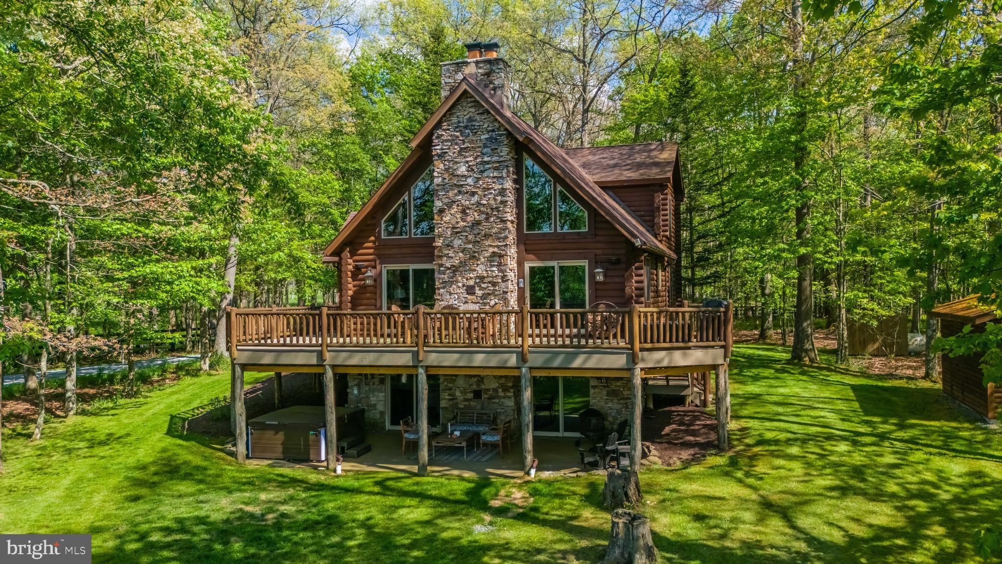 Some properties are simply built differently in every sense of the phrase. Set on nearly four private, wooded acres in the coveted southern end of Deep Creek Lake, 125 Ruta Lane is a custom Yellowstone log home that delivers the kind of craftsmanship, character, and setting that the lake area rarely sees come to market.

From the moment you arrive, the architecture commands attention. Yellowstone's signature oversized solid round logs give the home a presence that no modern construction can replicate, and the dry-stack fieldstone chimney rising through all three levels is a testament to a masonry artform that has all but vanished from today's building landscape, replaced elsewhere by faux composites, but preserved here in its full, labor-intensive glory.

Inside, the great room sets the tone for everything that follows. A floor-to-ceiling signature tree column anchors the space beneath soaring cathedral ceilings and hand-hewn log beams, while a dry-stack stone fireplace serves as the room's natural focal point. The open floor plan flows seamlessly from the renovated gourmet kitchen, featuring a dramatic granite island, stainless KitchenAid appliances, and custom knotty cherry cabinetry, through the dining area and out to the expansive deck, where wooded privacy gives way to lovely lake views that remind you exactly where you are.

Four bedrooms are spread thoughtfully across three levels, including the main level primary suite with an updated en-suite bath. The loft level adds two additional bedrooms, a full bath, and a cozy sitting area overlooking the great room below. The fully finished lower level, wrapped in authentic Tennessee barnwood, offers a fourth bedroom, a third full bath, a bar area, and walkout access to the newly covered patio, where a new hot tub, stacked native stone walls, and a fire pit create an outdoor living space worthy of the setting.
And then there is the lake. Two assigned DNR-permitted dock slips on a quiet, private cove are included with this sale, a distinction that genuinely sets this property apart, as two-slip access at this price point is rare at Deep Creek. A level, well-maintained path connects the property to the water, where boating, kayaking, swimming, and summer evenings on the dock await.

The nearly four acres, comprising two wooded lots conveying together, deliver a sense of seclusion and privacy that feels a world away, while still being just minutes from everything the lake area has to offer. Roof 2019. HVAC 2020. Septic pumped October 2025. Comcast broadband. Completely turn-key and ready for its next chapter.

4 BD | 3 BA | 2,624 Fin. Sq Ft |  4 Acres | 2 Dock Slips | Deep Creek Lake Access | Ardsley Farms HOA