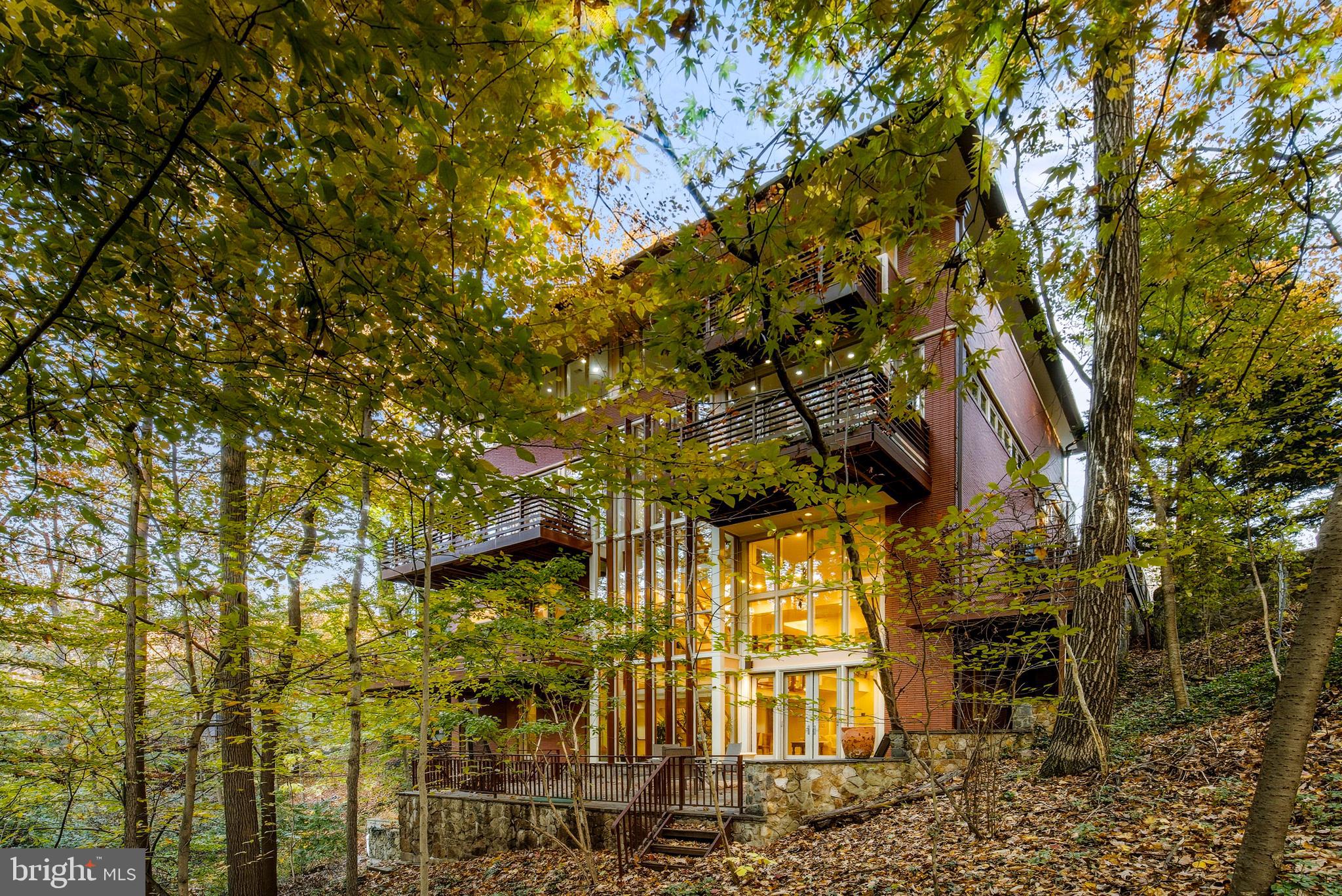 Now positioned at $3,995,000 - one of the best values in NW DC!! New HRLS photos and video forthcoming.  

This masterfully designed residence at the quiet end of a cul-de-sac bordering Rock Creek Park appears to emerge from the landscape itself. From the front approach, its restrained roofline, horizontal brickwork, and natural materials convey a calm order, an urban reflection of the organic principles advanced by Frank Lloyd Wright, and it features an elevator to all levels. The home feels timeless and assured, grounded in Washington’s built tradition yet oriented to the forest beyond.

At the rear, the façade becomes a masterclass in the fusion of dwelling and wooded landscape. Expanses of glass and carefully scaled terraces dissolve the boundary between structure and setting, allowing nature to animate the interior throughout the day.

Inside, the design by Travis Price, FAIA unfolds as a study in movement and light. A double-height great room anchors the plan, framed by floating landings and structural glass that draw natural light through every level. The arrangement creates a seamless progression from open gathering spaces to quieter moments of retreat, each revealing a distinct relationship to the wooded setting. Rooms adapt in purpose and scale, including a study or studio, a guest suite, a den that opens to a terrace, or a lower level designed for wellness and work.

Throughout, materials remain honest and enduring, with brick, glass, steel, and wood in balanced proportion. Every element serves the experience of living within the space rather than beside it.

The result is a home of enduring calm and presence, modern in spirit, profoundly connected to nature, and perfectly situated along one of the city’s most treasured park-front settings.