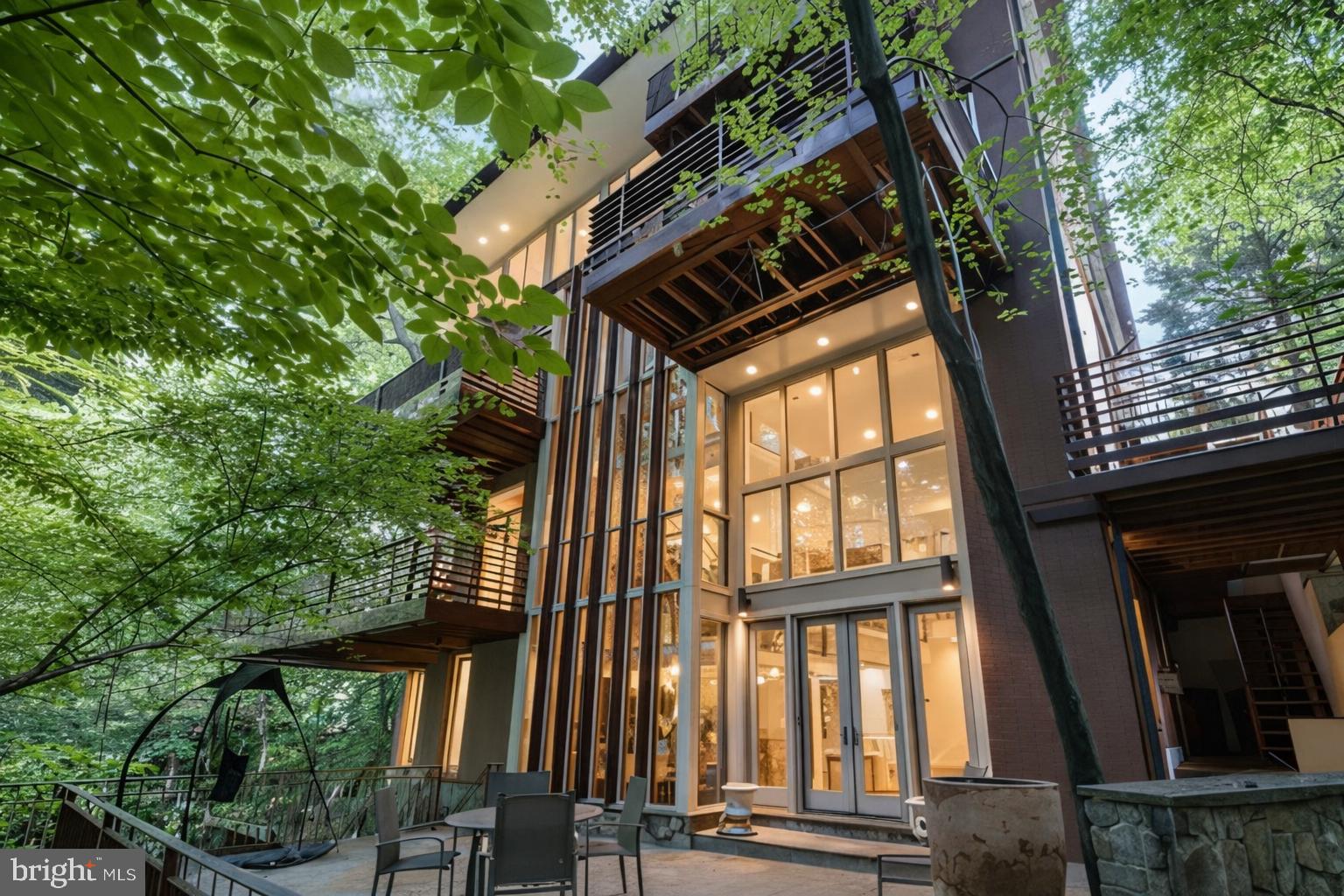 OPEN SUNDAY [6/07] from 1pm to 3pm   Now positioned at $3,995,000, this masterfully designed residence at the quiet end of a cul-de-sac bordering Rock Creek Park appears to emerge from the landscape itself. From the front approach, its restrained roofline, horizontal brickwork, and natural materials convey a calm order, an urban reflection of the organic principles advanced by Frank Lloyd Wright, and it features an elevator to all levels. The home feels timeless and assured, grounded in Washington’s built tradition yet oriented to the forest beyond.

At the rear, the façade becomes a masterclass in the fusion of dwelling and wooded landscape. Expanses of glass and carefully scaled terraces dissolve the boundary between structure and setting, allowing nature to animate the interior throughout the day.

Inside, the design by Travis Price, FAIA unfolds as a study in movement and light. A double-height great room anchors the plan, framed by floating landings and structural glass that draw natural light through every level. The arrangement creates a seamless progression from open gathering spaces to quieter moments of retreat, each revealing a distinct relationship to the wooded setting. Rooms adapt in purpose and scale, including a study or studio, a guest suite, a den that opens to a terrace, or a lower level designed for wellness and work.

Throughout, materials remain honest and enduring, with brick, glass, steel, and wood in balanced proportion. Every element serves the experience of living within the space rather than beside it.

The result is a home of enduring calm and presence, modern in spirit, profoundly connected to nature, and perfectly situated along one of the city’s most treasured park-front settings.