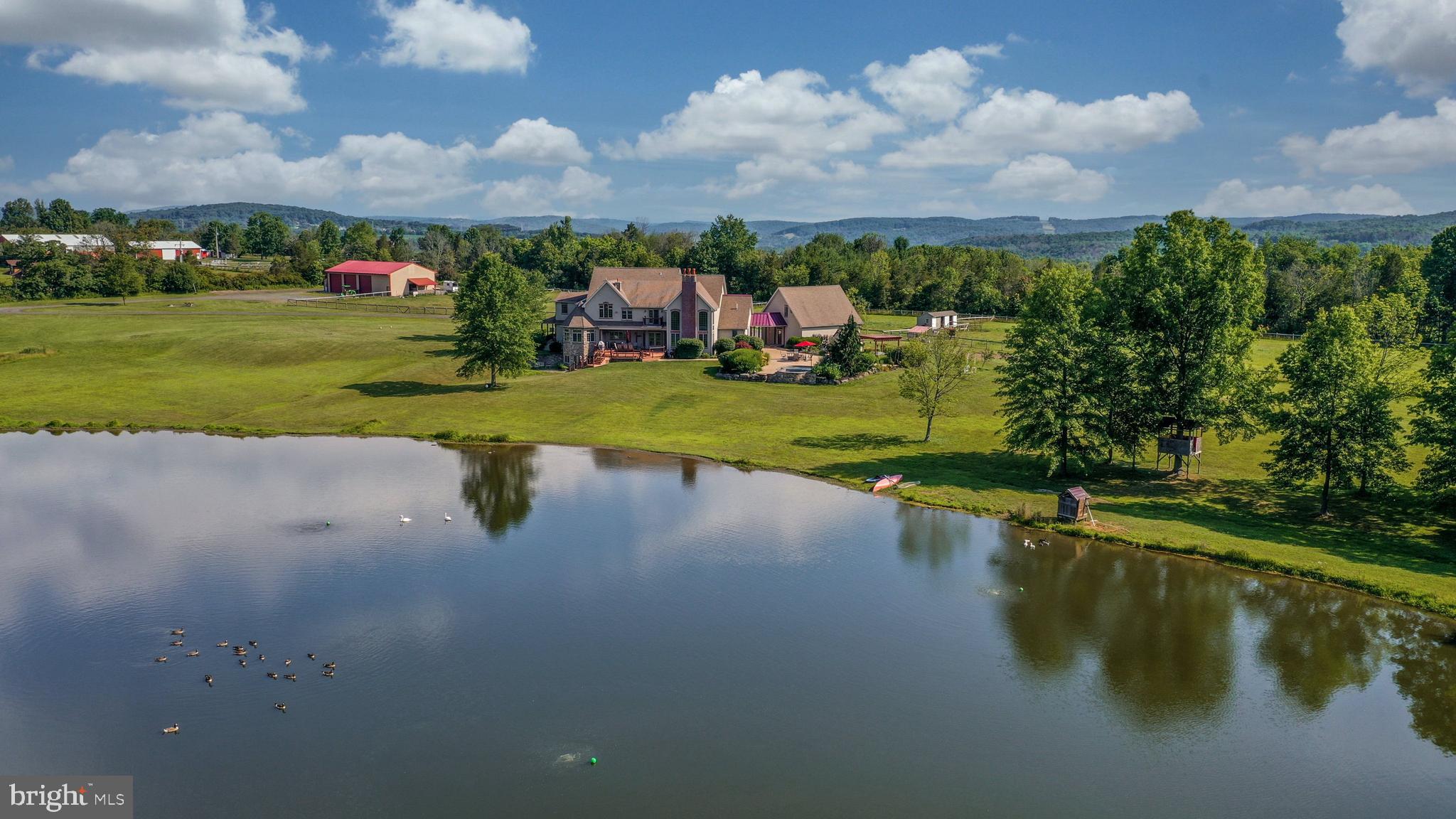 Purchase this stunning farmhouse along with two additional building lots for a total of 42.25 acres in beautiful Upper Bucks County. The house parcel includes a 3-acre pond, fenced pastures, & multiple outbuildings. 

Entry to the 6,800 square foot home begins with a 2-story stone entry and large wrap-around porch. Radiant heat floors run throughout the main level, under Brazilian cherry and brick tile flooring. A gas fireplace in the living room is flanked by bookcases, while the nearby game room is flexible space suited for a multitude of uses. A butler's pantry and sunroom complement the oversized kitchen, with brick tile floors and cherry cabinetry. Granite countertops, newer appliances and a gas cooktop are perfect for gatherings of all sizes, and the breakfast area opens to a large deck looking out over the pond. The adjacent family room with vaulted ceiling offers a wet bar and wood-burning fireplace. Office space, laundry/mud room, a full bath and powder room round out this floor. Newly installed carpeting runs throughout the second floor. The primary suite is luxurious with a private balcony and double sided gas fireplace leading to the en suite bath with radiant heat floor, double sinks and jacuzzi tub. A second suite is found on this floor, along with two large bedrooms connected by a jack-and-jill bath, and a second laundry room. The walkout lower level has high ceilings and lots of potential for additional living space. 

Outdoor amenities include a 3-car garage with 2nd floor storage space. Concrete patios lead to the in-ground pool with waterfall and hot tub. A large barn features custom studio space and a powder room, along with ample storage. A small stable includes two run-in stalls and a tack room. Outlying Acres is located in the Palisades School District and is close to shopping, dining and commuter routes. The vacant lot has Bucks County Horse Park trails on it.