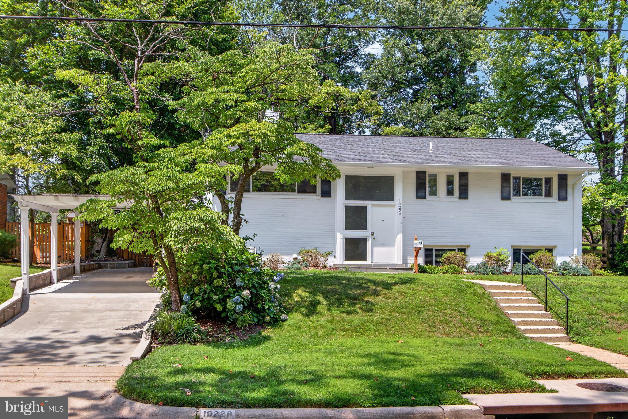 Location, space, and timeless character come together at 10228 Hatherleigh Drive in Wildwood Manor, one of Bethesda’s most desirable neighborhoods. Built in 1957, this classic all-brick split-foyer home is beautifully positioned beneath mature trees and surrounded by lush landscaping.

The light-filled main level features hardwood floors, recessed lighting, a spacious living room, and a dining room lined with oversized windows. The updated kitchen offers granite countertops, stainless steel appliances, generous cabinetry, and convenient access to the outdoors. Three bedrooms and two full bathrooms, including a primary en suite, complete this level.

Downstairs, the fully finished walkout lower level expands the home’s versatility with a large recreation room anchored by a wood-burning fireplace, a fourth bedroom, a full bathroom, and a dedicated laundry room. The flexible layout is ideal for guests, a home office, fitness space, or additional recreation.

Outside, an expansive patio overlooks the beautifully landscaped, fully fenced backyard, creating a private setting for outdoor dining, entertaining, gardening, or quiet relaxation. An attached carport, concrete driveway, and storage shed add everyday convenience.

All of this is just blocks from Wildwood Shopping Center and close to neighborhood parks, community recreation, bus routes, and the Red Line Metro. A wonderfully maintained home offering comfort, flexibility, and an exceptional Bethesda location.