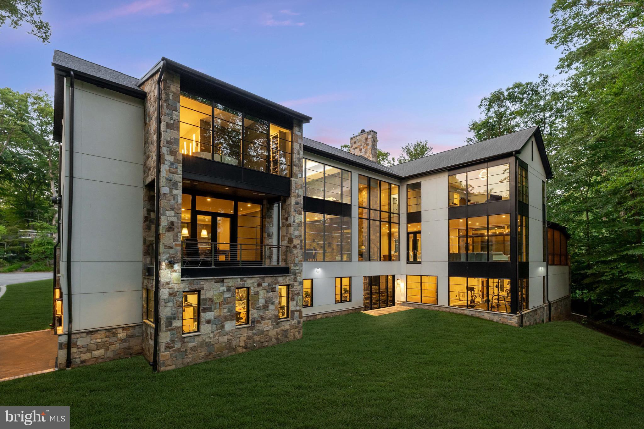 Tucked away, just off the convenience of Massachusetts Avenue, lies idyllic Bay Tree Lane, adorned by lovely homes on large lots and under the canopy of gorgeous mature trees. Perfectly positioned on the best lot of the quiet cul-de-sac, is the stunning contemporary estate of 3 Bay Tree Lane. Constructed in 2018, this 12,700 square foot masterpiece stands at the epitome of cutting-edge design and masterful craftsmanship. The distinctive facade is clad in an effortless combination of natural stone, mahogany, stucco, and lit by swirling gas lanterns, a combination that make this home feel like it could just as easily be mountainside at an exclusive ski resort. 

Arranged in an L-shape, the home is approached by two separate driveways leading to an upper three-car and lower two-car garage for the automobile enthusiast. The arrival parking pad is generous in scale and provides a grand, flagstone approach to the main entrance. An oversized mahogany door pivots open to reveal the grand foyer. Effectively a glass section bridging two separate masses, the feeling is as if you are standing in the surrounding nature of the home. The double-height entryway is flooded with natural light on both sides via floor to ceiling windows with motorized blinds, illuminating the 8-inch quarter-sawn white oak floors. A functional work of art, the floating staircase is framed with tempered glass and stainless steel. 

Opposite is a towering two-sided stone fireplace, through which is the expansive living room. Gracious in scale, the space is surrounded by wooded views and fully opens onto an oversized screened-in porch for seamless indoor/outdoor living. Amenity rich with a pizza oven, wood-burning fireplace, grilling station, and custom wooden ceiling complemented by an iron chandelier forged in Aspen’s Roaring Fork Valley, it is an ideal place for al fresco entertaining. Also adjacent is the outstanding chef’s kitchen. 

A true showstopper, custom cabinetry, an inlaid modern marble backsplash, and skylights illuminating exposed beams in the vaulted ceiling overhead set the tone for a space which is luxurious yet exceptionally functional. A custom stainless steel range hood and an illuminated glass backboard on one of the two mitered-edge, 10 ½-foot Blanco quartz islands serve as statement pieces, while a fully redundant suite of Miele, SubZero, and Wolf appliances, including a Wolf steam oven as the third oven, represent the top-of-the-line in equipment. 

The dramatic formal dining room features floor-to-ceiling wooded views, a porcelain stacked stone feature wall, and marble serving station. No need to descend to the lower level, this home offers a dignified post-dinner retreat in its unique main level billiard room lounge. The bar is fully equipped with a Miele and SubZero appliance suite, while a striking Da Vinci gas fireplace with integrated lighting and a textured, tufted surround inject warmth into the space. Double glass doors provide private terrace access. 

With soaring 11 foot ceilings throughout, an office with a custom fabricated door composed of resin and wood sliding seamlessly on a Sun Valley Bronze polished nickel frame and a generous mudroom, each with custom Sroka built-ins complete the main level.