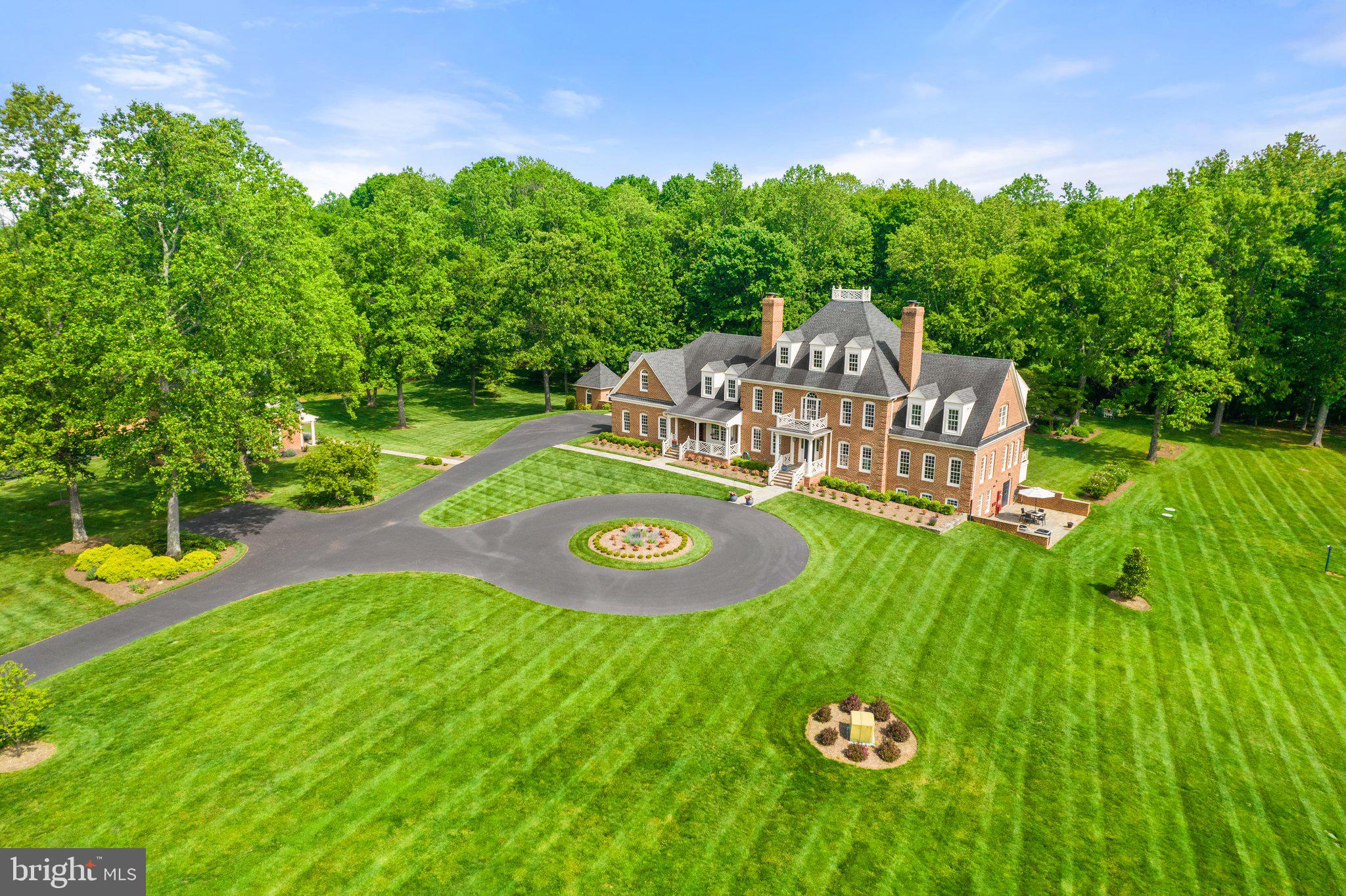 Flent Hall, a stunning Colonial Williamsburg-inspired home, originally built in 1990, has been lovingly remodeled inside and out during the past four years.  Situated on 20 manicured acres in the Old Dominion Hounds hunt country and in an area of numerous protective conservation easements, this all-brick wonderful country house is immaculate in its many luxurious offerings. One enters the two-story reception hall featuring a grand staircase. From there, one finds the 22x23 great room with floor to ceiling stone, woodburning fireplace, numerous sun-burst windows, and access to the rear porch. Off to the left is the open, fully-fitted and recently remodeled 17x31 kitchen with lots of table space, Italian Fulgor Milano appliances, Kraftmaid cabinetry, marble and quartzite counters, Blanco sinks and Brizo faucets, two kitchen islands and a woodburning fireplace. Nearby is the 16x17 dining room, 35x14 family room with French doors to the porch, the cozy library with woodburning fireplace and a powder room. There is a full bath off the kitchen that also serves the pool. Up the grand staircase (there is also a back staircase that comes down to the kitchen) one finds the 20x26 primary bedroom, 3 walk-in closets, lots of windows taking in the view, a woodburning fireplace and an exceptional bath with two hammered nickel sinks, bidet, copper tub with hammered nickel finish and large shower. There is an upstairs reading room with fireplace and four additional bedrooms. On the lower level there is a full bath, bedroom with walk-in closet and lots of windows, 21x21 recreation room with fireplace, an exercise room and two large storage rooms. 
The well-appointed house features all new Jeld-Wen double paned windows, 6-woodburning fireplaces, solid wood doors throughout, 3 ½ inch gleaming oak floors, particularly fine bathrooms, total garaging for four cars, all brick and Hardiplank construction – all maintained on a very high order. 
The brick guest house offers completely redecorated quarters with full bath, woodburning fireplace and a new heat pump. There is a 2-stall brick stable with tack room, hay loft, an attached run-in and chicken coop, and two paddocks. 
The home is enhanced by the immense character of the grounds including a long, paved drive approach to a circular front parking forecourt, exterior lighting on the house and garden, a lion’s head fountain into a garden pond, brick potting shed, all new stone patios and sidewalks, a 46-foot pool with new gunnite, coping and tile, a 80-head sprinkler system – all bathed in bursting flower gardens and shrubs – the base structure of the garden having been designed by Caroline Tait, a Royal Horticulture Society (RHS) Hampton Court, Palace Garden Festival award winner. 
To take in the splendid rural setting, perhaps your favorite spot might be relaxing on the 21x22 resort-like covered rear porch overlooking pastures, pool, gardens and woodland. It features delightful Chippendale railings and Ipe decking – truly a first-class setting.  9.9 miles via Crest Hill Rd. to Rte. 66 at Marshall.