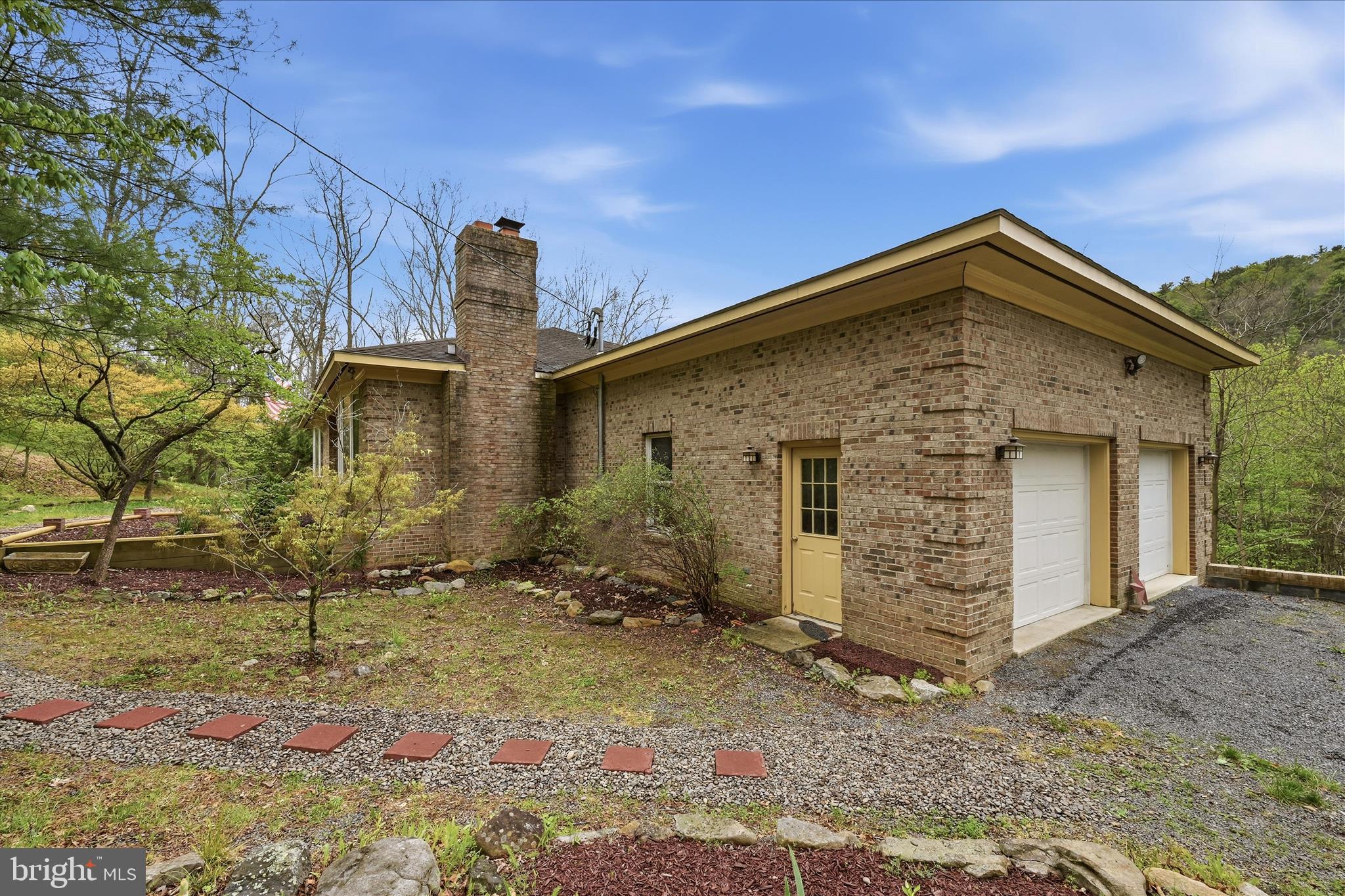 Private mountain living with real-world convenience. As the current owners and full-time healthcare professionals who personally commute to Winchester 4 days a week, this location has proven to offer both the peace and privacy buyers dream about—without sacrificing everyday practicality. Set on 5 private acres with creek frontage, this all-brick 4,100+ sq ft. retreat (finished and unfinished bonus space) offers space, flexibility, and a lifestyle the current owners have truly loved. The main level features an open-concept kitchen with real wood cabinetry, a center island for added storage, and a walk-in pantry. Hardwood flooring extends from the kitchen into the living room and across much of the main level. A wood stove, stacked stone fireplace, and light-filled bay window create a warm and inviting gathering space, while custom masonry details add character throughout the home.
The primary suite offers generous space, highlighted by a bay window, two walk-in closets, and an updated bath with a jetted tub. A private entrance from the suite leads to a screened deck overlooking the natural, mountainous backyard. The expansive rear deck provides additional space for outdoor entertaining. A secondary main-level bedroom includes a bay window, two walk-in closets, and its own bathroom suite.
The mostly finished lower level offers flexible living options, including a bedroom suite with built-ins, two closets, and a connected bath. A bonus room with a walk-in closet provides additional space for guests or office use. The lower level also features a large recreation room with a pool table, a second living area with a brick fireplace, and multiple storage spaces, including a shelved root cellar. Laundry hookups and two separate entrances add convenience and functionality.
Outdoor features include access to the creek, suitable for fishing, hunting, or enjoying the natural setting. A chicken coop and a multi-use shed are also on the property. The HVAC system has been replaced within the past two years. The attached two-car garage includes a 30-amp outlet for a generator, which conveys, or for other purposes, such as an RV or an electric car. 
Community amenities include a swimming lake, tennis courts, and a clubhouse. There are no HOA restrictions, and a yearly fee covers road maintenance and snow removal.