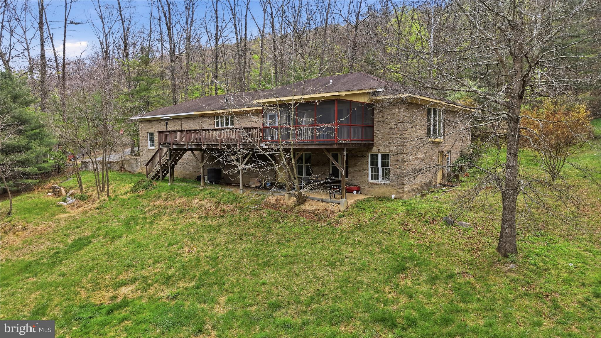 Private mountain living with real-world convenience. As the current owners and full-time healthcare professionals who personally commute to Winchester 4 days a week, this location has proven to offer both the peace and privacy buyers dream about—without sacrificing everyday practicality. Set on 5 private acres with creek frontage, this all-brick 4,100+ sq ft. retreat (finished and unfinished bonus space) offers space, flexibility, and a lifestyle the current owners have truly loved. The main level features an open-concept kitchen with real wood cabinetry, a center island for added storage, and a walk-in pantry. Hardwood flooring extends from the kitchen into the living room and across much of the main level. A wood stove, stacked stone fireplace, and light-filled bay window create a warm and inviting gathering space, while custom masonry details add character throughout the home.
The primary suite offers generous space, highlighted by a bay window, two walk-in closets, and an updated bath with a jetted tub. A private entrance from the suite leads to a screened deck overlooking the natural, mountainous backyard. The expansive rear deck provides additional space for outdoor entertaining. A secondary main-level bedroom includes a bay window, two walk-in closets, and its own bathroom suite.
The mostly finished lower level offers flexible living options, including a bedroom suite with built-ins, two closets, and a connected bath. A bonus room with a walk-in closet provides additional space for guests or office use. The lower level also features a large recreation room with a pool table, a second living area with a brick fireplace, and multiple storage spaces, including a shelved root cellar. Laundry hookups and two separate entrances add convenience and functionality.
Outdoor features include access to the creek, suitable for fishing, hunting, or enjoying the natural setting. A chicken coop and a multi-use shed are also on the property. The HVAC system has been replaced within the past two years. The attached two-car garage includes a 30-amp outlet for a generator, which conveys, or for other purposes, such as an RV or an electric car. 
Community amenities include a swimming lake, tennis courts, and a clubhouse. There are no HOA restrictions, and a yearly fee covers road maintenance and snow removal.