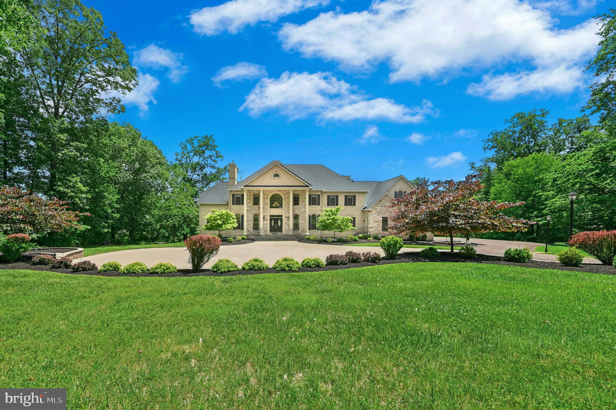 Set against the backdrop of Jericho Mountain and neighboring the prestigious Jericho National Golf Club, this extraordinary estate is tucked within one of Upper Makefield Township's most exclusive enclaves of custom homes. Privately positioned on 5.9 pristine acres, the property combines grand-scale living with the tranquility of a park-like setting framed by mature trees and partially wooded grounds.
A stately entrance marked by stone pillars, brick walls, and a winding drive creates a memorable arrival experience. The drive culminates in an impressive motor court offering abundant guest parking and access to the four-car garage with extra-height doors.
Designed for both elegant entertaining and comfortable everyday living, this 8,058-square-foot residence offers four levels of thoughtfully crafted living space with 8 bedrooms, 7 full baths, and 2 half baths. Rich architectural details include extensive custom millwork, five fireplaces, gleaming hardwood floors with decorative inlays, a dramatic curved staircase with iron balusters, and walls of windows that fill the home with natural light.
A grand two-story foyer introduces the home's sophisticated interior, where sightlines extend through the residence to a spectacular rear wall of glass overlooking the grounds. Formal living and dining rooms provide elegant gathering spaces, while the expansive family room is anchored by a floor-to-ceiling stone fireplace and opens seamlessly to the outdoor living areas.
At the heart of the home is a chef's kitchen designed to accommodate everything from intimate family meals to large-scale entertaining. Professional-grade appliances include a Sub-Zero refrigerator, Thermador Professional range with custom hood, additional cooktop, wall oven, and extensive solid-surface workspaces with dual sinks. A lighted tray ceiling adds warmth and character, while an adjoining catering kitchen and walk-in pantry—with an additional range and sink—make hosting effortless.
A composite deck spanning the rear of the home extends the living space outdoors and provides a picturesque setting for dining, entertaining, or simply enjoying the peaceful surroundings.
The main level also includes a private study with fireplace, a guest suite with full bath, a spacious laundry room, mudroom, and a versatile bonus room with built-in desk, storage bench, and Dutch doors—ideal as a playroom, creative studio, or second home office.
The second level is highlighted by an exceptional owner's retreat featuring a private sitting room separated from the sleeping quarters by a two-sided fireplace, a private den, two oversized walk-in closets, a cedar closet, and a luxurious spa-inspired bath with dual vanities, soaking tub, private water closet with bidet, and a multi-head shower system with body sprays.
Three additional bedroom suites on this level each offer walk-in closets, custom built-ins, and beautifully appointed en-suite baths.
The third floor provides remarkable flexibility with two additional bedrooms, a shared bath, and substantial walk-in attic storage.
The finished walk-out lower level is designed for recreation and entertaining. Highlights include a full bar with wine storage and beverage refrigeration, a gathering room with fireplace, space for a home theater or billiards area, fitness room, additional bedroom, and full bath. Glass doors open directly to a paver patio and the rear grounds.
With two laundry rooms, extensive storage, seller-owned solar panels, propane heat, and a floor plan ideally suited for multi-generational living, this exceptional Bucks County estate offers a rare combination of luxury, privacy, and versatility just minutes from New Hope, Newtown, Washington Crossing, and the cultural attractions of the Delaware River towns.