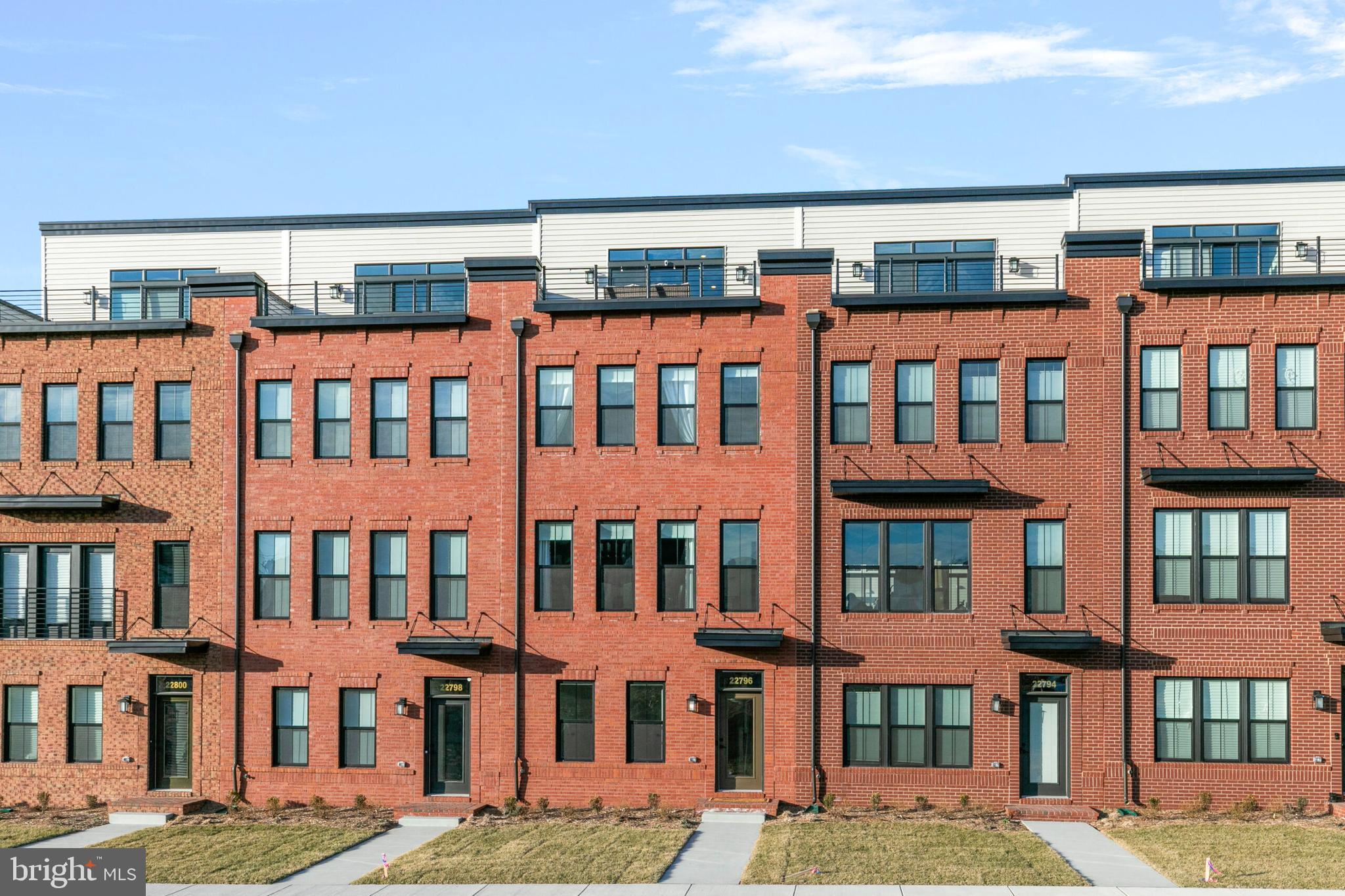 Why wait for a new build when this stunning, newly constructed townhome in Downtown Brambleton is ready to be yours now? Offering four levels of thoughtfully designed living space, this brick-front two-car garage townhome blends modern elegance with everyday functionality—all in an unbeatable location.

Step inside to a welcoming foyer that leads to a versatile entry-level suite, complete with a full bath. Whether you need a private guest retreat, a home office, or a personal gym, this space adapts to fit your lifestyle. Pre-wired ceiling fan connections in this room, as well as the living room, primary suite, second bedroom, and upper-level bedroom, ensure year-round comfort.

The heart of the home is the expansive main level, where an open-concept design creates a seamless flow between the dining area, chef’s kitchen, and inviting family room. The kitchen is a true centerpiece, featuring an oversized island with seating for four, sleek granite countertops, stainless steel appliances, and a gas oven/range. The warmth of wood-style LVP flooring extends throughout, complementing the gas fireplace in the family room. Step out onto the private deck—perfect for morning coffee or evening relaxation.

Upstairs, the primary suite is a private sanctuary with two walk-in closets and a spa-like en-suite bath with a dual-sink vanity and a walk-in shower. A second spacious bedroom, a well-appointed full bath, and a conveniently located laundry room complete this level.

The top floor offers a fourth bedroom, another full bath, and an open loft space ideal for entertaining or unwinding. From here, step out onto the expansive rooftop terrace—a rare feature that provides a private outdoor retreat with sweeping views.

Built with safety and peace of mind in mind, this home is equipped with an automatic fire suppression system on all levels.

Living in Brambleton means access to an unparalleled lifestyle. Enjoy a network of walking and biking trails, multiple pools, sports courts, scenic ponds, and vibrant playgrounds. Just moments away, Brambleton Town Center offers shopping, dining, a movie theater, and coffee shops. Hal and Berni Hanson Park is nearby, as are major commuter routes (Route 7, Dulles Toll Road) and Dulles International Airport.

Move-in ready and brimming with high-end features, this exceptional townhome is ready to welcome you home!