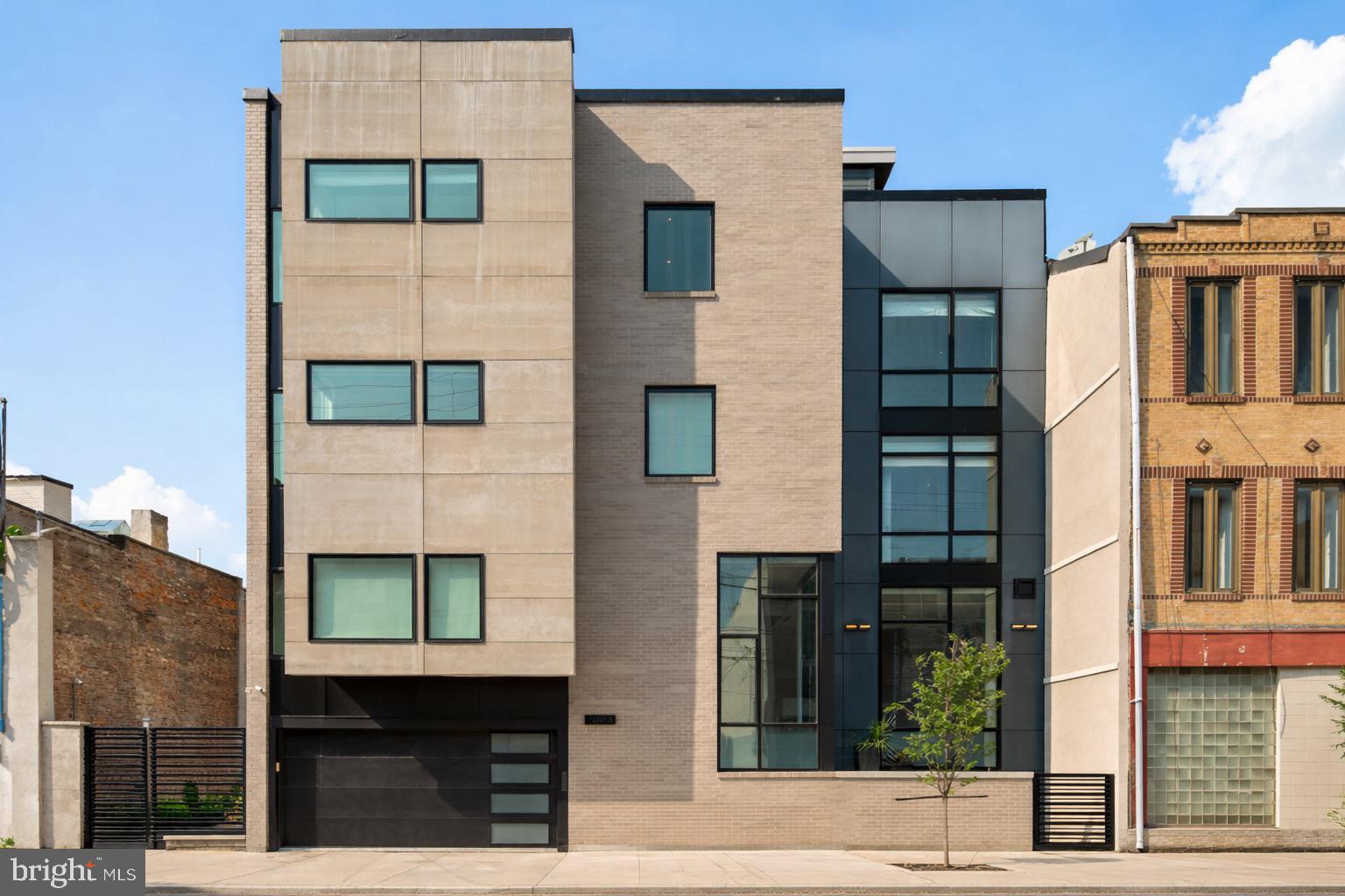 Elevated city living in the heart of Queen Village, where striking design, modern technology, and everyday comfort converge in this exceptional, extra-wide residence. Spanning approximately 4,200 square feet, this five-bedroom, five-bath home offers a rare combination of scale, privacy, and thoughtful craftsmanship—all complemented by a private two-car garage with an electric vehicle charger and a six-stop elevator servicing every level.

A dramatic entry sets the tone, opening into a light-filled living space with soaring ceilings and expansive floor-to-ceiling windows. The home’s contemporary architecture is on full display, anchored by a sleek fireplace and a sculptural floating staircase that wraps seamlessly around the elevator. 

Just a half-level above, the dining area overlooks the main living space, creating a striking, open connection between levels. The adjacent chef’s kitchen is designed to impress—wrapped in marble and outfitted with a premium appliance suite including Wolf, Sub-Zero, and Miele—perfectly suited for both everyday living and entertaining.

Upstairs, a well-designed level features a flexible bedroom or office, a full hallway bathroom, and the primary suite. The primary bedroom offers a serene retreat with a custom walk-in closet and a spa-inspired bath featuring radiant heated flooring, a dual vanity, jetted soaking tub, and a fully appointed steam shower designed for total relaxation.

Continuing to the next level, you’ll find three additional bedrooms, including one with its own ensuite bath, along with a full hallway bathroom and a conveniently located laundry room.

At the top, a fully equipped wet bar—featuring a sink, Miele dishwasher, and Electrolux beverage refrigerator—leads to an expansive private rooftop deck with sweeping views of the Philadelphia skyline and surrounding bridges.

The lower levels offer an exceptional extension of the home’s living space. The main lower level includes a spacious lounge and full bathroom, enhanced by radiant heated flooring. Beyond, a hidden door—cleverly concealed within a custom bookshelf—reveals an additional lower level retreat, creating a truly unique and private escape within the home.

Radiant heated flooring by Nuheat extends through the primary bathroom, lower level bath, and the hidden lower level, adding an extra layer of comfort and luxury.

Positioned just steps from neighborhood favorites, green spaces, and everyday conveniences. A rare offering that delivers scale, sophistication, and a truly distinctive living experience in one of Philadelphia’s most sought-after communities.