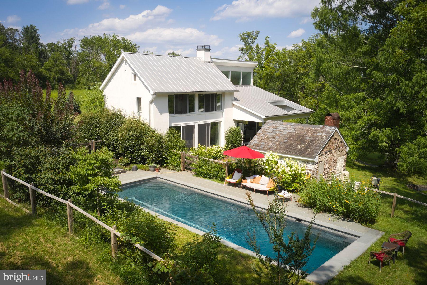 Retreat from the world on this expansive and private 89 acre Bucks County country estate.  A dream compound of two exquisite homes set within open fields and streams surrounded privately by mature forest of tulip, walnut, oak and pine.   Throughout the year your property will be the ideal place to observe the natural world from migrating hawks and eagles to deer, fox, and wild turkeys.   In summer it’s a festival of fireflies across the fields and into the forest canopy.  The mature landscaping around the houses has been designed to bring blooms and colors in every season.  

The Main House is a modern architectural gem built in 2013; it retains within its sculptural form the original 1805 farmhouse. Enjoy the charm of antique wood beams, pumpkin pine floors and a massive walk-in stone fireplace.  The rest of the home complements the charm of antique with a 21st century open plan featuring a chef’s kitchen and dining room under a two-story windowed cathedral ceiling and featuring natural slate floors, olive-veined black soapstone countertops, 6-burner Wolf Range, vast pantry space, and panoramic views that link indoors and outdoors. A NanaWall system opens the entire kitchen wall to the large slate patio overlooking a magical Dawn Redwood tree. Throughout the day, observe the sun and clouds shift sculpturally bathing the house with light. Upstairs, the expansive bedroom incorporates the vaulted ceiling and the pumpkin pine floors of the old farmhouse with a window wall toward serene views of the woods and stream.   The primary bath has slate floors and exquisite ceramic tile walls that surround a large soaking tub and glass shower.  The modern vanity is topped with olive-veined black soapstone.  

The Barn is its own sanctuary. This two to four bedroom renovated retreat is recently clad in antique barn boards and topped with an antique weather vane. Enjoy panoramic views of the property’s fields and distant views of the hillsides along the Delaware River from each room and the expansive terrace. The Barn kitchen has been renovated using antique barn wood.   There is also a second large and sunny temperature-controlled space appropriate for more living quarters, studio, or gym.   The third level of the barn is available for future development.
Both homes are heated and cooled efficiently by geothermal energy systems that use neither natural gas nor oil.   The windows in the main house are all thermally insulated and bathrooms and kitchen have radiant heating systems available.  

A wonderful gathering spot on the property is the large heated pool in a serene and private setting surrounded by mature plantings and looking out into the surrounding forest.   The pool has a tiled lap lane, bluestone deck and automatic pool cover.  The charming 19th Century Summer kitchen is ripe for use as a pool pavilion or writer’s cottage. 

On the land, enjoy the privacy and quiet, pick peaches, plums, and persimmons from your own orchard, raise vegetables in sun-drenched gardens. 

While the property feels like a retreat from the world, it is within 90 min. from NYC and Philadelphia and is surrounded by charming river towns of Frenchtown, Riegelsville, and Stockton, NJ, and Easton, Bethlehem and New Hope, PA.