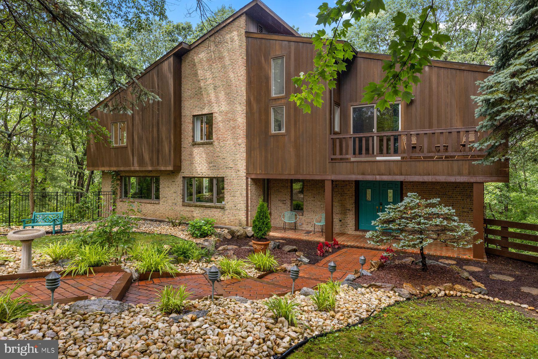 Tucked within the coveted Pine Top Trail enclave known as Camelot, this striking cedar and brick Contemporary offers a refined, design-forward lifestyle surrounded by the natural beauty of a private 1.12-acre wooded setting. Set quietly at the end of a cul-de-sac in Bethlehem, the home’s 5,209 SF of reimagined living space blends architectural drama with a warm, modern sensibility inspired by classic Mid-Century Modern design.
A landscaped approach and covered front porch introduce interiors filled with light, volume, and texture. Towering walls of glass frame verdant views from nearly every room, while extensive renovations have elevated the home with newly refinished oak floors, new hardwood flooring throughout, custom louvered railings and millwork, designer lighting, and beautifully updated baths featuring distinctive tile, curated fixtures, and timeless finishes. Opened sightlines and thoughtfully redesigned spaces create effortless flow for entertaining, everyday living, and flexible multi-generational arrangements.
The main living areas are both expansive and inviting. A dramatic living room with soaring 24-foot ceiling, brick accent wall, and fireplace with newer pellet stove anchors the home, while glass doors open to an expansive deck and screened porch overlooking the treetops. The spacious family room flows seamlessly into the stylish eat-in kitchen featuring freshly painted cabinetry, generous prep space, new appliances, and an LP cooking station designed for gathering as much as cooking. Nearby, the vaulted dining room is perfectly scaled for intimate dinners or larger celebrations, while the glass-enclosed sunroom offers a peaceful retreat immersed in nature.
The private primary suite is a true sanctuary with vaulted ceiling, balcony access, multiple closets including a walk-in closet, and a stunning renovated bath with freestanding soaking tub, double-head shower, marble-topped dual vanity, brass fixtures, and designer tile. Additional bedrooms and updated baths continue the home’s polished aesthetic throughout.
A richly detailed library with custom built-ins, additional guest bedroom, and flexible lower-level living quarters with separate entrance provide exceptional versatility for guests, extended family, au pair, or work-from-home needs. The lower suite includes a den with brick wood-burning fireplace, full bath, and fifth bedroom with direct access to the patio and spa area.
Outdoor living is equally compelling, with layered decks, screened porch, spa terrace, mature trees, and beautifully landscaped grounds creating a private resort-like atmosphere. An oversized two-car garage, curved brick driveway, security system with exterior cameras, and convenient proximity to shopping, dining, major routes, and Lehigh Valley International Airport complete this sophisticated contemporary retreat. Approximately 100 minutes to New York City and 80 minutes to Philadelphia. Please note that the interior photos have been digitally altered to remove the furnishings since the house is now vacant.