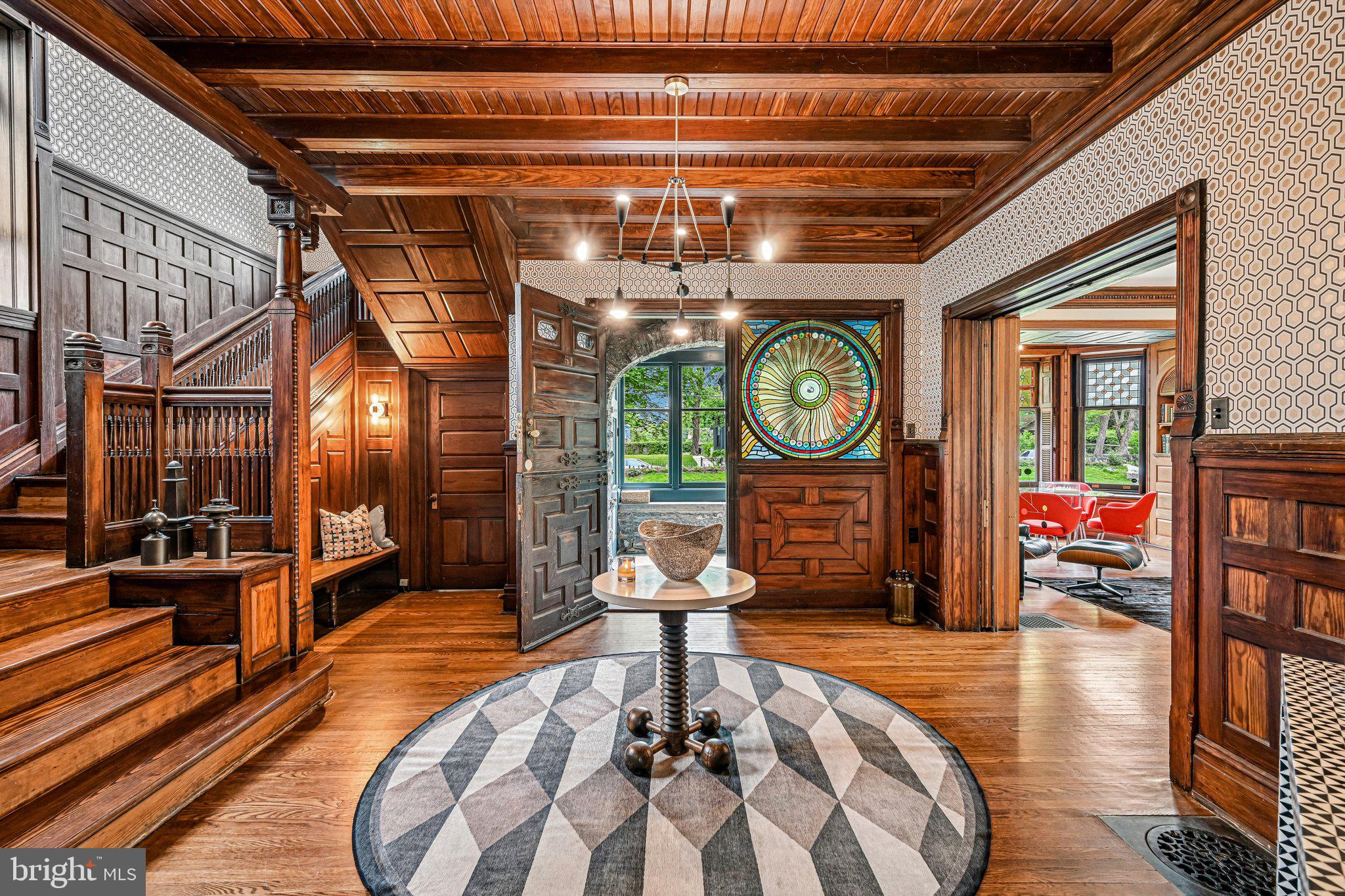Occasionally, a home with truly one-of-a-kind architectural elements is thoughtfully reimagined with deep respect for its original character. Welcome to 51 E. Penn Street, a distinctive Germantown residence designed by George T. Pearson, offering a rare opportunity to own a historically significant property where celebrated stewardship has seamlessly united the craftsmanship of the past with the comforts and sophistication of modern living.

This extraordinary home stands apart for its preserved artistry and cohesive design narrative centered around sun and star motifs, woven throughout its leaded and stained glass, millwork, and architectural detailing. A dramatic entry sequence introduces the home’s exceptional craftsmanship with richly preserved woodwork, intricate paneling, and striking original stained glass.

The main living space features a dramatic bay window with leaded glass, built-in oak bookshelves, and an ornate fireplace with integrated millwork and decorative floral relief tile. French doors open to a large patio, creating a natural extension of the living space for quiet mornings or evening gatherings.

A formal dining room, currently styled as a den and reading room, offers a second fireplace framed by richly detailed embossed ceramic tile with an organic floral motif.

The original butler’s pantry, complete with its copper sink and preserved cabinetry, remains a beautifully intact reflection of the home’s historic craftsmanship. The fully renovated chef’s kitchen was thoughtfully designed for modern living and entertaining, featuring a large island topped with Arabescato marble and deVOL plumbing fixtures. The adjacent mudroom includes laundry, powder room, and access to an expansive elevated patio ideal for outdoor dining and entertaining.

Upstairs, the second floor offers a spacious primary suite with sitting area, walk-in closet, wood-burning fireplace, Juliet balcony, and a beautifully updated en-suite bath with a curbless glass-enclosed shower, soaking tub, and radiant heated floors.

A second bedroom with its own wood-burning fireplace, generous linen storage, and an additional full bath with a large glass-enclosed shower complete this level.

The third floor provides three additional bedrooms and another updated full bath, offering flexibility for guests, offices, or creative spaces.

Additional highlights include a two-car garage with extra off-street parking, two-zone central air, custom Indow interior window inserts, fully updated electrical systems, and new copper water service.

Ideally located just 0.2 miles from Germantown Friends School and Pomelo Flowers, 0.3 miles from SEPTA’s Wister Station, 1.1 miles from Weaver’s Way Co-op, and 1.6 miles from the Wissahickon trailhead.

With extraordinary millwork, original hardwood floors, irreplaceable stained glass, and thoughtfully executed upgrades throughout, 51 E. Penn Street represents a rare opportunity to own an architectural work of art- a home where history, design, and modern living exist in exceptional balance.