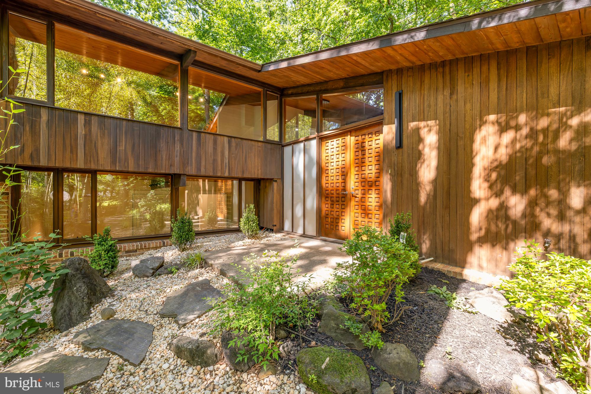 Tucked deep in the leafy quiet of Lake Barcroft Cloisters, this fully reimagined mid-century modern is one of the most architecturally distinctive homes to come to market in the community.
From the moment you arrive, the home announces itself differently — a zen-inspired entry garden of bamboo, river rock, flagstone, and flowering shrubs frames a striking dark wood facade with soaring rooflines and floor-to-ceiling black-framed windows. This is not a renovation. This is a reinvention.
Step inside to a breathtaking open great room where a vaulted wood-plank ceiling with exposed dark beams stretches the full length of the home — a signature mid-century architectural feature that floods the space with warmth and drama. Walls of glass and sliding doors open to a massive wraparound deck canopied by mature trees, blurring the line between inside and out. The chef's kitchen anchors the center of it all: a long quartz waterfall island, warm walnut cabinetry, professional range framed by matchbook-cut stone that mirrors the countertop slab, and a gorgeous deep blue subway tile backsplash that adds a rich, unexpected pop of color against the warm wood tones. Refined without being cold — every finish feels intentional.
The main level hosts two bedrooms including the private primary suite with walk-in closet and ensuite bath, joined by a second bedroom and full bath — ideal for guests or single-floor living. A family room, dining area, breakfast nook, and loft complete a main floor designed for both everyday living and effortless entertaining. An oversized deck connects you with the outdoors, giving plenty of space to entertain, dine al fresco, and enjoy the surrounding nature. The lower level features four additional bedrooms — including a generous room with its own walk-in closet — plus a large flex room, recreation room, two full baths, laundry, and dual utility rooms — space and flexibility for every lifestyle. Multigenerational living, home office suites, guest quarters — this floor handles it all without compromise. With 6 bedrooms, 4.5 baths, and 4,182 finished square feet across two thoughtfully designed floors on a private 0.42-acre lot, this home delivers scale, style, and soul in equal measure.