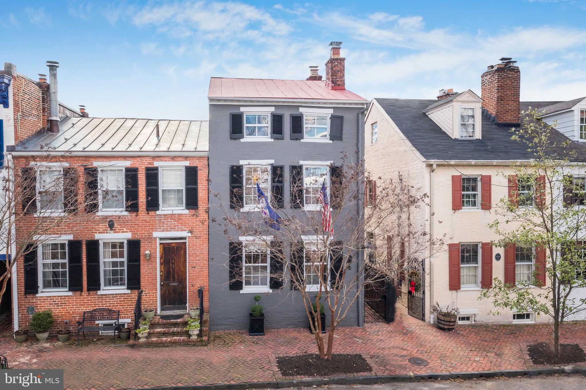 Built in 1820 and commemorated with a lovely plaque, this rare, historic semi-detached brick home in Old Town sits on a beautiful tree-lined block, in an excellent location near it all! Classic elegance meets modern luxury within this finely-renovated gem featuring 4 bedrooms, 2 and a half baths, and a gracious layout for living and entertaining. 

Charming gas lanterns, window shutters and boxwoods, American and Virginia flags, a standing seam metal roof, along with an iron-gate entrance and herringbone-patterned brick walkway to the main side door create welcoming curb appeal. Time outside is yours to enjoy on the large, private fenced-in patio garden with hydrangeas and azaleas, a perfect setting for lounging, reading and alfresco dining. Enhancing the allure is an irrigation system for planted areas and a delightful shed/unique brick artist studio off the patio brightened by 2 windows and a skylight.

Generous interiors of the house are also light-filled thanks to windows on triple exposures and a windowed stairway. Wonderful elements grace the ambience such as rich hardwood floors throughout, gorgeous original exposed brick in the front entry hall, 4 fireplaces, and tasteful moldings and millwork. The inviting living room/parlor is expansive and comfortable with 2 fireplaces and handsome built-ins. Prior owners used this room for living and dining, leaving a remaining chandelier connection under the ceiling plaster in the dining area should the new residents desire that layout. However, there is a wonderful separate formal dining room awaiting for your dinner parties, with access to the side patio garden via glass-paneled French doors.

The cook will delight in the offerings of the stunning renovated kitchen with a 13’ vaulted ceiling with wood beams, abundant cabinetry, Cambria quartz countertops in Dovedale White, a wood island/table, and premium stainless steel appliances including a gas oven/cooktop. An arched window overlooks a glorious Japanese red maple tree and the artist studio, and a glass door opens to the patio garden for hosting outdoors in warmer weather. A washer and dryer closet in the kitchen affords laundry ease. Plus, there is a guest powder room with marble floor completing the main level.

Sleeping quarters reside upstairs and provide a peaceful place to unwind. The primary bedroom is divine with a fireplace, sunny windows, 2 big closets, and a full hall bath with additional closets. The second bedroom with a fireplace and double closet is currently used as an office. Bedrooms 3 and 4 are well-appointed, one with built-ins, the other with plaid wallpaper from the UK.

Making this special home even more irresistible is the idyllic address in the coveted southeast quadrant of Old Town, minutes to shops, restaurants, parks, the river, public transportation, and the Mt. Vernon Trail.