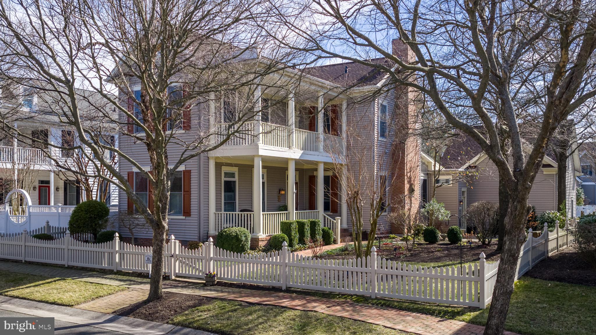 This two-story Charleston-style Colonial is located in the desirable Cooke’s Hope Village community and sits on an oversized lot with a fenced side and rear yard. The property includes a spacious entry-level side porch, second-level balcony, lush seasonal gardens, and a private fenced brick courtyard with built-in speakers for music and a retractable awning—perfect for outdoor entertaining. Hardwood flooring runs throughout the home. The main level offers a flexible layout with a bedroom just off the entry and a nearby full bath. The kitchen features double wall ovens and a gas cooktop in the island and opens to comfortable living spaces. The living room includes a gas fireplace, while the family room offers custom built-ins, a Vermont wood stove, and direct access to the courtyard and backyard. Upstairs, the primary suite includes a large bath with soaking tub, stall shower, and double vanity. A second en-suite bedroom currently serves as an office with extensive custom built-in cabinetry and could easily convert back to bedroom use. The second level also includes a generously sized laundry room. A mudroom off the attached two-car garage provides access to the side yard and leads to a staircase accessing a finished bonus room above the garage. This flexible space features independent heating and hot water and offers excellent options for guests, workspace, or additional living area. Custom built-ins are also found in the garage, family room, bedroom, and office.  Additional improvements include a roof replacement in 2025, upgraded heating system in 2020, and a Rinnai hot water system. The property also features an irrigation system to maintain the beautifully landscaped grounds. Cooke’s Hope residents enjoy walking trails, tennis courts, fitness center, dog park, and well-maintained community green spaces.