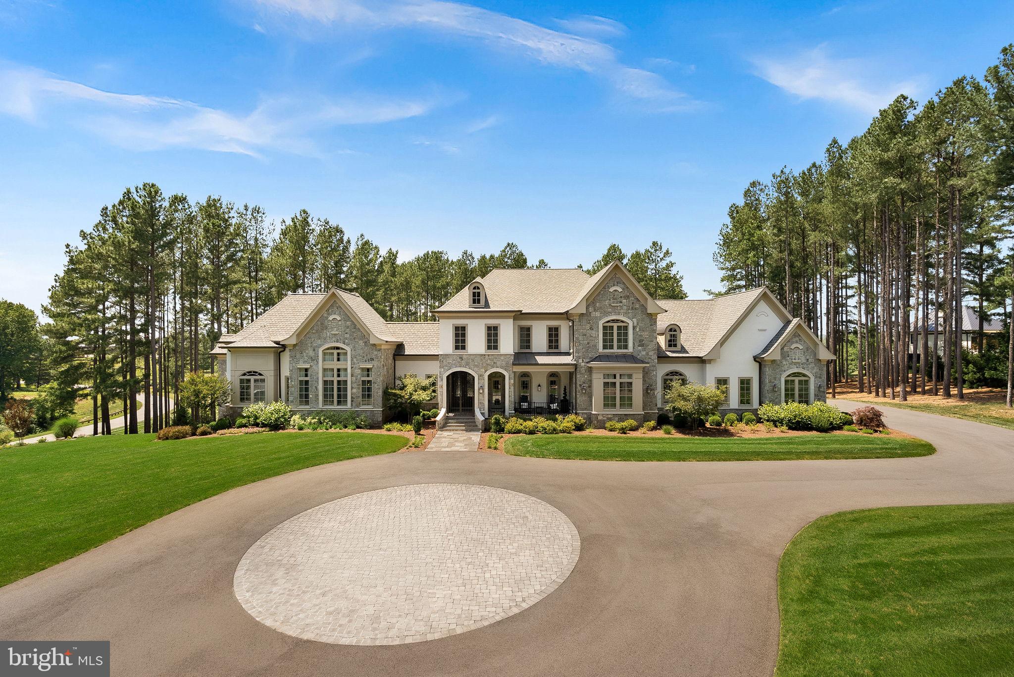 Within the preeminent Estates at Creighton Farms, this extraordinary residence, completed in 2023, sits on 3.25 acres where exceptional architecture and meticulous craftsmanship exist in sublime harmony. A timeless stone-and-stucco façade, complemented by extensive hardscape and curated landscaping, sets a distinguished tone. Ornate iron scrollwork gates open to the front porch, where stately double doors introduce the refined interiors on the other side.

Grace and sophistication unfold throughout the first floor, where 10’ ceilings, distinctive crown molding, elegant wainscoting, recessed lights, and a combination of tile and wood flooring create an atmosphere of understated luxury.  A columned gallery leads to the great room, where a coffered tray ceiling and stone surround fireplace provide a striking focal point. Nearby, dual chandeliers cast a warm glow over the dining alcove, while an adjacent dry bar ensures effortless entertaining. Designed for those who appreciate culinary creativity and freedom, the kitchen is anchored by a spectacular 10' x 6' quartz island that naturally draws guests together. A Bertazzoni range with a warming drawer and pot filler, double Cove dishwashers, and 36-inch stand-alone Miele refrigerator and freezer create a kitchen designed for both exceptional entertaining and everyday living.  A well-appointed butler's pantry and a fireside breakfast nook complete the space, blending timeless elegance with effortless functionality.

Your main-level primary suite is a private sanctuary, highlighted by soaring 15’ ceilings with double tray detailing, custom dual closets, and an exclusive balcony overlooking the tranquil grounds. Its impressive ensuite rivals a luxury spa, featuring heated floors, separate sink vanities, a mirrored makeup station, an elegant clawfoot soaking tub beside sunlit windows, and an oversized shower with a rain shower head and built-in benches.  Upstairs, 9’ ceilings continue throughout three beautifully appointed bedrooms, each with an adjoining bath, while a thoughtfully placed hall kitchenette adds both convenience and flexibility.

The walk-out basement is crafted for entertaining on a grand scale, with a wet bar finished with Dekton countertops, a beverage refrigerator, full dishwasher, ice machine, and a temperature-controlled wine cellar. A recreational area with a stone fireplace and billiards corner, a dedicated fitness studio, an ensuite guest room, a powder room, and abundant storage complete this remarkable haven.

An upper-level veranda features motorized screens, Infratech built-in heaters, and a fully equipped outdoor kitchen with a 42” Lynx infrared grill and beverage refrigerator. Below, a sunlit terrace overlooks the fenced lawn, while an inviting fire pit creates an idyllic setting for memorable evenings.

Notables include five HVAC zones, an elevator, whole-house generator, a laundry room with cabinets and dog bath, and an attached 3-car garage. Moments from championship golf, acclaimed wineries, fine dining, boutique shopping, and historic downtown Leesburg, come experience a home where every detail has been thoughtfully composed to elevate the everyday!
