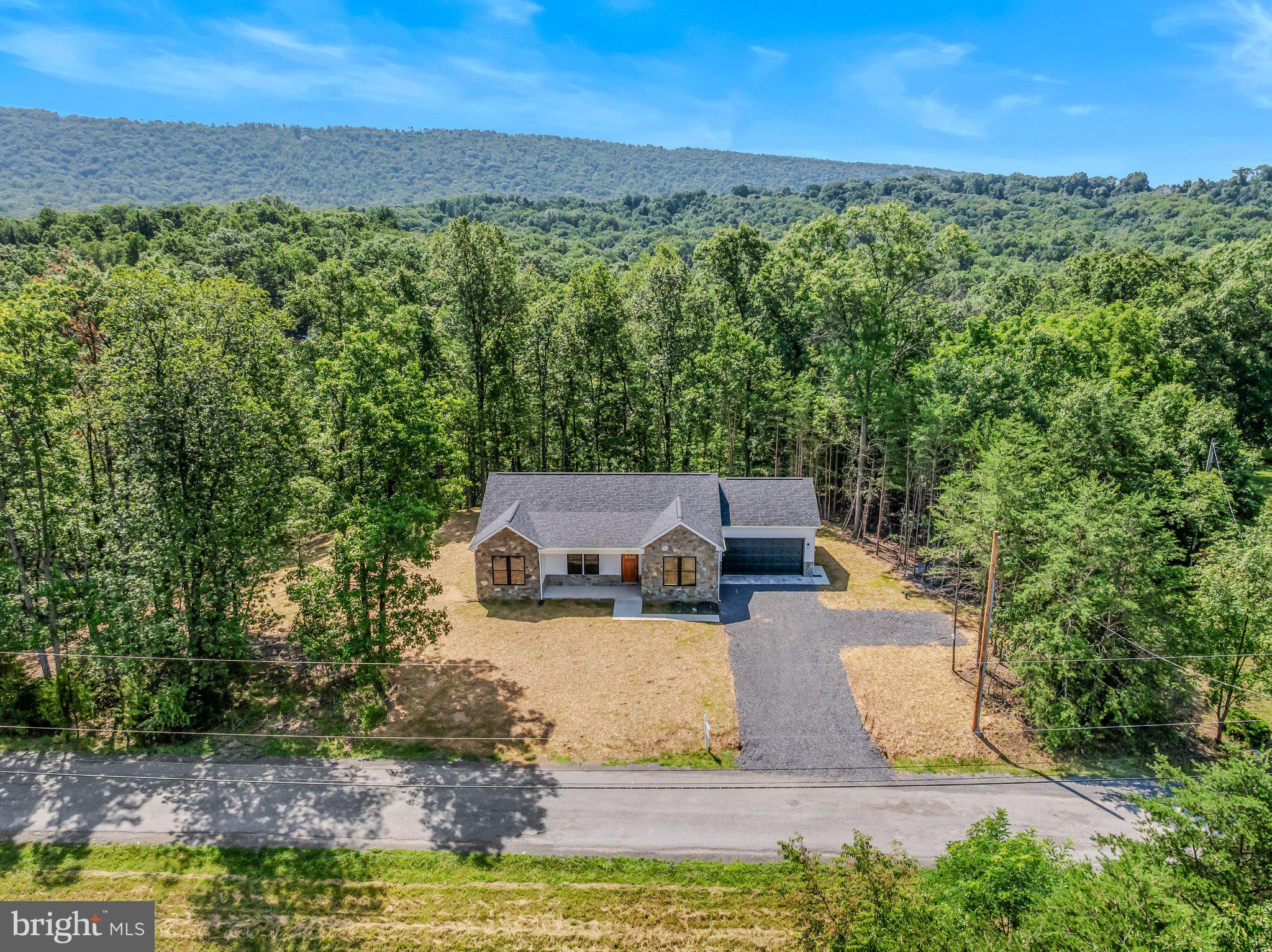 THIS NEW HOME IS COMPLETE and offers a rare blend of modern comfort in a peaceful setting—an ideal retreat from the pace of everyday life.  Located on 5+ wooded acres, this single-level home features approximately 1,600 finished square feet of living space and is thoughtfully designed with a layout that features 2 x 6 exterior walls, 3 bedrooms, 2 full baths, and a separate laundry room for added convenience. Rich solid hardwood flooring flows throughout the main living areas, including the bedrooms, adding warmth and timeless appeal. Ceramic tile adorns the bathrooms and laundry room for easy maintenance.  The kitchen is equipped with sleek stainless steel appliances, and the living room offers a vaulted ceiling to create a contemporary space ready for everyday living and entertaining. Just beyond the kitchen and dining area is the rear deck where the sights and sounds of nature take center stage—perfect for morning coffee, evening unwinding, or simply taking in the quiet beauty of the surrounding woods. A full, unfinished walkout basement with a full bath rough-in provides excellent potential for future expansion—whether you envision additional living space, a recreation area, or a private workspace. The insulated two-car garage offers enhanced protection against the harsh winter cold, thereby enhancing both convenience and functionality. Ideally located, this property offers the feeling of being “away from it all,” while still maintaining accessibility—approximately 30 minutes to Winchester, VA, Martinsburg, and Cacapon Resort State Park. Surrounded by natural beauty and set in a serene environment, this home delivers the balance of privacy, space, and modern living that you're searching for.  So, if you’ve been dreaming of a place where you can relax, recharge, and enjoy the outdoors—this is it.
