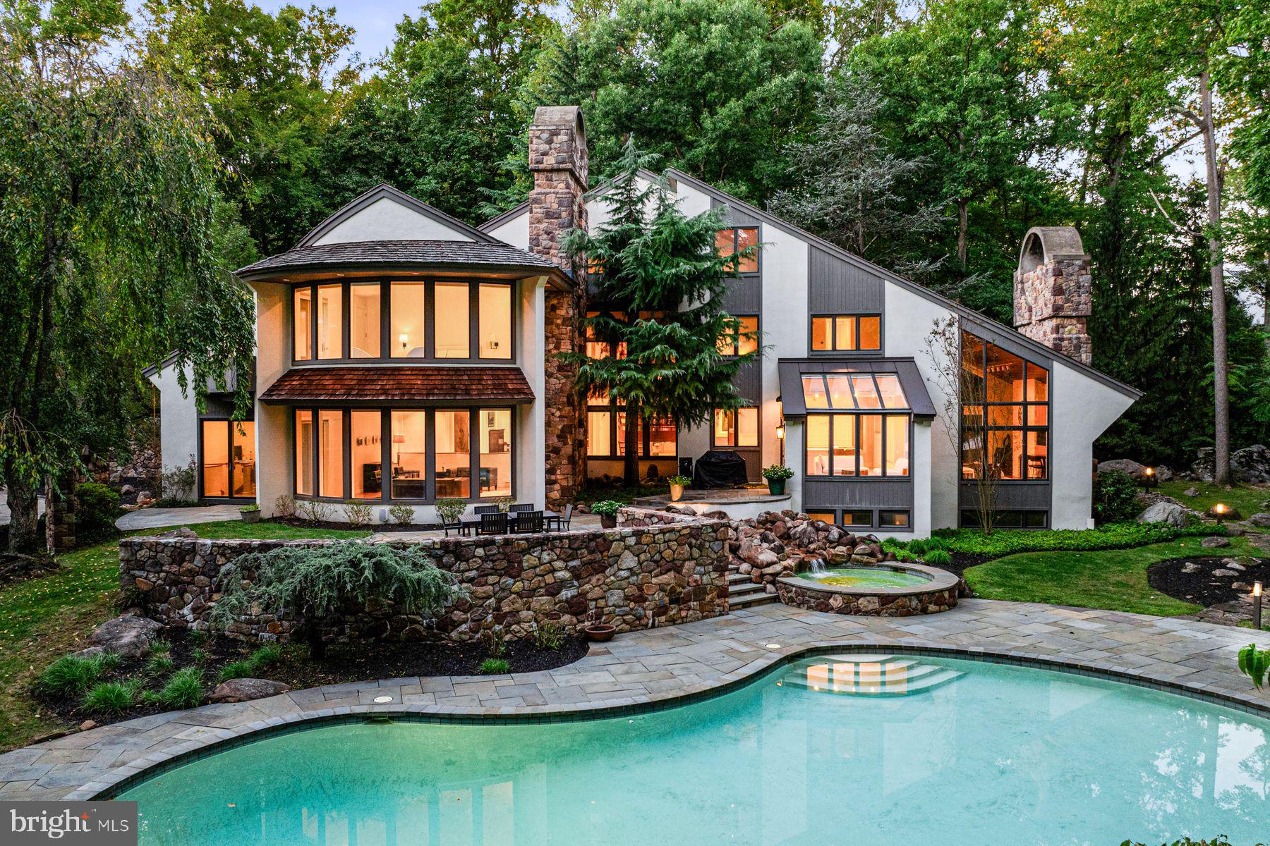 In one of Chester County’s most prestigious neighborhoods, this secluded 8,500 sq ft estate offers nearly four acres of private, luxury living with sweeping forest and stream views, a heated pool and spa, breathtaking architecture, and light-filled interiors crafted for both grand entertaining and everyday comfort.
Approach the property from a hidden extension off an already-quiet cul-de-sac, and be welcomed by a stunning stone driveway, additional stone-lined guest parking, and charming stone steps leading through the yard to the front entry.  Approaching the home, you’ll notice the privacy and rare connection to nature, while enjoying the warmth of a neighborhood where homes are hidden from view yet close enough for a friendly community feel.  The convenient location is unparalleled, with shopping and dining on the Main Line just minutes away, as well as the nationally acclaimed T/E School District. This unique combination- private retreat in nature with top-tier schools and local amenities minutes away- is rarely found.
Here, mornings begin in a peaceful habitat where you wake to birdsong and rustling leaves, and enjoy your coffee while watching deer, chipmunks, and turtles visit from the surrounding forest.  Designed by acclaimed architect Mark Stanish and crafted by Pohlig Builders, the home offers light-filled spaces with beautiful forest views from every room. 
The primary bedroom is a true haven with a curved wall of windows, a deck overlooking the wooded grounds, and a 14-foot heated cathedral ceiling. The spa-like bath features a two-person Jacuzzi with marble surround, heated floors, a seated shower, and dual walk-in closets.
The soaring 3-story travertine foyer sets the tone for welcoming guests, framed by dramatic walls of windows. The spacious living room features oak floors, a gas fireplace with carved stone mantel, and glass doors opening to a slate terrace with forest and stream views. The formal dining room dazzles with marble floors and sliders to a private deck, perfect for intimate dinners. Multiple home office spaces invite creativity, with gorgeous views, unique rooflines, and oak floors.
At the heart of the home, the chef’s kitchen is outfitted with Gaggenau gas cooktops, a grilling station, induction cooktop with range hood, Bosch dishwasher, Sub-Zero refrigerator/freezer and ice maker, double ovens, and abundant cabinetry and prep space. The sun-drenched breakfast room, with windows on all sides, opens directly to the terrace and outdoor grilling area, while the adjacent family room boasts an 18-foot vaulted ceiling, built-in cabinetry, a stone fireplace, and floor-to-ceiling windows bringing the outdoors in.
The expansive lower level is an entertainer’s dream, with a wine tasting room and classic brick wine cellar for 550 bottles, an Art Deco kitchenette, custom bar, and refreshed recreation spaces including a finished exercise room, pool table room, media room with fireplace, automated shades, movie-size TV, and game zone with foosball and air hockey—ideal for movie or pizza nights.
Outside, the heated pool and spa form a boutique-resort oasis beneath a canopy of trees, with surrounding flora, outdoor speakers, and subtle lighting for both sunny afternoons and evening swims.
With its rare blend of natural beauty, architectural sophistication, and premier location, this property is more than a home—it’s a private sanctuary where luxury, design, and nature exist in perfect harmony, just minutes from the heart of the Main Line.
