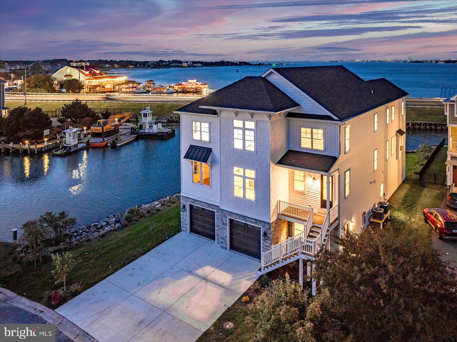 Stunning custom 5BR/5BA estate is located in the prestigious Estates at Inlet Isle Lane in West Ocean City.  This custom home showcases exceptional craftsmanship, a unique architectural style, and an unbeatable waterfront location. With panoramic views of the marina, bay, canal and ocean, this property offers the perfect setting to enjoy endless sunrises and sunsets. Boating enthusiasts will appreciate the deep-water slip that accommodates up to a 42-foot boat, providing easy access to the ocean through the inlet. The home’s exterior is sleek and modern, featuring clean white lines, stone finishes, and striking black accents that complement its coastal setting. Upon entering the first floor, you’ll find a spacious recreation room and a full bathroom—ideal for entertaining guests or relaxing after a day on the water. An elevator or staircase leads to the second level, where a gourmet kitchen awaits. This chef’s kitchen includes high-end appliances, quartz countertops, a custom coffee bar, and ample cabinetry, all set against a backdrop of wall-to-wall windows offering breathtaking water views. The adjacent family room features soaring ceilings, a dramatic floor-to-ceiling stone fireplace, and cedar wood accents that draw your eye to the expansive windows overlooking the bay. This open and airy space is perfect for entertaining family and friends. Also on this level is a luxurious primary suite complete with a large walk-in closet with custom shelving, a spacious custom shower, and a beautiful soaking tub. A second bedroom and bathroom are also located on this floor. The third level offers even more space to relax and unwind with a second family room/lounge area featuring another coffee bar and panoramic water views. This floor includes a second primary suite with its own spa-like bathroom, plus two additional bedrooms that overlook the marina.
Multiple decks on every level allow you to enjoy the fresh air and cool summer breezes from sunrise to sunset. The oversized garage provides plenty of space for large SUVs and all your beach gear, with potential to finish part of the space if needed. Located close to world-class marinas, golf courses, Assateague Island, the Ocean City Boardwalk, and some of the area’s best restaurants, this home offers the perfect blend of luxury, comfort, and coastal living. It’s a place where you and your loved ones can create memories that will last a lifetime.