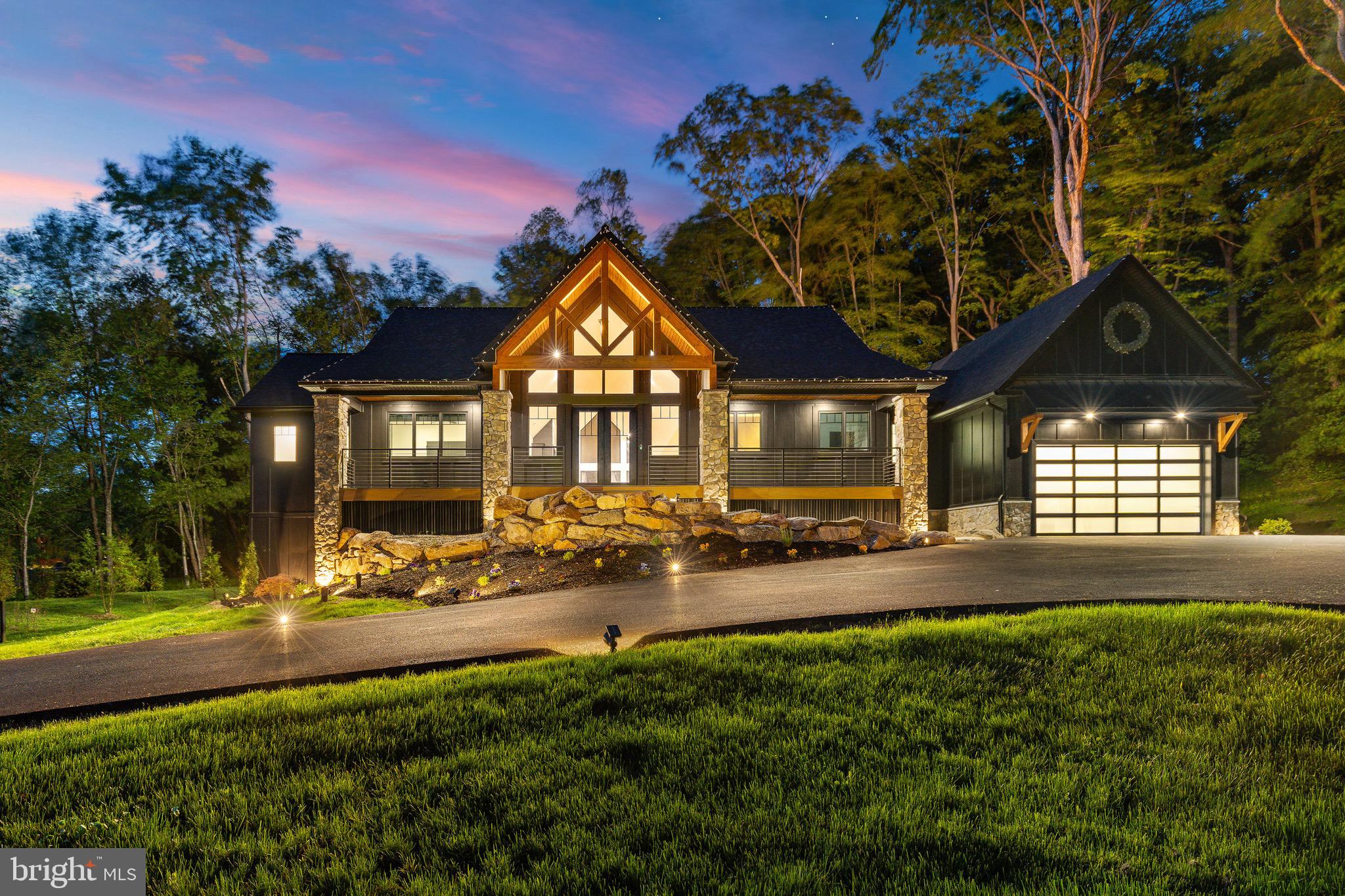 Introducing Midnight Ridge Manor, a striking architectural statement tucked privately among the trees in one of Doylestown’s most picturesque settings. As you wind down the long private driveway, the home slowly reveals itself through the landscape like a modern mountain retreat, where dramatic rooflines, warm stone accents, and illuminated walls of glass create an unforgettable first impression. Designed to feel both sophisticated and deeply connected to nature, this newly constructed luxury residence blends bold contemporary design with the warmth and serenity of a private woodland sanctuary.
At the heart of the home, soaring vaulted ceilings and breathtaking architectural windows flood the main living space with natural light while framing peaceful wooded views in every direction. The open-concept design was created for elevated everyday living and effortless entertaining, anchored by a dramatic floor-to-ceiling fireplace feature wall with custom built-ins and rich wood accents. Oversized 16’ x 8’ glass sliders seamlessly extend the living space outdoors to the expansive TimberTech deck and resort-inspired entertaining areas, complete with cable railings, extensive hardscaping, ambient lighting, and a stunning fire feature courtyard that feels truly magical at dusk.
The gourmet kitchen is both functional and beautifully curated, featuring custom inset cabinetry, quartzite countertops, a substantial center island, butler’s pantry, wine storage, and a full suite of premium GE Monogram appliances including a 48” six-burner range, double ovens, 30” refrigerator column, and 18” freezer column. Every finish was thoughtfully selected to create a refined yet inviting atmosphere throughout the home.
The main level primary suite serves as a luxurious private retreat with spa-inspired finishes, tranquil views, and direct access to outdoor living spaces. An additional bedroom and full bath are also located on the main level, along with a spacious laundry room designed for convenience and everyday ease.
The lower level continues the home’s exceptional design with radiant heated floors, a second family room, full kitchen and entertaining space ideal for extended guests or a private mother-in-law suite with kitchen. Two additional bedrooms and two full baths provide comfortable accommodations, while a dedicated fitness room is pre-wired for a future sauna, creating the ultimate wellness retreat experience.
Above the attached garage, a private additional bedroom and bath offer ideal flexibility for guests, office space, or an additional suite.
Built with uncompromising attention to quality and performance, Midnight Ridge Manor features Hardie Board and batten siding, standing seam roofing accents, ProVia Endure casement windows, solid wood doors and trim, hardwood flooring throughout, full-home audio, comprehensive security, Starlink commercial-grade satellite capability, WiFi access points throughout, closed-cell spray foam insulation, Rockwool mineral wool insulation, pre-wiring for a backup generator and 220 compressor, and numerous custom utility upgrades rarely found in residential construction.
Set on 1.31 serene acres with permit approval already secured for an 18x34 pool, Midnight Ridge Manor offers a rare opportunity to experience luxury living that feels both architecturally significant and deeply personal a modern retreat designed to be experienced as much as admired.