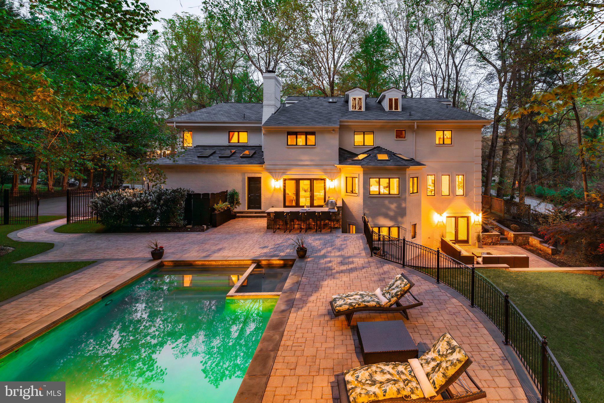 Prominently perched on over half an acre in Bethesda, 9200 Hollyoak Drive is a stately brick Colonial that has been thoroughly reimagined for modern living. Its crisp white brick façade delivers an immediate sense of sophistication, hinting at the balance of luxury and comfort to be found within.

A gently curving driveway opens into an expansive motor court, where a winding flagstone path leads to the front entry, gracefully set within a rounded stone turret.

Inside, the grand foyer makes a striking first impression—gleaming marble floors, a sweeping curved staircase, and a radiant chandelier suspended beneath a soaring double-height ceiling speak to the home's impressive scale. A guest powder room and deep coat closet are discreetly tucked away, while formal rooms unfold from the reception hall with seamless flow.

The study exudes a dignified presence with built-in shelving and the flexibility of an ensuite full bath and closet, allowing it to serve as a complete bedroom suite. Across the hall, the formal living room spans embassy scale, with a wood-burning fireplace and oversized windows framing the front lawn. Twin archways lead to the banquet-sized dining room, which connects directly to the showpiece kitchen.

Outfitted with high-end white shaker cabinetry, streaked marble countertops, and dark-stained hardwood floors, the kitchen offers both form and function. Its appliance suite includes a professional-grade Viking range and wall ovens, a coveted SubZero Pro 48 refrigerator, and three dishwashers tucked beneath a skylit bay window.

A dedicated wet bar with dual wine coolers serves the adjacent family room, which features its own fireplace, outdoor access to the kitchen terrace, and a dramatic opening to the sitting room above.

Completing the main level is a well-appointed mudroom with access to both wings of the three-car garage.

Upstairs, a sweeping circular gallery wraps the landing, leading to a private primary suite with its own fireplace and serene views over the front lawn. The suite includes a spa-like bath with soaking tub and walk-in shower, twin walk-in closets with custom built-ins, and an adjacent sitting room with an additional full bath.

Three secondary bedrooms offer generous proportions, each with walk-in closets and en-suite baths. The top level includes a versatile fifth bedroom or studio space, while the lower level boasts a full kitchenette, fitness center, lounge, and two additional baths.

Outside, lush landscaping, a turfed lawn, extensive paver hardscape, and a heated saltwater pool with cabana complete this private, move-in ready retreat.

Blending timeless architecture with thoughtful upgrades and exceptional outdoor amenities, 9200 Hollyaok offers an elevated lifestyle in one of Bethesda’s most prestigious settings.