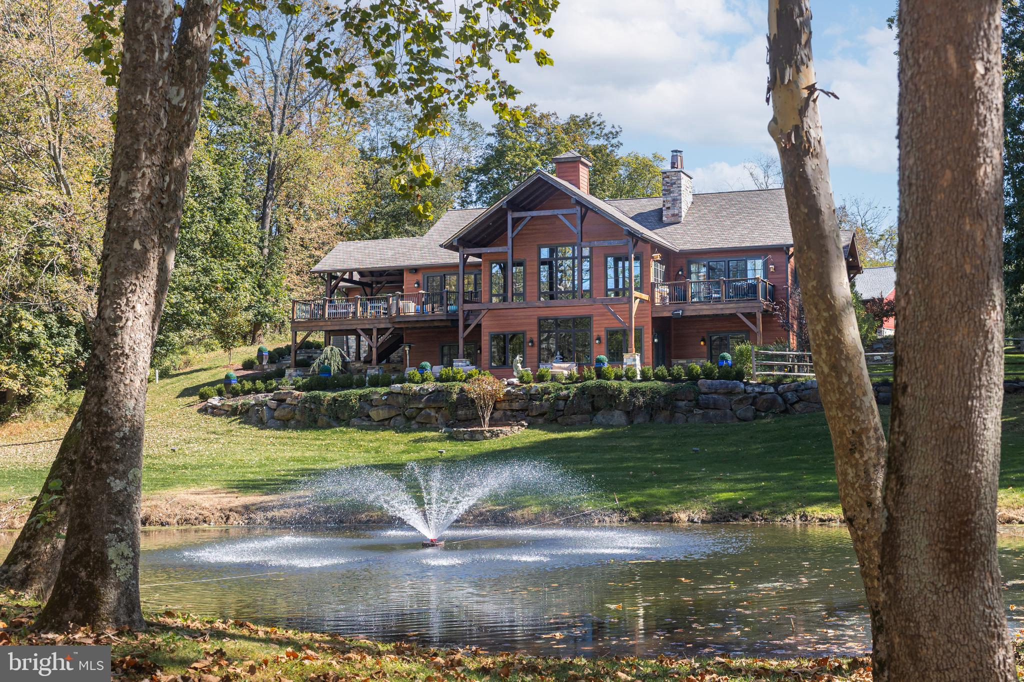 In the heart of Bucks County, this stunning 4-bedroom, 4 full baths & 2 half baths offers the perfect balance of rustic charm and modern comfort. From the moment you arrive down a long and private scenic driveway,  you’ll be captivated by the views, peaceful surroundings, and inviting design that make this property a true retreat.  Step inside to a bright and airy open-concept living space, where vaulted ceilings, exposed beams, and a stone fireplace create a warm, lodge-like atmosphere. Large windows frame an outdoor pond with water features and fill the home with natural light. The chef’s kitchen features "leathered" granite countertops, a center island with counter seating, stainless steel appliances, and ample space for both cooking and entertaining.  Adjacent to the kitchen is a spacious dining area which overlooks the outdoor beauty.  Step outside the kitchen and enjoy effortless entertaining or peaceful relaxation on the expansive deck that also includes an outdoor grilling area, offering the perfect setting for dining al fresco or enjoying quiet moments surrounded by nature.  The first floor primary suite offers a private escape with its own balcony, walk-in closet, and spa-like bath. Three additional bedrooms, one on the first floor and two on the lower level, provide flexibility for family, guests, or even a home office.   Step into the lower level and you will be greeted by an oversized family room, complete with a gas fireplace, wet bar sink, ice maker, mini refrigerator, dishwasher, wine cellar, and gaming area. In addition to the home's attached 2.5 car heated garage, there is a 7-door heated pole barn with electric. that can accomodate 10 cars. One of the doors is extra large to allow parking for a camper or a boat. This expansive space is perfect for an art studio, hobbyist, car collector, etc. This spectacular home delivers it all—comfort, privacy, and endless natural beauty just outside your door.