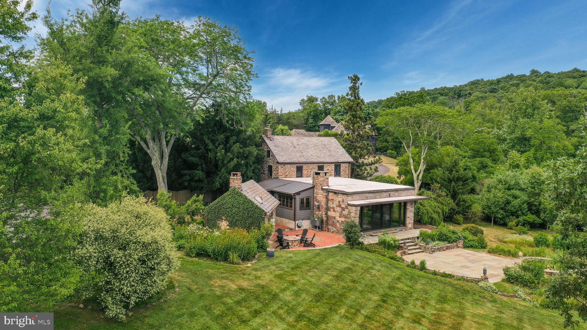 A scenic and serene landscape is the setting for Meadowview, a classic gentleman’s farm in beautiful Upper Bucks County. The 8-acre parcel is a blend of fields, gardens, and creek, a restful haven in a peaceful rural setting, yet close to everyday necessities. Circa 1813, the stone farmhouse retains pumpkin pine floors, deep silled windows, and exposed wood beams. An inviting den with coffee bar, and adjacent full bath and bedroom are found in this portion of the original dwelling. Upstairs, two additional bedrooms include a primary suite with a copper clawfoot soaking tub, spa shower and dressing room encompassing its own floor. Seamlessly integrated open and modern living space brings a stunning Great Room. A floor-to-ceiling stone fireplace and French doors to bluestone patios with breathtaking views stretching across the acreage to mountains in the distance enhance this area. The kitchen gleams with marble countertops, a Bertazzoni gas range, exposed stone wall and radiant heat flagstone floor and the former detached summer kitchen is now a cozy guest cottage with vaulted ceiling and stone fireplace. Wander the grounds to dozens of raised bed flower and vegetable plantings, putter in the sunny greenhouse, and stroll to the property’s perimeter where Cook’s Creek crosses the property. A gas fire pit provides the perfect spot to stargaze throughout the seasons. Standing near the home, a converted bank barn is a useful 2-car garage with EV hookup, equipment bay, and loft area suitable for hobbies and workspace. All within a 90-minute   of Manhattan and Philadelphia, country roads beckon for leisurely bicycle rides or a short drive to New Hope and the river towns along the Delaware. The Lehigh Valley to the north offers shopping, dining, and historic sites.