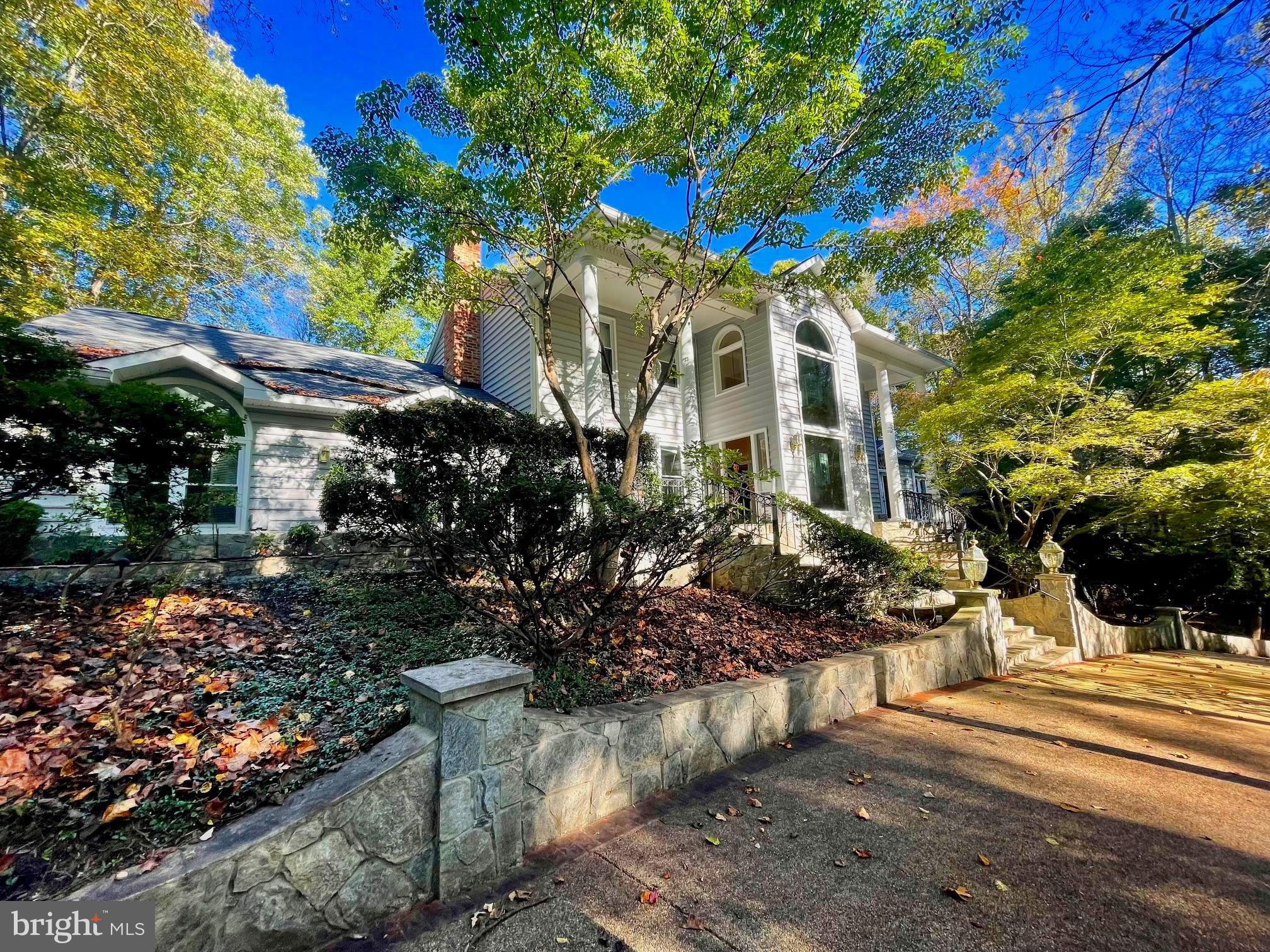 Can you imagine a property that is close to everything, but feels like a vacation retreat? Look no further than 2904 Brians Hill Lane, where protected parkland is outside your door. Nestled on a secluded lot in a 7-house enclave, this serene home sits near the end of a private lane off Fox Mill Road. With 5 bedrooms, 4.5 baths, and 6,868 finished square feet, the 3-level house was built for residents to embrace its space, but it's also perfect for holiday gatherings, weekend entertainment, and extended stays by friends and family. A NEW ROOF IS BEING INSTALLED WITH A 10-YEAR TRANSFERABLE WARRANTY TO THE NEXT OWNER. Interior features include a fabulous foyer with a two-story glass window,  a stately dining room, and a traditional kitchen with heaps of storage. The kitchen boasts a Subzero fridge and freezer, black marble countertops, and a comfy breakfast area.  Off the kitchen is a hallway that leads to a stunning Great Room with cathedral ceilings, a built-in mahogany bar, and a soaring two-sided stone gas fireplace to warm your party guests. On the opposite side of the fireplace is a sunken sitting room with steps that lead to built-in benches for relaxation. French doors on both sides open to a wrap-around patio/deck with wrought-iron railings and a new furniture set that conveys. The main level has a second wing, which includes a family room with a wood-burning fireplace, a cozy office to telework in, and a sunroom with skylights to warm your soul. A curved staircase weaves its way to the second level which features a large primary suite with a walk-in shower and a jet-soaking tub. Natural hardwoods lead to a full bath and three secondary bedrooms with built-ins and window views of the wooded backyard. With 4,900 square feet of space on the main level, there is plenty of room to carry out weekly chores. Next to a full bath sits a laundry room with two washer-dryer combo units. Clothes get cleaned twice as fast with these all-in-one machines. Guests will appreciate the fully-finished basement which can also serve as perfect living quarters for an au pair. The lower level includes a kitchenette, bedroom, full bath, bonus room, and den. It also features a walkout to a large covered patio and a workshop that can double as a storage room.
The fenced-in backyard includes a lovely stone grilling area for Summer BBQs and parking is easy with a 3-car garage and a half-circle driveway that leads to slate steps at the front of the house. Located in Oakton's High School Pyramid, it's 10 minutes from Fairfax City, 15 minutes from Dulles Airport, and within 20 minutes of shopping venues in Fair Oaks, Reston, and Tysons Corner. If you enjoy the metro, check out the new Silver Line station at Reston Town Center. Park and ride one way for a night out in Arlington, or go the opposite way for a flight out of Dulles. For those who work in DC, the home is a half-hour commute and a peaceful reprieve from the stress you leave behind. Tranquility lives at Brians Hill. Make this gem your own!