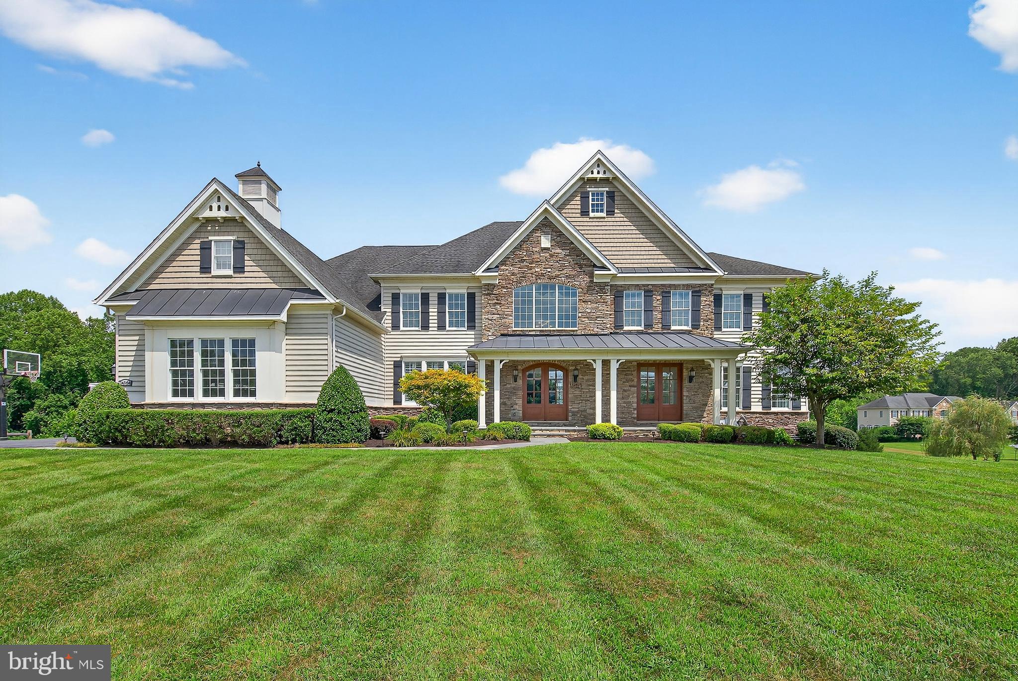 Welcome to The Reserve at Triadelphia Crossing, where luxury, craftsmanship, and elegance come together in this extraordinary stone and siding estate home offering over 10,000 square feet of meticulously designed living space. With 5 bedrooms, 5 full and 2 half baths, and a rare 4-car garage, this exceptional residence is nestled on a premium lot backing to serene woods and open space that will remain untouched—offering unmatched privacy and tranquility. Step onto the expansive covered front porch and into a grand interior featuring gleaming hardwood floors, rich crown moldings, custom wrought iron railings, and a dual staircase that frames the dramatic foyer. The heart of the home is a true gourmet kitchen outfitted with high-end stainless steel appliances including a Wolf gas stove, Sub-Zero refrigerator, new dishwasher, oversized granite island with prep sink and a breakfast bar, large walk-in pantry, and a butler’s pantry with wine fridge and mini-fridge—ideal for entertaining. Just off the kitchen, enjoy meals in the spacious breakfast nook or in the bright and inviting sunroom or step outside to a large deck that leads to a custom slate patio, complete with a built-in outdoor kitchen and stone firepit. The main level also offers a formal living and dining room, a spacious conservatory filled with natural light, a cozy family room with stone fireplace, private home office, a half bath, and a fully equipped mudroom with custom built-ins. The laundry room boasts brand new washer/dryer, sink, and abundant cabinetry. Upstairs, the lavish primary suite impresses with a tray ceiling, private sitting room, and an enormous walk-in closet that must be seen to be believed. The luxurious primary bath includes dual granite vanities, jetted Kohler tub, large walk-in shower, and two water closets. Bedrooms 2 and 3 each feature their own sitting rooms and en-suite baths, while Bedroom 4 offers an en-suite bath and attic access. The fifth bedroom is a step-up flex space, currently serving as a media room. The fully finished walk-out lower level is an entertainer’s dream, featuring a large recreation room, custom wet bar with pendant lighting, wine fridge, dishwasher, mini-fridge, ice maker, and rich cabinetry. The in-law suite includes a full second kitchen with stainless steel appliances, island, gas stove, and its own full bath. The basement also features a kids gym with 12’ ceilings and basketball goal, a separate adult gym or bedroom, powder room, and ample storage. Additional upgrades include 10' ceilings, whole-house audio, 4-zoned HVAC (2 gas furnaces, 2 heat pumps), an Amish-built custom shed with electric, a concrete pad with electric for future hot tub, and a peaceful backdrop of woods and open space. This is estate living at its finest—with too many upgrades to list. Prepare to be captivated by the style, space, and sophistication of this stunning one-of-a-kind residence.