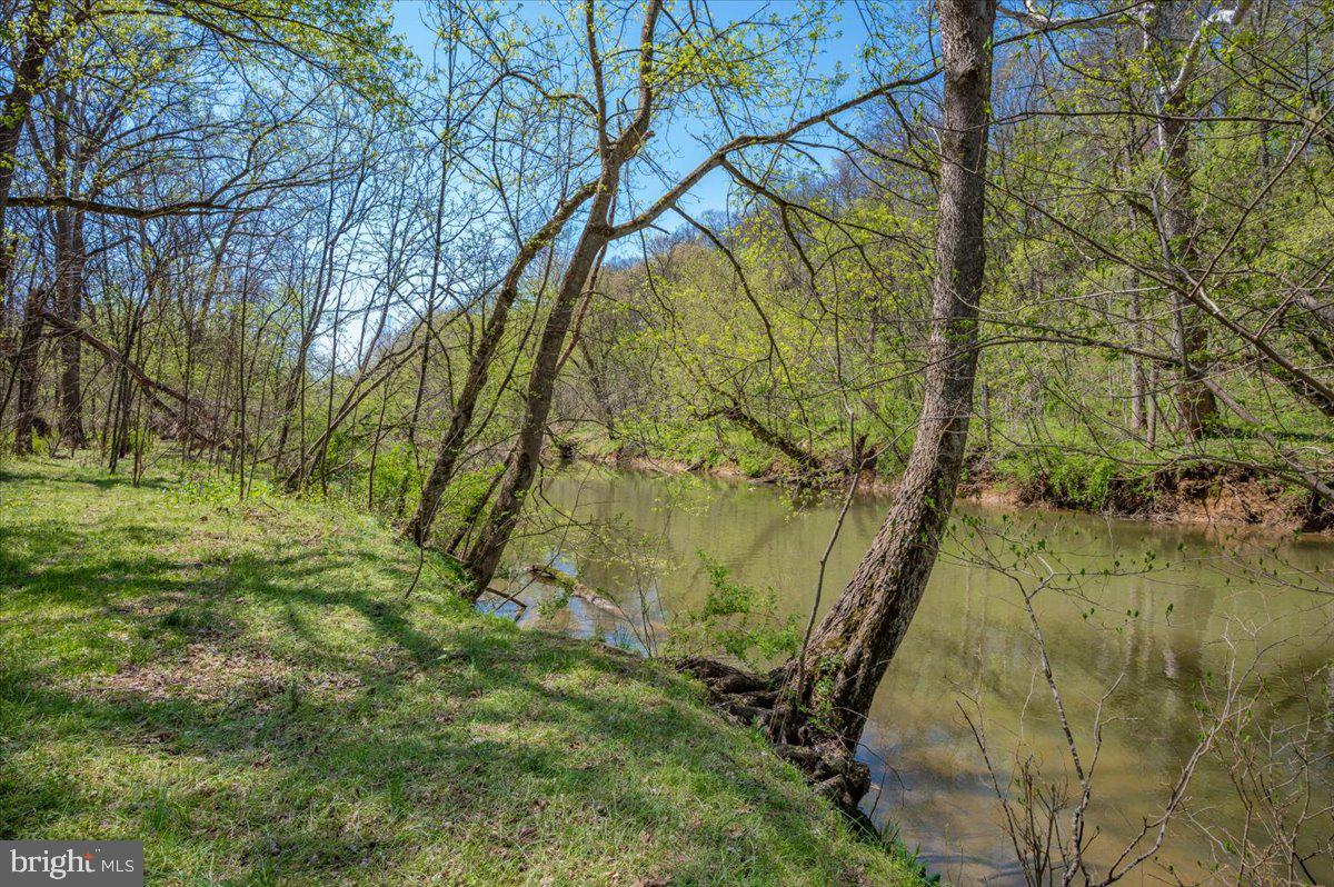 Summer on the creek has been waiting for you!  Welcome to this pretty 3 bedroom, 2 full-bath ranch home sitting on 3.46 private creekfront acres.  Call it home or call it your getaway.  Situated towards the end of a quiet roadway in the sought-after country community of Horseshoe Bend!  Country-living at its very best.  When you pull in the circular drive, you will notice a spacious front deck welcoming you.  It opens to a central living room, with two bedrooms and one full bath to the left.  To the right you will see the kitchen, another full bath, and stairway access to lower level.  Located on the  light-filled lower level is a walk-out to the back acreage, an additional bedroom/den, a huge family room, laundry facilities, and a bonus room now used for storage.  Creek views are visible from the home when the leaves are down.  Outside is a spacious yard for play and entertaining.  To the left of the home is an oversized workshop sitting close to the garden.   A path to the right of the home (look for the sign!) leads you to a small hike down to the creek and the spacious creekside resting area--perfect to sprawl out with a picnic or beverages.   Or, keep your floats and fishing rods close for adventures!  In addition to your own private 3.5+/- acres, just one parcel beyond is 42 community acres along Sharmans Run (an offshoot from the creek) to hike and explore.  Or enjoy the 32 +/- community acres just down the way for fishing, floating, walking, or just enjoying.  The HOA tends to the roadways and upkeep of community land.  Bring your pets, chickens, horse, and other critters.  Spend a little time enjoying seclusion or meet others in the community lands.  Either way, own your own hide-away for part-time or full-time living at its best.