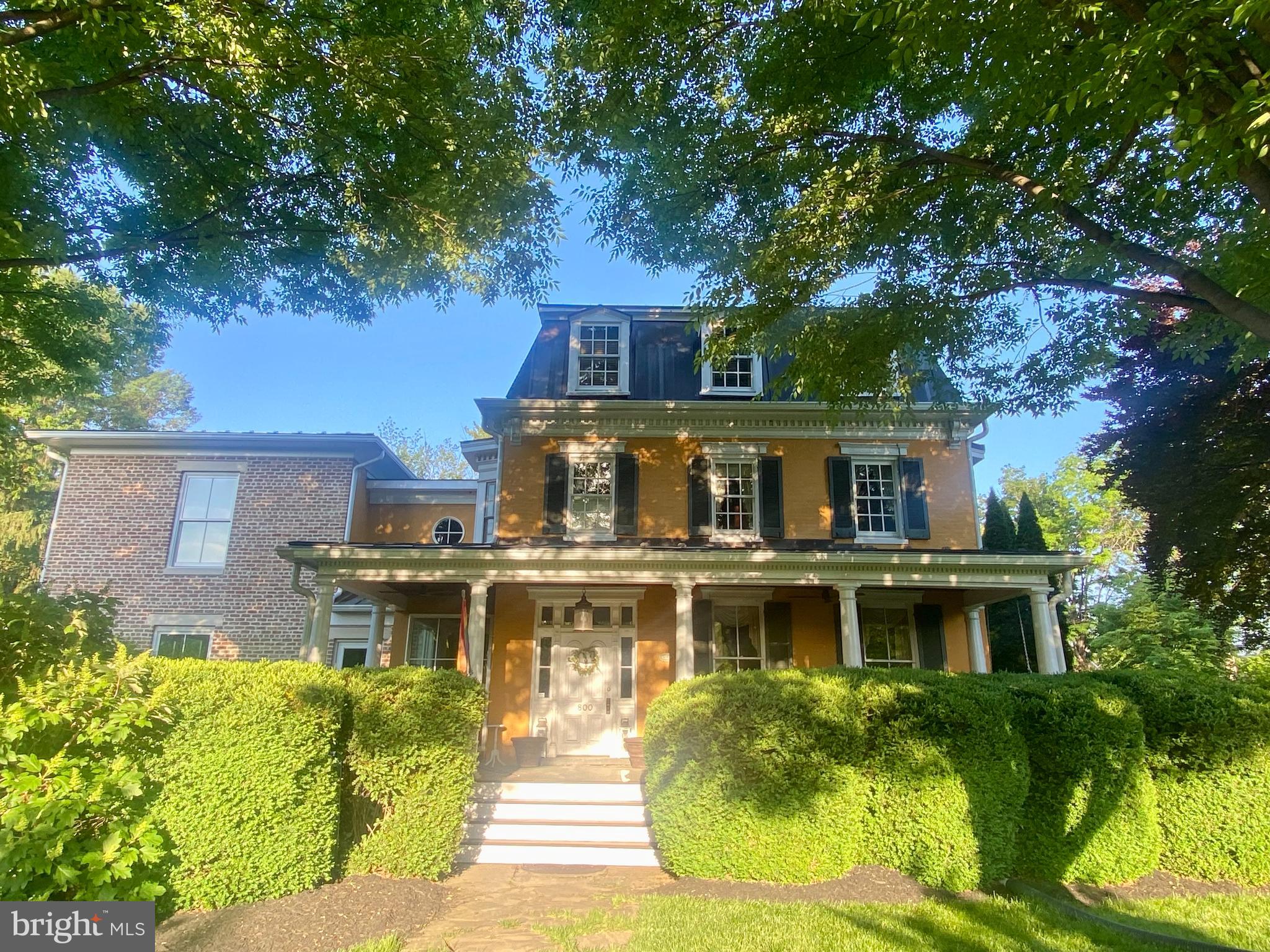 A once-in-a-generation opportunity to own one of Frederick’s most historically and architecturally significant residences—gracefully positioned along iconic Baker Park with views of the covered bridge and Carroll Creek.

Originally constructed in 1743 by Henry Brunner, brother of Elias Brunner—builder of what is now Schifferstadt Architectural Museum—this extraordinary property reflects the architectural evolution of Frederick from an 18th-century farmhouse into an elegant Second Empire residence crowned by a distinctive copper mansard roof, while a breathtaking modern addition seamlessly carries the home into the 21st century.

Set on a rare .93-acre lot fronting Baker Park, the home blends historic craftsmanship with striking contemporary design. A deep front porch—worthy of long afternoons on a porch swing—welcomes guests into a grand foyer with freshly refinished hardwood floors. To one side, a gracious formal parlor, currently serving as a dining room, honors the home’s historic roots, while the stunning modern addition unfolds with dramatic 10-foot ceilings, stained concrete floors, radiant geothermal heating, and walls of floor-to-ceiling windows overlooking the private backyard.

Architect Gary Baker and builder Tony Chmelik thoughtfully designed the addition to complement the original structure, even carrying the beadboard detail from the front porch ceiling into the new spaces. A curved wall of windows and beamed ceiling define the dining area, which opens seamlessly to both the kitchen and living room for effortless entertaining.

The living room features custom built-ins and sophisticated architectural lines, while the kitchen offers extensive floor-to-ceiling cabinetry, abundant workspace, center island, and gas range designed for serious cooking and gathering. Behind the kitchen, the original family room showcases thick stone walls, wood floors, and a substantial fireplace connecting to the former summer kitchen.

The second floor features an extraordinary primary suite with two walls of windows, a custom walk-in closet, and a luxurious ensuite bath with dual vanities and an impressive stone, tile, and glass shower. Three additional large bedrooms, two more full baths, bedroom-level laundry, and a flexible gym or office space complete this level.

The third floor serves as a private suite with walls enhanced by reclaimed barn wood, a spacious full bath, and preserved remnants of the home’s former widow’s walk access.

With over 5,400 square feet above grade plus a finished basement rec room, this home offers remarkable scale while maintaining warmth and livability. Modern amenities include geothermal heating and cooling and on-demand hot water.

Perhaps most extraordinary is the original stone-vaulted cellar, a feature shared with the nearby Schifferstadt Architectural Museum. Beneath the home, a natural spring still flows through a trough at approximately 60 gallons per minute—once serving as the home’s water source and now supporting the geothermal system.

An irreplaceable blend of history, architecture, and modern luxury in one of Frederick’s most iconic locations.