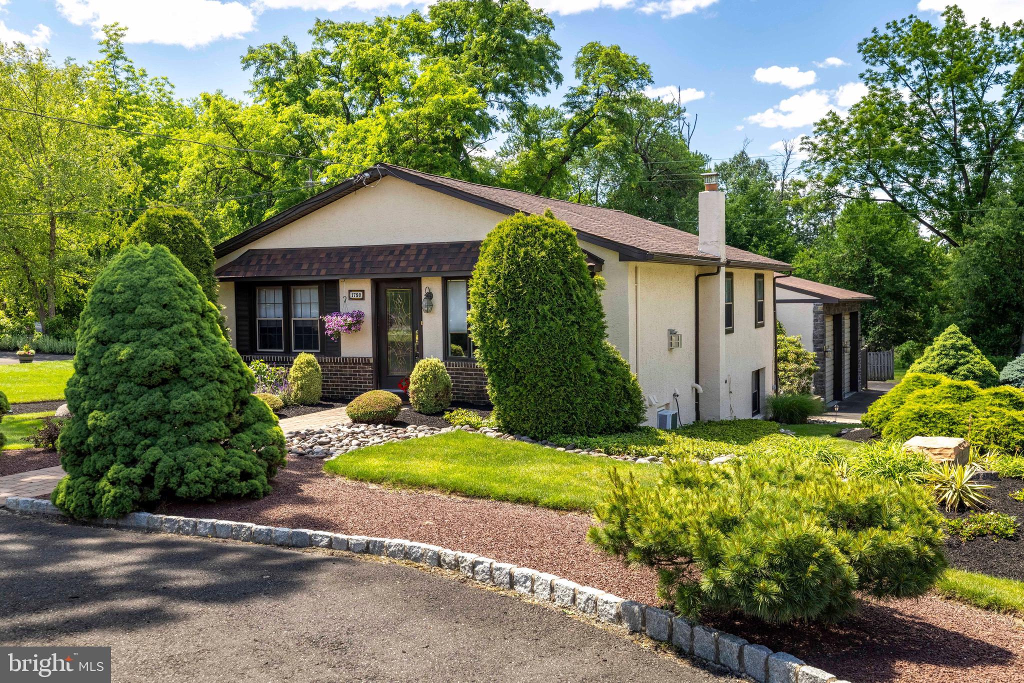 Set among beautifully maintained grounds in Upper Dublin Township, this distinctive 3-bedroom, 2.5-bath home offers exceptional flexibility, outdoor appeal, and rare garage/workshop space. The home features 1,260 sq. ft. above grade plus approximately 1,260 sq. ft. of finished walk-out lower-level space, creating far more usable living and work space than meets the eye. A circular driveway, mature landscaping, hardscaped paths, and welcoming exterior setting create a memorable first impression. Inside, the open concept first floor features vaulted ceilings, exposed beams, recessed lighting, and a propane fireplace with a dramatic stone surround.  The adjoining kitchen and dining area offers an easy flow for everyday living and entertaining, with white cabinetry, stainless steel appliances, granite counter, and a large island/breakfast bar. The deck is located directly off the kitchen, making it easy to step outside for grilling, relaxing, or enjoying the surrounding landscaping. The main level includes a comfortable primary suite with private bath, two additional bedrooms, and a hall bath.  The finished walk-out lower level is a major highlight, offering a separate exterior entrance to the rear patio, multiple finished spaces including an office with built-in fish tank;  laundry area with newer washer and dryer;  and a large half bath that could potentially be converted into a full bath to support an additional bedroom, guest suite, office, or extended living setup. The separate entrance also makes this level ideal for a contractor, small business owner, or anyone needing functional space apart from the main living area.  The oversized heated and cooled detached garage is another standout feature, complete with tall garage doors, high ceilings, rubber flooring, a gantry crane and extensive attached shelving/storage. Two additional large sheds with power provide even more storage at the rear of the property. Additional highlights include a newer boiler (a high efficiency combi boiler), generator for key elements, recessed lighting throughout, public water and sewer, and excellent overall versatility. Conveniently located near shopping, restaurants, Twining Valley Park, the regional rail station, and easy access to the Pennsylvania Turnpike, this is a rare opportunity for buyers who need comfortable living space, serious storage, and exceptional workshop functionality in Upper Dublin School District. (Basement family room is being sold "as is")