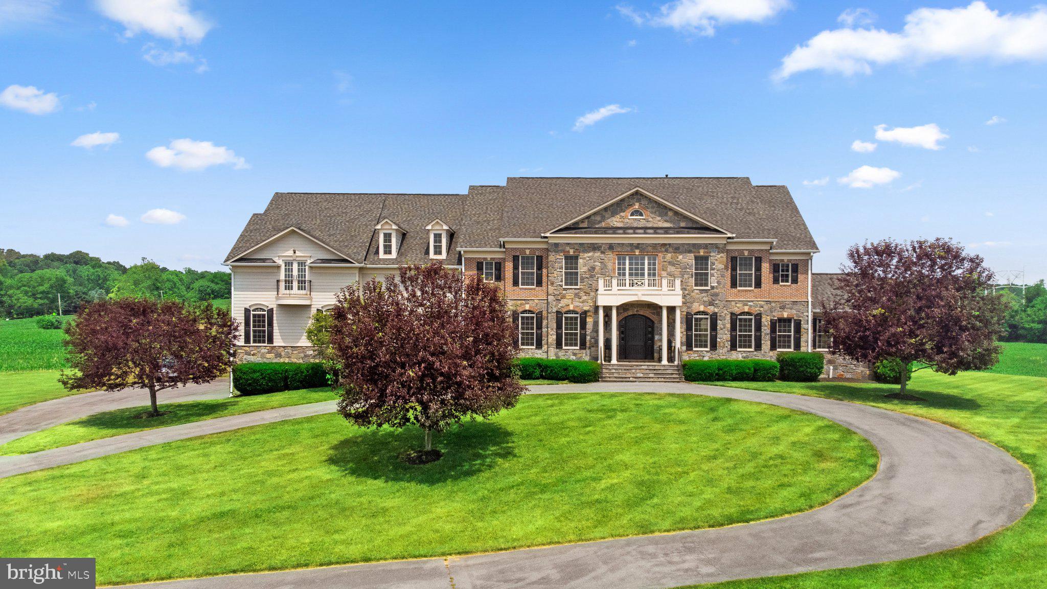 Welcome to this extraordinary custom-built stone estate, situated on over five private acres and offering an impressive 12,166 square feet of luxurious living space across four impeccably finished levels. Designed for grand-scale entertaining and refined everyday living, this remarkable residence showcases wood flooring on all three above-grade levels, complementing the home’s timeless craftsmanship and architectural elegance. With seven bedrooms—each with its own private bath—seven full baths, and two powder rooms, comfort and privacy abound. Five fireplaces, a whole-home entertainment sound system, and exceptional millwork further elevate the living experience. Car enthusiasts will appreciate the extraordinary 8-car, 42’ x 45’ garage featuring elevated ceilings, a car storage lift, and truly a rare offering, also equipped for a boat and/or RV storage. A dramatic two-story foyer with a graceful curved staircase sets the tone for the grandeur within. The foyer is flanked by an immense formal dining room and an elegant living room with a gas fireplace and arched openings. Beyond, the magnificent great room impresses with a soaring stone floor-to-ceiling fireplace and a wall of windows providing deck access and sweeping views. The gourmet kitchen is nothing short of spectacular, complemented by an oversized breakfast room. Additional main-level highlights include a distinguished formal library, a stunning sunroom with cathedral ceilings and abundant natural light, a mudroom, and two conveniently located powder rooms. Upstairs, the primary suite is a private sanctuary featuring a sitting room with a see-through fireplace, a wet bar with refrigerator beneath granite counters, a 16’ x 16’ fitness room with balcony access, and a lavish primary bath with dual lavatories. The suite is completed by a private second laundry room, exquisite millwork, and an extraordinary 25’ x 15’ custom closet space. The regal landing with iron rod railings overlooks both the grand foyer and great room below. Four additional expansive en-suite bedrooms—one featuring a stone fireplace—and a second laundry room complete this level. The lower level spares no expense and is designed for exceptional entertaining and relaxation, featuring a recreation room with a stone fireplace, a game room, an office/den, a full bath, a media room, and a stunning bar with expansive granite counters, a sink, a refrigerator, rich wood cabinetry, and seating for six. Walk-up stairs provide convenient access to the rear grounds. No detail has been overlooked in this extraordinary estate—a masterful blend of luxury, comfort, and architectural distinction.