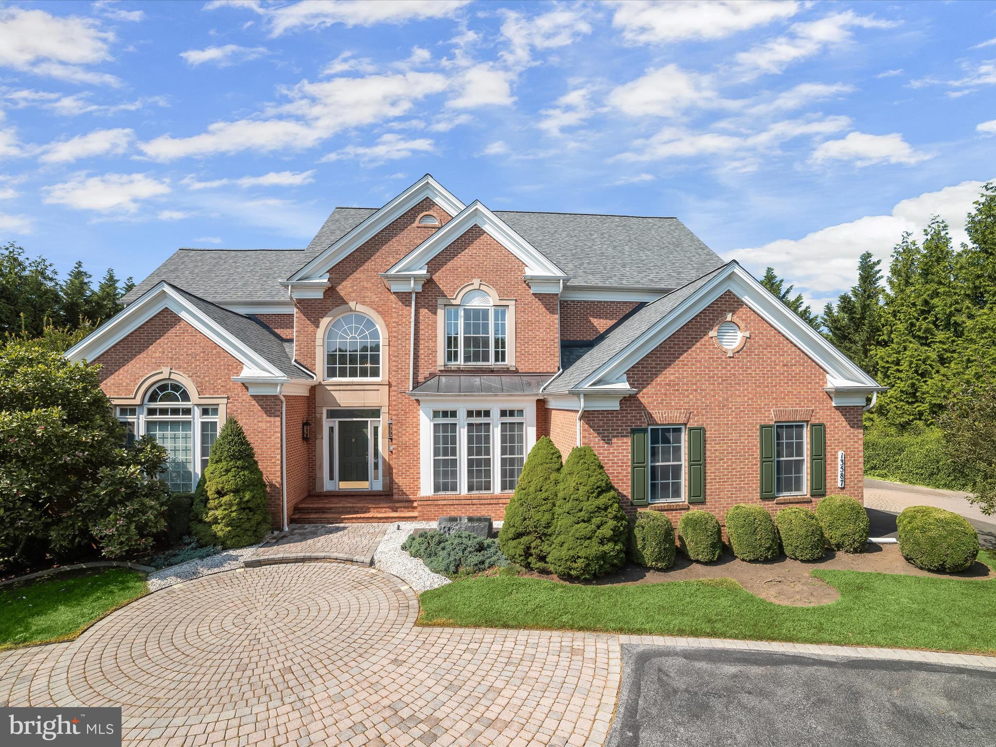 This exquisite brick estate, maintained by its original owners, offers more than 7,000 square feet across three finished levels, all nestled on nearly an acre of lush, private land. Blending timeless craftsmanship with luxurious amenities, the home presents a thoughtful balance of grand entertaining spaces and tranquil private quarters. With custom details, soaring ceilings, multiple fireplaces, a main-level primary suite, roof replaced in 2023, and even an interior sauna, this residence is as impressive as it is inviting. A stately circular driveway with a paver-stone approach welcomes you to the front entrance. Inside, the two-story foyer sets the tone with gleaming marble floors and elegant picture frame molding. To the right, the formal dining room mirrors these finishes and adds crown molding for a refined touch. To the left, a distinguished home office features a fireplace flanked by built-in bookcases and a striking coffered ceiling, ideal for work or study. At the heart of the home is the magnificent great room, where a soaring two-story ceiling and a wall of windows flood the space with natural light. An atrium door, framed by sidelights and topped with clerestory windows, opens to the rear deck, seamlessly connecting indoor and outdoor living. Anchored by a cozy fireplace, this room gives access into the open-concept kitchen, breakfast area, and family room, creating a unique layout perfect for both everyday life and elevated entertaining. The kitchen features 42-inch cabinetry with display space, granite counters, GE Profile stainless steel appliances including a gas cooktop and double wall ovens, a walk-in pantry, and a convenient breakfast bar. The adjoining family and breakfast rooms share a dual-sided fireplace with the great room and have a vaulted ceiling, offering another warm and welcoming gathering space. A butler’s pantry connects the kitchen to the formal dining room, and nearby, the laundry room and access to the three-car side-loading garage offer everyday functionality. The main-level primary suite is a luxurious retreat with double door entry, rich hardwood flooring, picture frame molding, a tray ceiling, and a sunlit bump-out sitting area. The spa-like primary bath includes a double sink vanity, a soaking tub, and a tiled shower with frameless glass, and direct access to two spacious walk-in closets. Upstairs, four generously sized bedrooms each feature walk-in closets. One has a private en-suite bath, and two of the bedrooms are connected by a shared full bath, offering comfort and convenience for family or guests.
The lower level evokes the ambiance of a high-end boutique hotel. Rich wood accents, sconce and pendant lighting, a sleek stone faux fireplace, and multiple sitting areas create an upscale lounge atmosphere with access to the backyard. A raised platform stage is perfect for at-home performances or karaoke nights. The wet bar with seating and a beverage refrigerator anchors the space, and the hardwired sound system enhances the experience. This level also includes a bonus room ideal for exercise or hobbies, a spacious hobby room with multiple potential uses, and a moody full bath complete with steam shower, heated floor, and a sauna large enough for multiple guests. There is also ample unfinished storage space for seasonal or long-term items. The backyard is a private, park-like escape. A large composite deck overlooks a winding paver walkway, detailed with inset landscaping, a decorative bridge, and mature plantings. This walkway leads to a second patio with a pergola, perfect for outdoor dining or quiet reflection. A six-foot fence encloses most of the backyard while maintaining views of the surrounding landscape and gardens. Additional features include a zoned HVAC, a side-loading three-car garage, and access to highly rated schools. Ideally situated and thoughtfully designed, this exceptional home offers luxury, comfort, and distinction in equal measure.