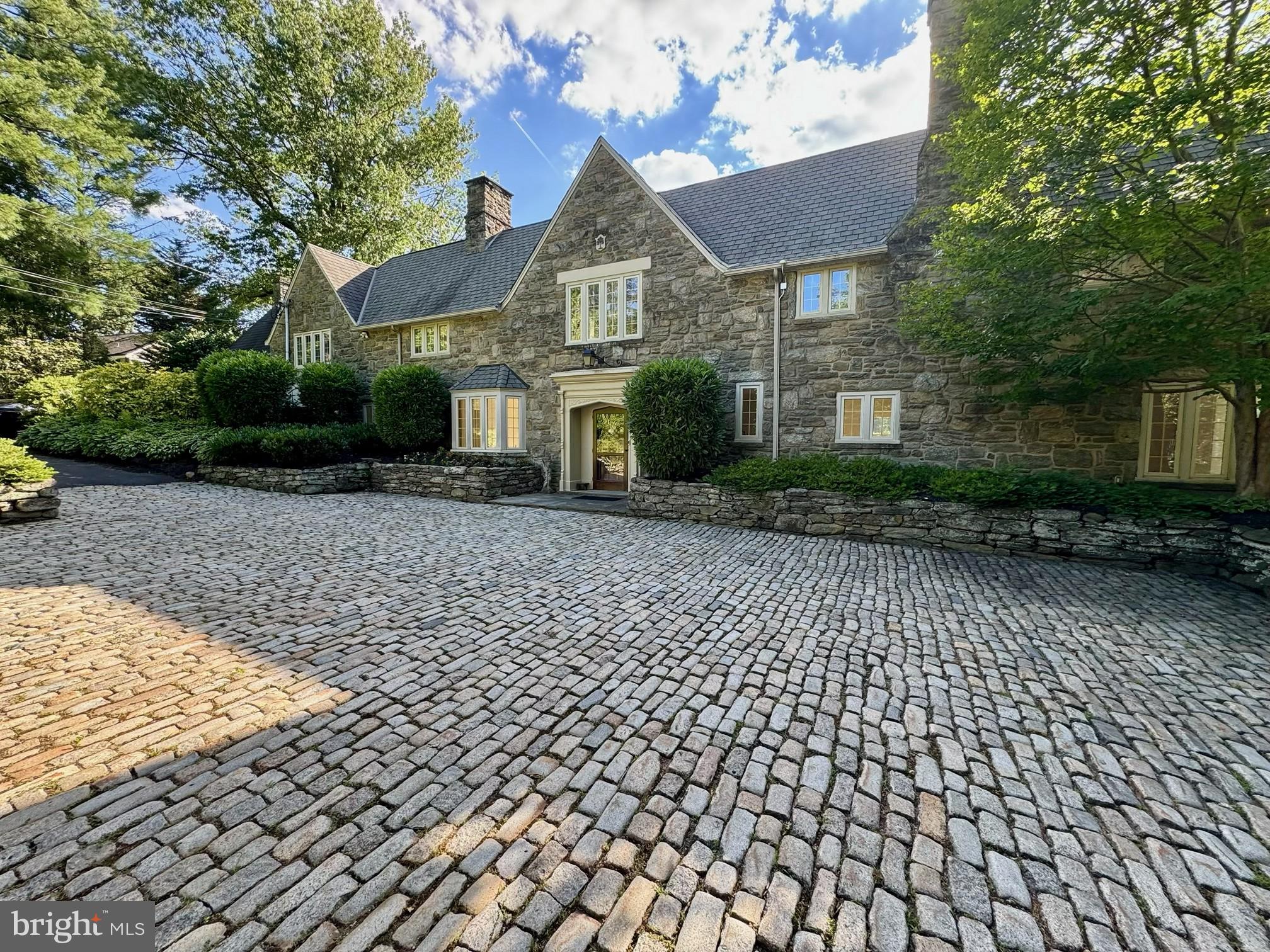 Set on one of Northside Haverford’s most prestigious lanes, this exceptional 1918 all-stone English Cotswold residence, designed by noted architect Walter Durham, blends timeless architecture with elegant living spaces and beautifully maintained grounds in a premier Main Line location.

Approached from the street through an impressive Belgian block courtyard and driveway, the home immediately conveys classic sophistication and architectural presence. A gracious foyer welcomes you inside and opens to beautifully scaled formal spaces designed for both entertaining and everyday living.

To the right, the elegant living room features a fireplace, beautiful bay windows overlooking the impressive grounds, and direct access to the rear flagstone patio. Adjacent is a distinguished wood-paneled library with its own fireplace, creating a warm and refined retreat. A conveniently located main-level powder room serves this wing of the home.

The bright formal dining room is filled with natural light through expansive five-window arrangements overlooking both the front and rear grounds and flows seamlessly into the gourmet chef’s kitchen. Designed for serious cooking and gathering, the kitchen features a Vulcan commercial-grade oven, Sub-Zero refrigerator, and stunning honed Calacatta Gold marble countertops. A practical mudroom, abundant closet space, and a full bathroom conveniently positioned for outdoor entertaining and pool use complete the first floor.

Upstairs, five spacious bedrooms and four full bathrooms provide exceptional accommodations. The luxurious primary suite offers peaceful views over the landscaped grounds, a separate alcove with custom built-in cabinetry, additional built-ins throughout the dressing and closet areas, and a private primary bath featuring double sinks and an oversized shower. A full room-sized upper-level laundry room and convenient rear staircase add functionality and ease to daily living.

Additional highlights include hardwood floors throughout, multiple zoned HVAC systems, and a full-size basement offering abundant storage and flexibility.

Outside, the property continues to impress with beautifully landscaped grounds featuring mature trees,  garden beds, and exceptional privacy. Tucked away from view, the lovely pool and pool area create a serene retreat surrounded by lush landscaping—an ideal setting for relaxing, entertaining, and enjoying the beauty of the seasons. Outdoor spaces are thoughtfully designed to offer both elegance and seclusion. Two separate garages complete this remarkable offering.

Ideally located just moments from Merion Cricket Club and offering exceptional convenience to the best of the Main Line, this home provides easy access to Bryn Mawr, Villanova, township parks, Center City Philadelphia, Philadelphia International Airport, and major commuter routes while maintaining the privacy and prestige of one of Haverford’s most sought-after neighborhoods.

A rare opportunity to own a distinguished Walter Durham-designed estate where historic character, exceptional craftsmanship, and elegant living come together.