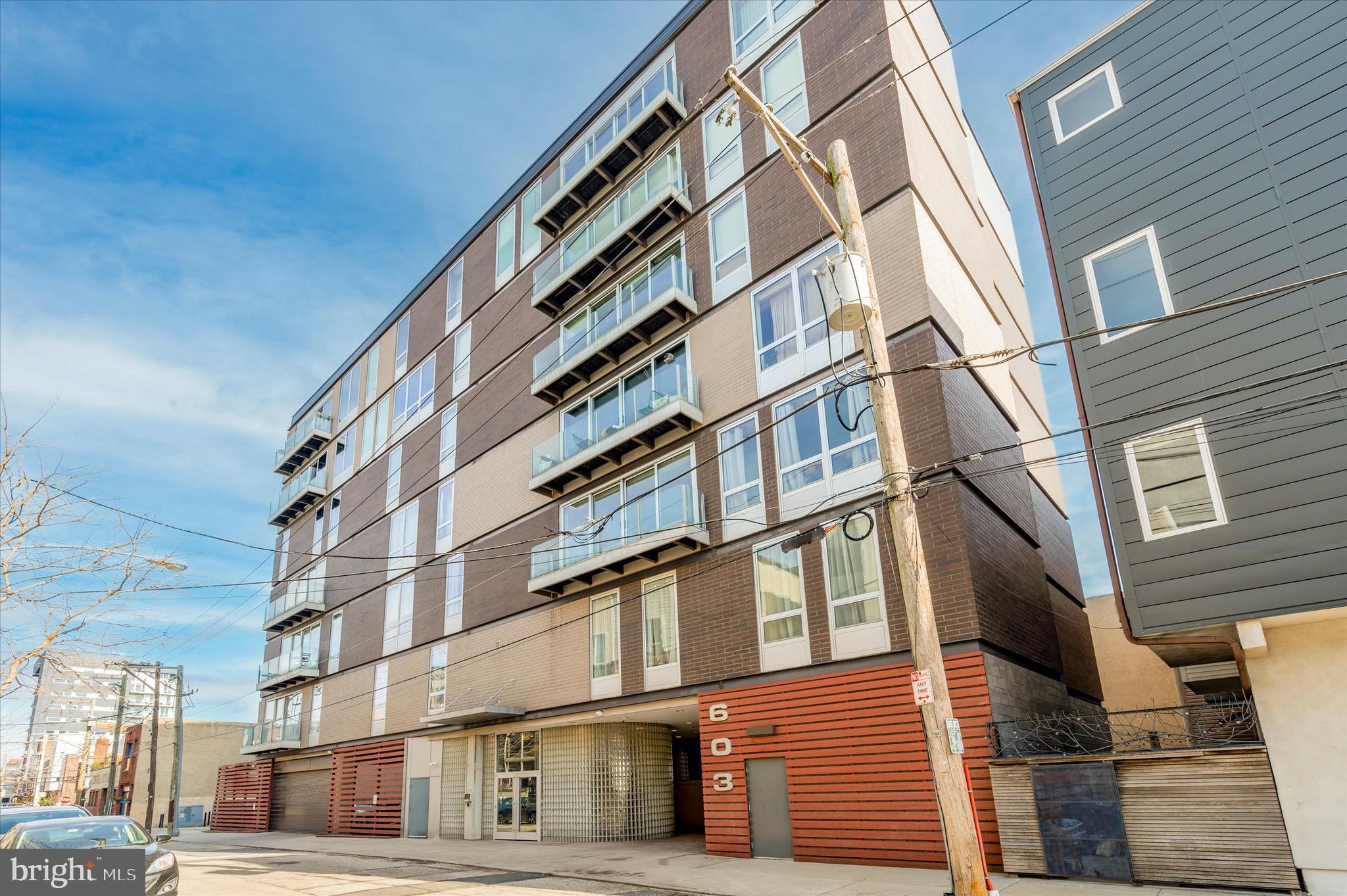 Rare opportunity to own a desirable, impeccably maintained corner split 2BR/2BTH unit in The L'eau Condominium so close to everything Northern Liberties has to offer.   This decidedly modern  2009  brick 7 story mid-rise building was designed by architect Erdy McHenry.  There is a total of 24 "flats",  4 per floor on floors 2-7,  with minimal shared walls between units and poured concrete between floors.   603 has a gated on-site ground level on-site assigned covered 1 car parking space.   Gracious  lobby with street entry, stairwell (one of two) and elevator, door to parking lot.  Inside 603 , experience  extraordinary space with 1,455 square feet,  10' ceilings, 8' windows, beautiful custom kitchen and baths, upgrades and amenities  including custom shades, window privacy filters, Lutron Caseta smart light switch system , ecobee thermostat, custom closets/storage and each bedroom has a walk-in closet.  There are truly awesome city views from any window or from the living room balcony.  Entry hall with large storage/pantry  closet, mechanical closet, small side hallway with coat closet to main bedroom suite.  Convenient full hall bath shared with bedroom 2.  From the entry hall area step into an inspiring open living/dining/kitchen space with outstanding scale and light.   Fantastic well thought out center island Kitchen with quality finish details and appliances, perfect for both every day and entertaining.  Walk-in laundry/storage  closet with tile floor, tall privacy glass  window.  Open dining area adjacent to the kitchen.  Large, wide and deep living area which allows for flexible furniture placement and great wall space for art; there are concealed window roller shades.  Light filled primary bedroom with window wall and motorized black out window shades, walk-in closet with tall privacy glass window.  Great looking primary tile bath with big walk-in shower with frameless glass door,  double vanity sink, wall of California Closet storage cabinetry -- drawers/shelved/hanging closets.   Bright 2nd bedroom with 8' high window with motorized blackout shade and custom walk-in closet, door to second bath.  Crisp, bright second bath with beautiful tile,  tub with tile surround, vanity sink,  deep shelved linen/storage closet.   603 is sleek and sophisticated yet offers  an inviting  subtle warm retreat sensibility;  it is deluxe, delightful and in truly move-in condition. This  location is really close to neighborhood restaurants, bars, brewpubs, chain and independent coffee shops, bakeries, easy food shopping, gyms, galleries, music venues, people and dog parks.  Minutes  to nearby Fishtown, Old City, Penn's Landing and the developing waterfront attractions/parks/trails.  Septa bus transit and the  Market-Frankford line, I-95 and major roads are all just minutes away.