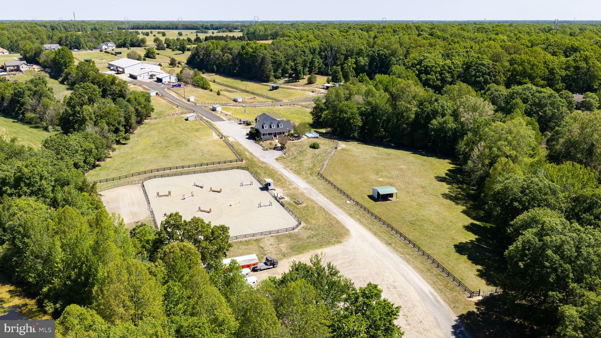 Set among rolling hills and framed by mature trees, EKG Stables at Hill Valley Farm presents an exceptional opportunity for the serious horse enthusiast, trainer, boarding operation, or equestrian entrepreneur seeking a fully established facility with both scale and functionality. Located at 5 Appaloosa Drive, this 36.21-acre property has been thoughtfully developed to support a wide range of equestrian disciplines and operations, all within a private and picturesque setting. A tree-lined drive winds through the neighboring community before opening to 19 fenced paddocks, wonderful pastureland, and a pond complete with dock access. The farm was built by the trainer's father and has been loved and cared for by the family since the beginning. It was originally envisioned as a continuation of the surrounding community, yet today it stands as a destination unto itself and is now ready to be passed on. Hill Valley Farm has evolved into a property capable of accommodating training programs, boarding operations, clinics, and horse shows. Designed with both horse and rider in mind, the farm features three-board fenced paddocks, each equipped with individual water access and run-in sheds. A shaded riding trail extends from the original barn to the water’s edge, creating a peaceful setting for a leisurely stroll to the water. Two barns anchor the equestrian improvements. One expanded barn offers 13 stalls and operational flexibility, while the larger barn has 16 stalls and incorporates a one-bedroom, one-bath apartment with living room and kitchen space, ideal for staff, trainers, guests, or additional rental opportunities. Additional improvements include a hay shed, generous gravel drive & parking areas for trailers and equipment, and a 100x200 indoor arena perfectly suited for year-round riding, lessons, training, clinics, and hosting equestrian events or shows. The overall layout creates a turnkey environment for both private enjoyment and professional equestrian pursuits. Outdoor spaces throughout the farm have been carefully considered, from the peaceful pond and shaded trails to elevated hilltop vantage points offering sweeping sunset views across the surrounding countryside. The setting provides the kind of privacy, beauty, and usability that is increasingly difficult to find in today’s equestrian market, especially one so close to town. The residence itself has been fully renovated and offers comfortable, updated living with flexibility for a variety of needs. The 4,600+ square foot brick cape cod features refinished pine flooring, a remodeled kitchen with stainless steel appliances and updated finishes, renovated bathrooms, multiple living spaces, and a fully finished lower level with additional kitchen area and gathering space. An attached apartment above the garage provides even more versatility for guests, staff, multigenerational living, or supplemental income potential. Major mechanical systems throughout the property, including updated HVAC systems, and a new well pump connected to a 565-foot-deep well source, have been refreshed within the past three years. Oh, and the roof is new! Despite its peaceful and private setting, this property remains remarkably accessible, located within approximately 15 minutes of Cosner’s Corner and I-95 access at both Massaponax and Thornburg, and less than 30 minutes from downtown Fredericksburg and Lake Anna State Park. Hill Valley Farm offers the rare combination of a professionally equipped equestrian facility, multiple housing opportunities, and the natural beauty and infrastructure necessary to support a true horse-centered lifestyle or business.