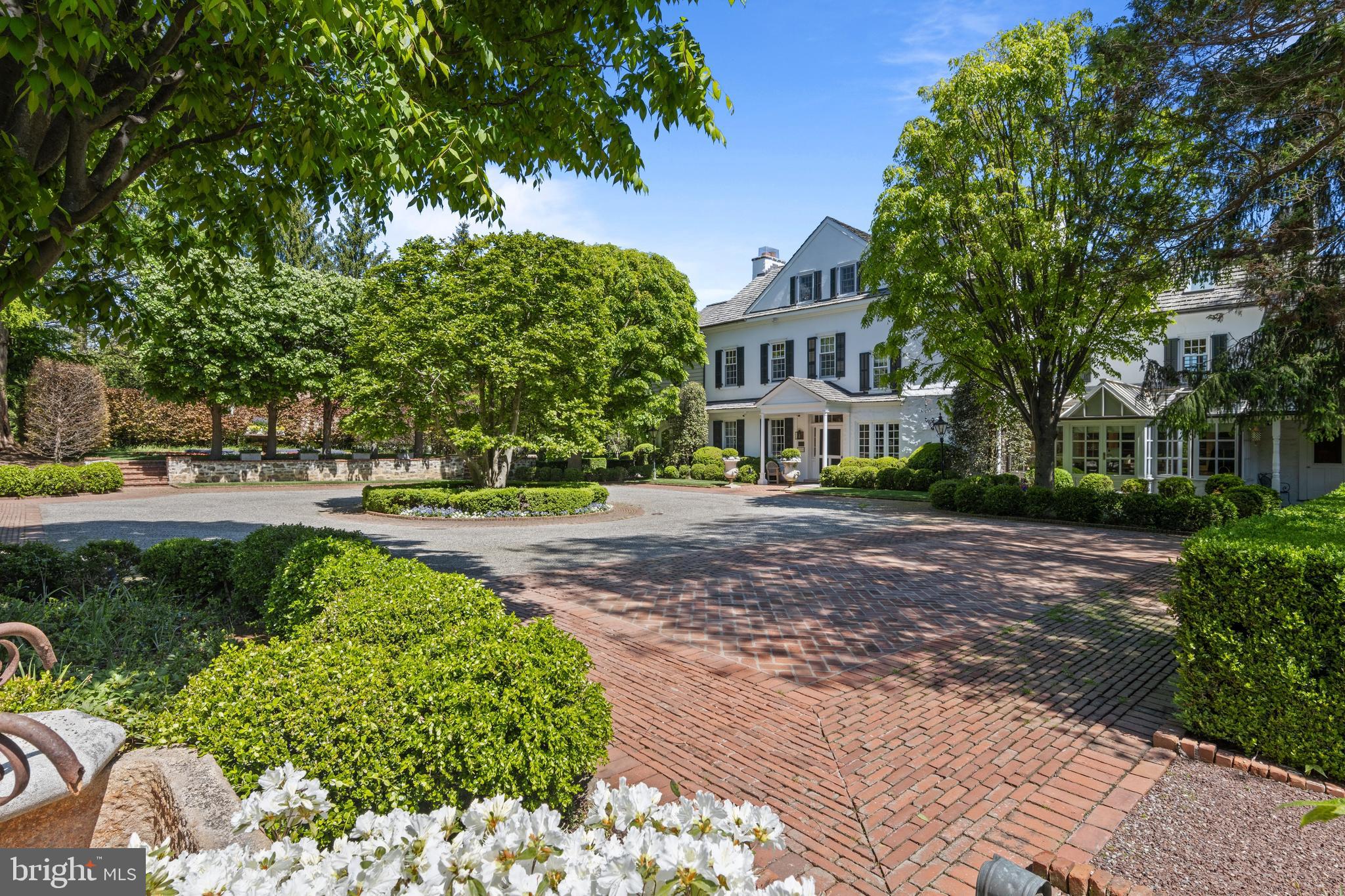 One of only six residences along a private Gladwyne lane, 1320 Huntsman Lane is a quietly masterful composition—where architecture and landscape are conceived as one continuous experience, and where restraint, proportion, and craftsmanship define its character.
A painted white stone farmhouse anchors the end of a wide gravel court, the approach unfolding in glimpses. A beech lawn, enclosed by mature trees and patterned with a restrained formal garden, introduces the first of many outdoor rooms. Elsewhere, a stone wall with an arched opening leads to a more intimate enclosure and a separate structure suited for a studio, gym, or private office—each element placed with intention rather than display.
Inside, the home honors its origins while elevating them. A straight-through foyer with richly stained original floors opens to terraced gardens beyond. Principal rooms balance refinement with ease: a living room extends to a screened garden space overlooking a formal walk of towering trees and cutting gardens; a fireside library offers quiet contrast; and a dining room opens seamlessly to a bluestone terrace. A glass-wrapped solarium adapts effortlessly to daily life, always oriented toward the landscape.
The kitchen and adjoining spaces continue this dialogue. Substantial materials—wide-planked floors, marble surfaces, professional appliances—are paired with uninterrupted views outward. A glass-enclosed breakfast room opens to a wisteria-covered pergola with a fireplace, creating a space defined as much by nature as by structure. Nearby, a large family room offers a more relaxed counterpoint, with a detailed wood ceiling, wraparound windows evoking a treehouse-like setting, and a fireplace with concealed media—equally suited for gathering or retreat.
Upstairs, an arched stair window frames the symmetry of the gardens below. The primary suite is warm and composed, with thoughtfully divided baths, tailored dressing spaces, and views to the cutting gardens. Additional bedrooms are generous and well-appointed, while a private guest suite and upper-level retreat provide flexibility for extended stays. A light-filled gym, defined by exposed stone and high ceilings, completes the interior.
Here, the grounds are not ancillary; they are integral. A sequence of garden rooms unfolds along stone and brick paths that reveal rather than present. A grass tennis court, enclosed by intricate lattice fencing, is both refined and restrained, with a charming shed positioned along its center line. An allée of trees leads to the pool—rectangular, softened by a waterfall and balanced by curved seating—while two stone pavilions, seamlessly integrated, shelter dining and a waterfall-edge hot tub.
A fire pit and a discreet clock tower with bath and changing space allow days to extend fully outdoors. Specimen plantings, antique garden elements, and thoughtfully placed lighting lend a sense of permanence, while centennial brick and stone paths ground the composition.
At 1320 Huntsman Lane, beauty is not singular or immediate—it is cumulative, revealed gradually through movement, season, and time.
