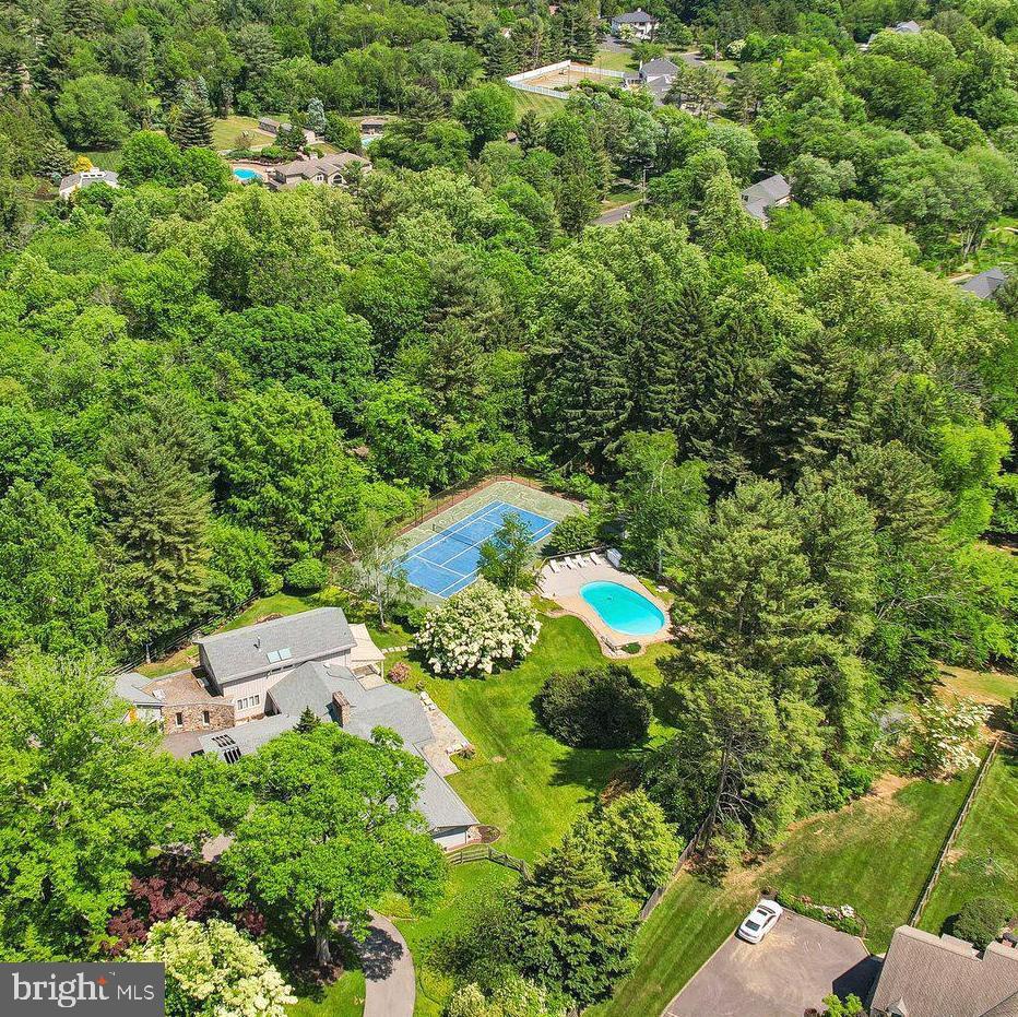 Introducing The Estate on Paper Mill, a rare private residence where architectural character, Mid-Century Modern influence, and resort-style living come together on 1.75 beautifully landscaped acres. Set in one of Meadowbrook’s most desirable locations, this distinctive 5-bedroom, 4.5-bath home offers over 4,800 square feet of living space, a saltwater pool, private tennis court, mature gardens, and exceptional indoor-outdoor living. 

A glass entry introduces the home’s striking personality and opens to a dramatic vaulted great room with soaring ceilings, a wall of windows, parquet wood floors, a gas-burning stone fireplace, wet bar, and direct access to a flagstone patio overlooking the private rear grounds. Thoughtfully oriented toward the backyard, the home is filled with natural light, garden views, and seamless access to outdoor living spaces.

The first-floor primary suite is a true retreat with serene views, a sitting room with built-in bookcases, walls of windows, multiple walk-in closets, and two separate baths. The formal dining room seats twelve and features a skylight, built-in china cabinetry, and generous storage.

The kitchen blends warmth, function, and professional-grade performance with white cabinetry, butcher block countertops, a large island with seating, vegetable sink, pantry, sitting area, window seat, and premium appliances including a 6-burner Wolf range, Sub-Zero refrigerator and freezer, Miele oven, and Bosch dishwasher. Direct access to the covered patio makes outdoor dining effortless.

Additional first-floor spaces include a family room with Amish-crafted built-in desks, a cubbied mudroom, and laundry room with Miele washer and dryer leading to a fenced vegetable garden. Upstairs, four additional bedrooms offer large windows, organized closets, and access to two full baths.

Beyond the heated two-car garage are rare bonus spaces including a bike room, workshop, garden room, and upstairs studio ideal for an office, fitness room, art space, or quiet retreat.

The grounds are the signature. Cultivated over decades, the property features mature trees, lush landscaping, flagstone paths, a fenced rear yard, saltwater pool redone in 2021, expansive lounging deck, storage/bar area, and views toward the private tennis court. Whether entertaining, swimming, playing tennis, gardening, or relaxing on the patio, this property offers a private resort lifestyle rarely found in Meadowbrook.

Additional amenities include a whole-house generator, drainage system, deer fencing, 5-zone heating and air, expanded circular driveway with carport, alarm system, tennis storage shed, and extensive storage throughout. Conveniently located near train lines to Center City, Pennypack trails, Huntingdon Valley Country Club, hospitals, and within the Abington School District.