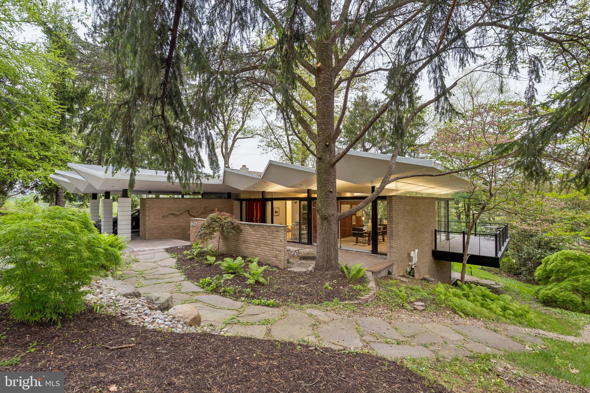 Set at the end of exclusive Monk Road on the cul-de-sac, this Midcentury Modern masterpiece by noted architect Irwin Stein is a rare expression of thoughtful design, natural beauty, and timeless livability in the heart of Gladwyne. Built into a picturesque hillside overlooking wooded surroundings above the Schuylkill River, the residence embraces its setting through expansive glass, abundant exposures, and a seamless connection to landscape from nearly every room.  The dynamic "folded plate" roof, a signature of Steins, appears to float above the home.

A paved patio leads to the ground-level entrance, where a bright and welcoming foyer immediately showcases the home's generous proportions and architectural character. Original details blend effortlessly with tasteful updates, while Stein’s signature approach to light and sightlines is evident throughout—framing mature trees, natural foliage, and long views at every turn.

The main level offers an ideal everyday layout. The primary suite is privately positioned and includes an ensuite bath and copious closets. Two additional bedrooms on this floor enjoy large windows, tranquil views of the property, and share a full hall bathroom. Nearby, the updated kitchen, clad on three sides with original Walnut boards, features granite countertops, stainless steel appliances, and an electric cooktop, while the adjacent dining room is perfectly placed for both casual meals and entertaining. There is also an expansive, sunken living room highlighted by a fireplace, butt-glazed corner glass windows and a surrounding deck. 

Downstairs, a more intimate family room creates a warm and inviting gathering space centered around a cozy fireplace. Designed for entertaining and relaxed living alike, this level also includes two additional well-sized bedrooms sharing a full hall bath, offering flexibility for guests, offices, or fitness needs.  There is also an expansive bonus room ready to be made into a home gym or craft center and the original bomb shelter (the home was designed in the sixties!) ready to be converted into a wine cellar.  

Glass doors open directly onto an organically shaped custom patio with unique rock formations that catch the water as it plunges from the roof on rainy days; it's where the home’s indoor-outdoor lifestyle truly shines. A few steps down into the yard, a heated in-ground pool set against a dramatic stone wall provides the perfect summer retreat.

Completing the property is a covered carport equipped with a Tesla electric charger, thoughtfully integrated for modern convenience. Surrounded by wooded scenery and elevated river views, this exceptional residence offers a rare opportunity to own a true architectural gem in one of the Main Line’s most coveted settings.